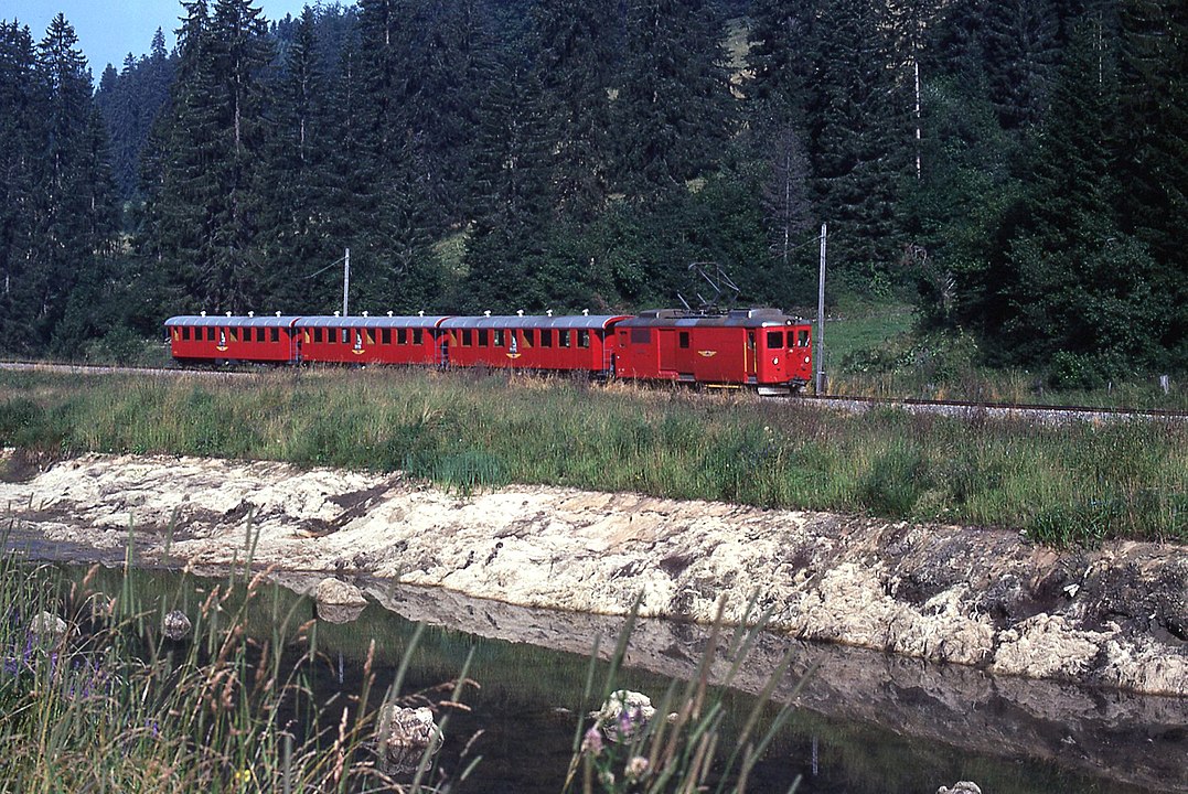 Personenzug im Jahr 1977 mit Gepcktriebwagen De 4/4 und Wagen B 761–763 mit offenen Plattformen zwischen Pr-Petitjean und La Combe (Quelle Wikipedia, Bild Alain GAVILLET, CC BY 2.0)