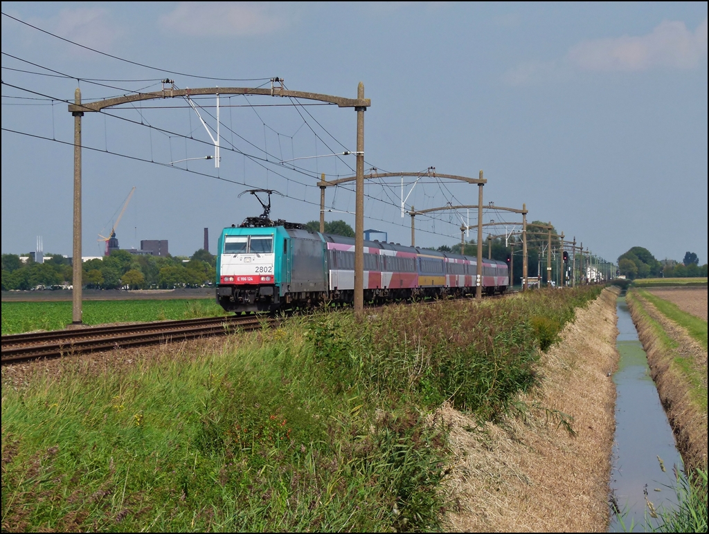 Am 03.09.2011 zieht die Traxx 2802 einen IC B (Benelux) Amsterdam – Bruxelles durch die sch�ne niederl�ndische Landschaft zwischen Oudenbosch und Zevenbergen, wo es noch die tollen alten Fahrleitungsmasten gibt. (Jeanny)

Dieser st�ndlich verkehrende Zug, welcher die belgische Haupstadt mit Amsterdam und vice versa verband, gibt es nicht mehr. Die 7,5 Milliarden Euro teure niederl�ndische Hochgeschwindigkeitsstrecke sollte besser ausgelastet werden und so bestellte man in Italien (!) bei AnsaldoBreda Triebz�ge, welche den bew�hrten IC Benelux ersetzen sollten und auf der HSL-Zuid fahren konnten. Nach 5 Jahren (!) Testfahrten, sollten die V 250 jetzt endlich am 09.12.2012 zum Einsatz kommen und zwar nicht mehr st�ndlich, sondern nur noch alle 2 Stunden. In der ersten Woche erreichte nur 1 Zug von 4 sein Ziel. Viele wichtige Bahnh�fe werden nicht mehr bedient (Roosendal, Dordrecht, Den Haag) und zu allem �bel brauchen den Fahrg�ste f�r jede Fahrt mit dem Fyra eine Reservation. Da diese Z�ge besonders in den Niederlanden t�glich von vielen Pendlern benutzt werden, grenzt das schon an Schikane. 

Die Tatsache, dass die niederl�ndische Hauptstadt nicht mehr von diesem Zug bedient wird, war wohl ausschlaggebend, dass er nun wieder eingestellt wurde. Der gute alte IC Benelux soll wieder st�ndlich fahren, aber leider sind die Loks schon weg. Da die Traxx nur gemietet waren, wurden sie bereits an andere Gesellschaften weiter vermietet und jetzt bem�ht man sich die Loks wieder nach Belgien zu holen. Sie sollen am 7. oder 8. Februar zur�ckgef�hrt werden.

Seit dem Bestehen (1980er Jahren) des IC Benelux bestand der Zug aus einer belgischen Lok und niederl�ndischen IC Wagen mit Steuerwagen. Damals wurde sogar extra f�r diesen Zug eine Baureihe in Belgien gebaut, die S�rie 11, die sich durch ihre Fargebung von den anderen belgischen Baureihen unterschied. Die sogenannte Livr�e Benelux (Bordeaux rot und beige) passte farblich zu den niederl�ndischen IC Wagen und verlieh so dem Zug ein einheitliches Aussehen. http://www.rail-pictures.com/name/train-photo/9547/gallery/Belgium~Electric+locomotives~Serie+11.html Diese sch�nen Loks wurden sp�ter durch die Traxx ersetzt und die Wagen hatten auch nicht mehr alle dieselbe Farbgebung, daf�r war der Zug bunter geworden und war vor allem sehr beliebt bei den Fahrg�sten.
