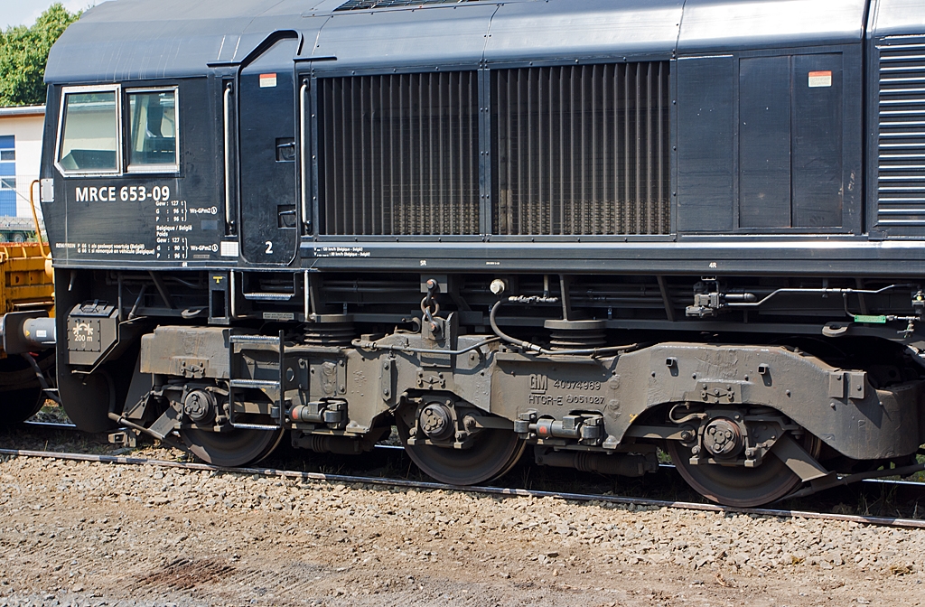 Detail eines m�chtigen dreiachsigen HTCR-E Drehgestelles der Class 66.
Hier der MRCE 653-09 (92 80 1266 119-7 D-DISPO) eine EMD JT42 CWRM (Class 66/9) am 13.07.2013 in Ehringshausen (Lahn-Dill-Kreis).
Die dreiachsigen HTCR-E Drehgestelle verf�gen �ber gegenl�ufig radialgelenkte Endachsen, die Mittelachse ist seitenverschiebbar, diese erm�glichen den Betrieb dieser insgesamt 6-achsigen-Lokomotive (sie haben 2 Drehgestelle) auf Strecken die in der Regel auf 4-achsige Lokomotiven eingeschr�nkt sind.

Weitere Vorteile sind:
- Kleinster befahrbarer Radius der Lok ist so 80 m
- Die seitlichen Schiene-Kr�fte sind dadurch auch gesenkt
- Geringere Gefahr von Entgleisungen
- Reduzierter Verschlei� der Komponenten, somit erstreckt sich das Drehgestell �berholungsintervalle auf 1,6 Mio. km