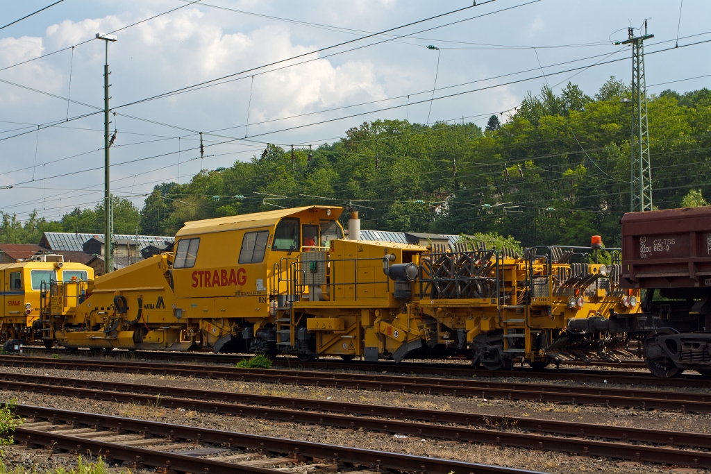 Die MATISA R24 Schotterplaniermaschine der STRABAG Rail GmbH (Schweres Nebenfahrzeug Nr. 99 80 9225 001-3 D-STRA) ist am 30.05.2012 in Betzdorf/Sieg abgestellt.

Die Maschine wurde 2009 von der MATISA Mat�riel Industriel S.A. in Crissier (Schweiz) unter der Fabrik-Nr. 47051 gebaut.

Die R 24 ist eine Hochleistungs-Schotterplaniermaschine auf Drehgestellen, speziell konzipiert f�r den Bau und den Unterhalt der Hochgeschwindigkeitsstrecken. Ihre beiden Kehrbesen garantieren eine ausgezeichnete Kehrleistung bei einer Geschwindigkeit von +/- 6 km/h.
Der erste Kehrbesen f�r die Strecke, best�ckt mit einem L�ngsf�rderband, sammelt den �bersch�ssigen Schotter auf den Schwellen und transportiert ihn mit dem F�rderband  in das15 m� gro�e Silo. So kann �bersch�ssiger Schotter zur�ck gewonnen und in Bereichen mit Schottermangel verteilt werden. Die 4 unabh�ngige Schotterhosen unter dem Silo verteilen den Schotter vor den Pfl�gen, welche diesen im gleichen Arbeitsgang auf dem Gleis verteilen. Der zweite Kehrbesen, f�r Weichen, ausger�stet mit einem Querf�rderband, verteilt den Schotter zur linken und rechten Seite. Mit seiner sehr ger�umigen Kabine, die auch an spezifische Kundenw�nsche angepasst werden kann, bietet die R 24 einen gro�en Komfort.

Die Maschinen sind mit einem hydrostatischen Fahrantrieb ausgestattet, der einfach und bequem zu bedienen ist. Die Fahrgeschwindigkeit kann ohne Rucken durch Schaltvorg�nge gesteuert werden. Das ruckfreie Fahren erh�ht den Komfort und ist ein Gewinn f�r Mensch und Maschine, und das jeden Tag. Ein weiterer Vorteil des hydrostatischen Fahrantriebs ist, dass ein Schlupf der R�der beim Anfahren verhindert wird.

TECHNISCHE DATEN: 
Spurweite: 1.435 mm  (Normalspur)
Achsanzahl: 5 (2 Drehgestellen, eine einzelne Achse)
Achsformel: Bo´ + A1´ + 1
L�nge �ber Puffer: 26.500 mm
Drehzapfen- bzw. Achsabstand: 12.500 mm / 8.000 mm
Achsabstand in den Drehgestellen: 1.800 mm
Treib- und Laufraddurchmesser: 920 mm (neu)
H�he: 4.263 mm
Breite: 3.050 mm
Eigengewicht: 68.420 kg
Anh�ngelast: - t
Zur Mitfahrt zugel. Personen: 5
H�chstgeschwindigkeit (geschleppt): 100 km/h 
H�chstgeschwindigkeit Eigenfahrt: 25 km/h (nur als Rangierfahrt)
Max. Geschwindigkeit beim Planieren: 15 km/h
Max. Geschwindigkeit beim Kehren: 6 km/h     
Zugelassen ab Streckenklasse: C2 
Kleinster befahrbarer Kurvenradius:  R 250 m  (Fahrzeug allein 90 m)
Min. Radius bei Arbeit: R 190 m
Bremse: 2 x KE-GP (K), Max. 57 t
Dieselmotor:  DEUTZ wassergek�hlter V8-Zylinder-Viertakt- Dieselmotor mit Turboaufladung, Ladeluftk�hlung, Vierventiltechnik und wassergek�hlte Abgasrohre vom Typ DEUTZ BF 8 M 2015 CP 
Motorleistung: 440 kW (598 PS) bei 2.100 U/min
Motorhubraum: 15,9 Liter (Bohrung 132 mm / Hub 145 mm)
Motorgewicht: 1.060 kg
Gr��e Schottersilo:15 m�  (Standard 10 m�)
Tankvolumen: 3.000 Liter  (Standard 2 m�)

Bemerkung: Laut Prospekt von Matisa kann die Maschine in Eigenfahrt auch 100 km/h schnell fahren (dann hat sie nur 2 Achsen angetrieben), aber laut Anschriftentafel ist eine Eigenfahrt nur als Rangierfahrt mit 25 km/h zugelassen.
