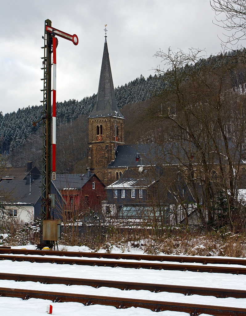 Einfl�geliges Form-Hauptsignal (hier auf Hp 0 „Halt!“) als Ausfahrtsignal  (in Richtung Betzdorf) am Gleis 1 vom Bahnhof Herdorf (09.02.2013). 

Unten links am Bildrand das Signal Ra 12 / So 12 (Grenzzeichen), dies zeigt die Grenze an , bis zu der Fahrzeuge bei Weichenverbindungen profilfrei abgestellt werden d�rfen.
Bei Weichenverbindungen, an der ja zwei Gleise zusammenlaufen, ber�hren sich die Lichtraumbereiche beider Gleise. Der Punkt, an dem sie sich gerade ber�hren, ist dieses Zeichen gekennzeichnet. Bis zu diesem Zeichen d�rfen Fahrzeuge abgestellt werden, ohne da� Fahrzeugbewegungen im Nachbargleis behindert werden.

Im Hintergrund die katholische Kirche St. Aloisius.
