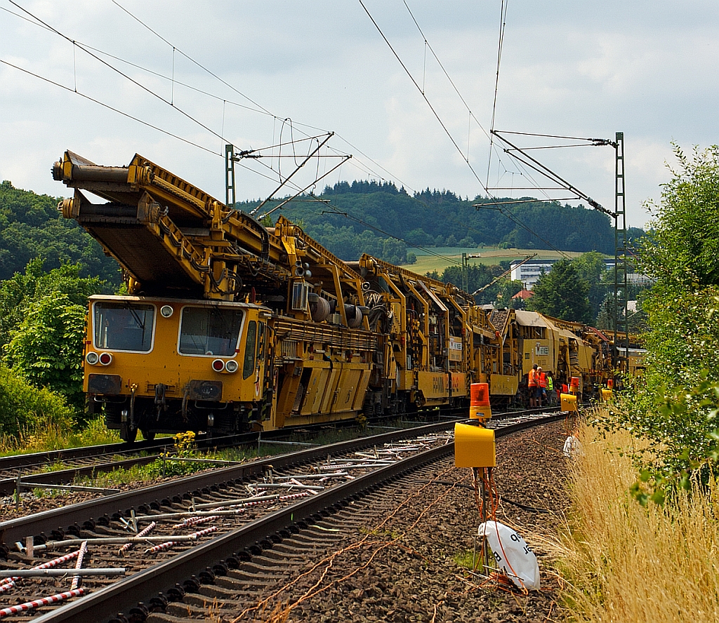 
Plasser & Theurer Planumsverbesserungsmaschine RPMW 2002–2 der GBM Wiebe Gleisbaumaschinen GmbH, Schweres Nebenfahrzeug Nr. 99 80 9415 002–1 am 13.07.2013 bei Katzenfurt (Lahn-Dill-Kreis) an der KBS 445 (Dillstrecke). Die Maschine steht, da die MSF-Wagen mit Abraum voll waren und entladen werden m�ssen.

Der gro�e Unterschied zwischen Planumsverbesserungsmaschine und Bettungsreinigungsmaschinen besteht darin, dass Planumsverbesserungsmaschine nicht nur den Schotter ausheben und recyceln kann sondern auch einen Teil Planums (Unterbau) ausheben (bis 1.200 mm unter SO). Zudem kann die RPM vor der Neuschotterung (Recycling- mit Neumaterial) auch eine Planumsschutzschicht (PSS-Material) einbringen.

Die RPM 2002 – 2 ist die hat ein Gewicht von 560 t und hat eine L�nge �ber Puffer von 140 m. Die Motorengesamtleistung betr�gt 2.860 PS / 2.100 kW die aber weniger der Fortbewegung dienen, sonder zur Erzeugung der hydraulischen und elektrischen Energie.

Der Neuschottern wird durch die Stopfeinrichtung 09-32 Stopfsatellit das Gleisbett verdichtet und ist danach wieder mit 70 km/h befahrbar.

