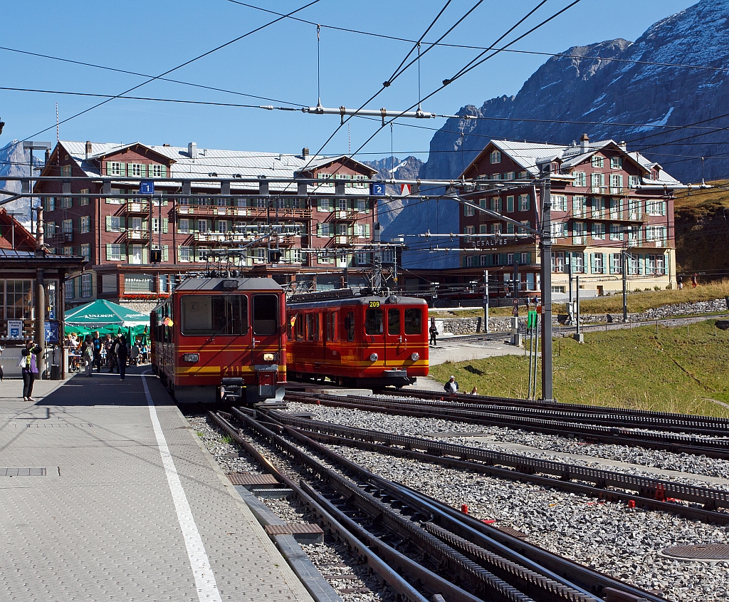 Vor der Kulisse des Hotel Bellevue des Alpes: Triebzug (2 gekuppelte BDhe 4/8) der Jungfraubahn vorne Triebwagen Nr. 214 hinten 211 verl�sst am 02.10.2011 den Bf Kleine Scheidegg (2064 m. �. M.), und f�hrt hinauf zum Jungfraujoch. Rechts abgestellt Dhe 2/4 Triebwagen Nr. 209 mit Steuerwagen Bt 33.