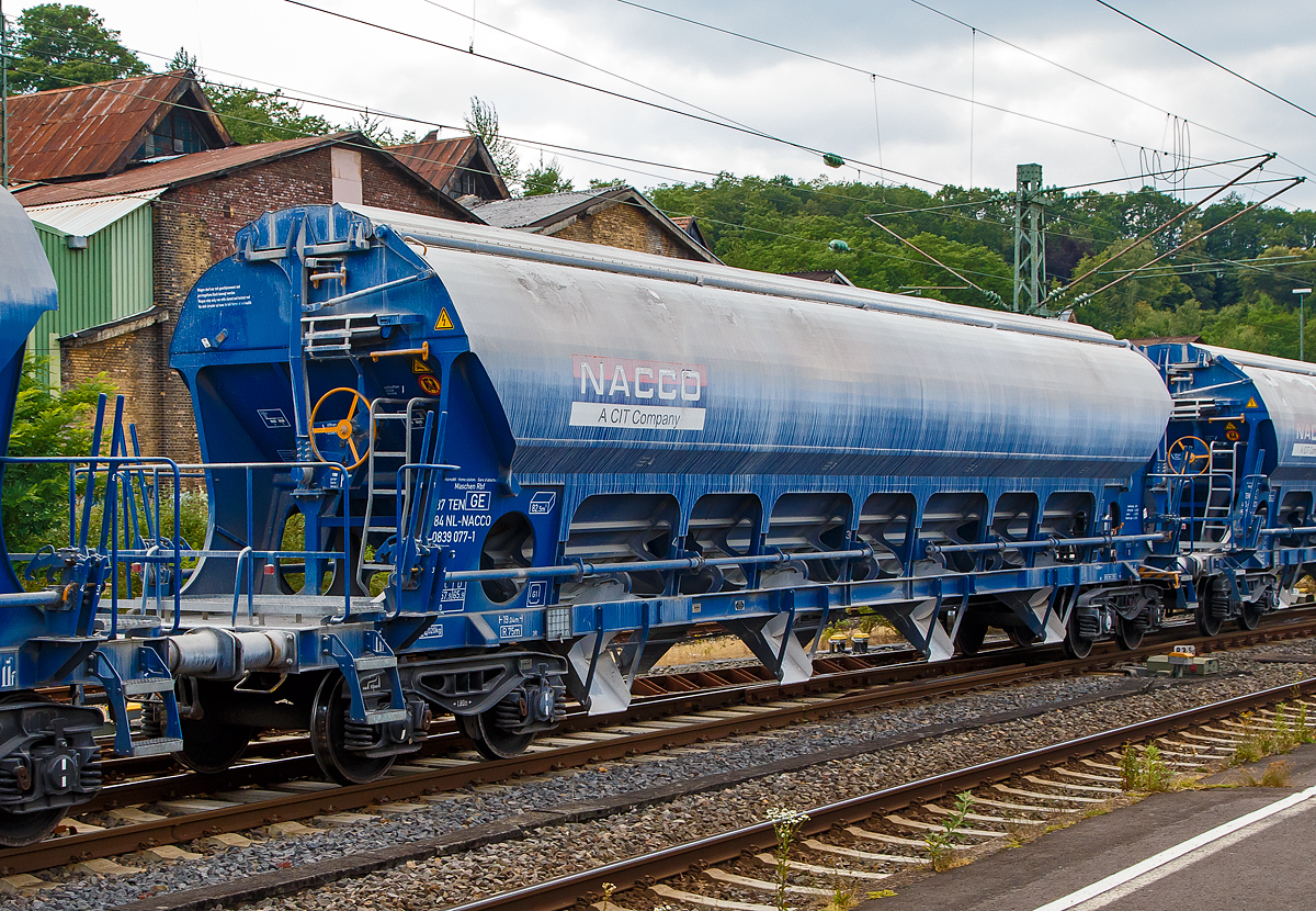 4-achsiger Trichtermittenentladewagen 82,5 m³ der Gattung Tadns (Drehgestell-Schüttgutwagen mit Schwenkdach) beladen mit Kalk, 37 84 0839 009-4 NL- NACCO, der NACCO GmbH, am 07.07.2019 im Zugverbund bei einer Zugdurchfahrt in Betzdorf (Sieg). Seit August 2018 gehören diese Wagen der WASCOSA AG und wurden später umgezeichnet. 

Der mit einer hohen bilateral kontrollierten Schwerkraftentladung und einem zu öffnenden Dach ausgestattete Wagen ist für den Transport von Kalksteinen und anderen Schüttgütern, die vor Witterungseinflüssen geschützt werden müssen, konzipiert worden. Das Schüttgut wird mit Hilfe der Schwerkraft über die Dachöffnung eingefüllt. Das kontrollierte Entladen wird manuell durchgeführt. Die Entleereinrichtung besteht aus 4 Auslauftrichtern die mit je 2 Klappen verschlossen sind und manuell per Hebel, einzeln von den beiden Plattformen an den Wagenenden aus betätigt werden. Die Komplette Entladung des Wagens ist durch Öffnung auf nur einer Seite möglich. Die Entladung des Wagens erfolgt auf Förderbändern oder in unterirdische Bunker.

TECHNISCHE DATEN:
Hersteller: Astra Rail Industries (Rumänien) gehört zu Greenbrier Europe
Spurweite: 1.435 mm
Ladeprofil: G1-TSI
Länge über Puffer : 19.040 mm
Drehzapfenabstand: 14.000 mm
Achsabstand im Drehgestell: 1.800 mm
Eigengewicht: 24.750 kg
Höchstgeschwindigkeit: 100 km/h (beladen) / 120 km/h (leer)
Maximales Ladegewicht: 65,2 t (ab Streckenklasse D)
Kleinster bef. Gleisbogenradius: 75 m
Rauminhalt: 82,5 m³
Ladeöffnung: 15.080 x 1.200 mm
Dach: Spritzwasserfestes Hub-/Schwenkdach mit Handbetätigung
Drehgestell-Typ: Y25Lsd-KP1
Laufraddurchmesser: 920 mm (neu)
Bremse: KE-GP-A (K) max. 58 t
Bremssohle: C 810
Intern. Verwendungsfähigkeit: TEN GE 
Heimatbahnhof: Maschen Rbf

Ein paar Worte zu ehemals NACCO:
Die VTG AG in Hamburg hatte die CIT Rail Holdings (Europe) SAS, der Eigentümerin der NACCO-Gruppe im März 2018 übernommen. Die zuständigen Kartellbehörden hatten der VTG AG den Erwerb unter der Auflage genehmigt, dass rund 30 Prozent des Güterwagenbestands an einen Dritten zu veräußern sind.

Die Schweizer Wagenvermieterin Wascosa AG hat rund 4.400 Güterwagen von NACCO/CIT und somit und 30 Prozent der Güterwagenflotte der NACCO-Gruppe übernommen. Nebst dem operativen Geschäft und den Wagenmietverträgen hat Wascosa auch die Mitarbeiter der NACCO GmbH in Hamburg übernommen. Mit der Übernahme der rund 4.400 Güterwagen ist die Flotte von Wascosa auf über 14.000 Güterwagen angewachsen.Damit rückt das Unternehmen hinter VTG, Ermewa und GATX an die vierte Stelle der europäischen Wagenvermieter.