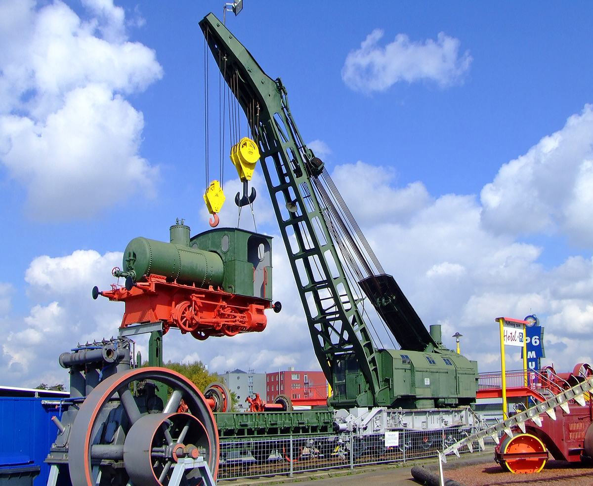 
57t-Ardelt Dampfkran, ex DB 30 80 974 0 035-9, ex DB 6601  Karlsruhe  , ex DB 6600 Mainz, ex DRG 735001 Mainz, am Haken mit angehänter Dampfspeicher Lok O&K 3420/1909 am 18.09.2010 im Auto und Technik Museum Sinsheim.  

Im Jahr 1949 wurden dieser Dampfkran der Firma Ardelt mit 57 Tonnen Traglast in Betrieb genommen. Dies war die maximale Tragkraft, die mit einem 6-achsigen Fahrzeug ohne Überschreitung der mittleren Achslast von 18 t, einer angemessenen Ausladung und einer tragbaren Abstützbreite von 6 Metern ausführbar war. Zudem konnten bei diesem Kranwagen die Gegengewichte am Fahrzeug verbleiben und mussten nicht wie bei seinen schwereren Geschwistern mit 75 und 90 t Tragkraft abgenommen und auf einem separaten Gewichtswagen transportiert werden. Lediglich der das Lichtraummaß überschreitende Schornsteinaufsatz musste abgenommen werden und wurde während der Fahrt hinten über den Gewichten verzurrt. Zur Beförderung über längere Strecken konnte das Gespann in Güterzüge bis zu einer Reisegeschwindigkeit von 80 km/h eingestellt werden. Dennoch konnte man mit 2 dieser 57 Tonnen Kräne auch die schwersten Lokomotiven zurück ins Gleis setzen. Der Kranwagen hat ein Gesamtgewicht von 106 t, um ein Ausschwenken des Auslegers während der Fahrt zu verhindern, wurde ihm als Schutzwagen ein Rungenwagen mit Lagerbock vorangestellt. Die Gesamtlänge des Gespanns über Puffer betrug 22,6 Meter. Bewegt wurde der Dampfkran über eine umsteuerbare liegende Zweizylinder Dampfmaschine mit 75 PS. Je nach Ausladung des Auslegers konnte dieses Fahrzeug sogar unabgestützt noch 23 t in Gleisrichtung heben oder alternativ sogar 15 t rundherum. So ausgerüstet war der Ardelt Dampfkran mit 57 t ein gern und oft gebrauchtes Werkzeug auf Gleisen der DB. Das Einsetzen von Fahrzeugen ins Gleis, Brückenbaustellen und Umladungen waren seine Hauptaufgaben, bei schweren Aufgaben sogar im Zusammenwirken zweier Kraneinheiten. Im Auto-Technik-Museum Sinsheim ist noch der Kran 6601 „Karlsruhe“ (ehem. DRG 735001 Mainz) museal erhalten geblieben. Dieser wurde erst 1979 als letztes Exemplar der Serie ausgemustert.

Gut zu erkennen ist dass der Kran einen zweiten Haken hat, dies ist der Hilfshub. Mit ihm kann er 15 Tonnen bei 15 Metern Ausladung heben.

TECHNISCHE DATEN von dem Kran:
Spurweite: 1.435 mm
Anzahl der Achsen: 6 in 2 Drehgesellen
Baujahr: 1949
Gewicht:  105.720 kg   
Tragkraft:  57 t   
Höchstgeschwindigkeit: 65 km/h  (Teilweise 80 km/h)
Länge über Puffer (Fahrgestell):  10,5 m   
Hubkraft Haupthub: 57 Tonnen bei 7,5 Metern Ausladung (abgestützt)
Hubkraft Hilfshub: 15 Tonnen bei 15 Metern Ausladung (abgestützt)
Ausmusterung: März 1979 als DB 30 80 974 0 035-9 im Bw Ludwigshafen