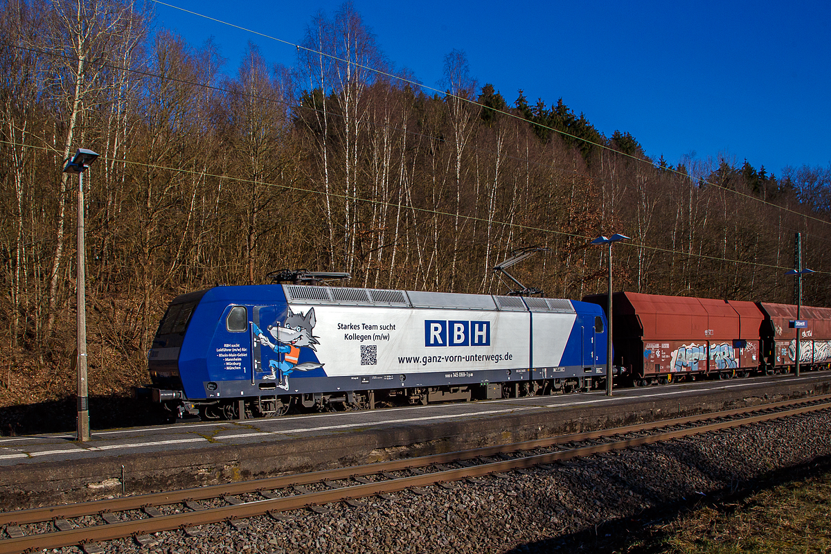 Auch wenn eine Lampenmast etwas stört, noch ein Seitenpotrait....
Die an die RBH Logistics vermietete 145 069-1 (91 80 6145 069-1 D-DB) der DB Cargo AG fährt am 01.03.2021, mit einem Schüttgutwagenzug (leere 4-achsige offene Schüttgutwagen mit schlagartiger Schwerkraftentladung der Gattung Falns 121), durch Dillbrecht an der Dillstrecke (KBS 445) in Richtung Siegen.

Die TRAXX F140 AC wurde 2000 von Adtranz in Kassel unter der Fabriknummer 33396 gebaut und an die DB geliefert, bis 2018 fuhr si für die DB Cargo und wurde dann an die RBH Logistics GmbH in Gladbeck vermietet und dort unter der internen Nummer RBH 228 geführt. 

Die RBH Logistics ist ein Tochterunternehmen der DB Cargo Deutschland AG und die Nachfolgegesellschaft von Werks-, Zechen- und Hafenbahnen im Raum der Bergwerksdirektion Recklinghausen. Durch die verschiedenen Firmenzusammenschlüsse und -aufteilungen ergab sich seit 1913 eine wechselvolle Geschichte. Das heute als Teil des Firmennamens genutzte Akronym RBH stand einige Jahre für die RAG-Bahn- und Hafenbetriebe und wurde beim Verkauf von dieser an die Railion Deutschland im Jahr 2005 beibehalten. Nach damaliger Angabe des neuen Eigentümers stehen die Buchstaben R, B und H nun für die Kernkompetenzen des Unternehmens: Eisenbahnverkehr (Rail), Binnenschifffahrt (Barge) und Hafenumschlag (Harbour).
