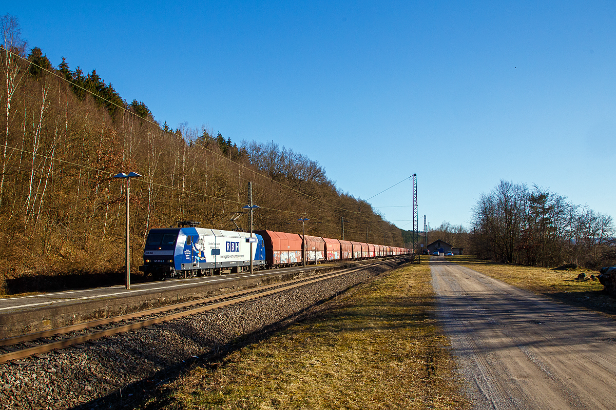 Auch wenn eine Lampenmast etwas stört....
Die an die RBH Logistics vermietete 145 069-1 (91 80 6145 069-1 D-DB) der DB Cargo AG fährt am 01.03.2021, mit einem Schüttgutwagenzug (leere 4-achsige offene Schüttgutwagen mit schlagartiger Schwerkraftentladung der Gattung Falns 121), durch Dillbrecht an der Dillstrecke (KBS 445) in Richtung Siegen.

Die TRAXX F140 AC wurde 2000 von Adtranz in Kassel unter der Fabriknummer 33396 gebaut und an die DB geliefert, bis 2018 fuhr si für die DB Cargo und wurde dann an die RBH Logistics GmbH in Gladbeck vermietet und dort unter der internen Nummer RBH 228 geführt. 

Die RBH Logistics ist ein Tochterunternehmen der DB Cargo Deutschland AG und die Nachfolgegesellschaft von Werks-, Zechen- und Hafenbahnen im Raum der Bergwerksdirektion Recklinghausen. Durch die verschiedenen Firmenzusammenschlüsse und -aufteilungen ergab sich seit 1913 eine wechselvolle Geschichte. Das heute als Teil des Firmennamens genutzte Akronym RBH stand einige Jahre für die RAG-Bahn- und Hafenbetriebe und wurde beim Verkauf von dieser an die Railion Deutschland im Jahr 2005 beibehalten. Nach damaliger Angabe des neuen Eigentümers stehen die Buchstaben R, B und H nun für die Kernkompetenzen des Unternehmens: Eisenbahnverkehr (Rail), Binnenschifffahrt (Barge) und Hafenumschlag (Harbour).