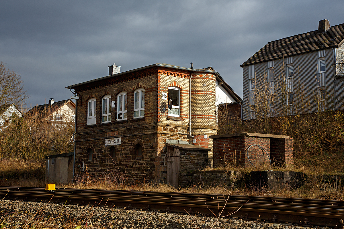 Das 1901 gebaute mechanische Weichenwärter Stellwerk Herdorf Ost (Ho), an der Bahnstrecke Betzdorf - Haiger (KBS 462, auch als Hellertalbahn bezeichnet), hier am 15.02.2022.

Ja, in Herdorf gibt es immer noch den Luxus von zwei in Betrieb befindlichen Stellwerken das Stellwerk Herdorf Fahrdienstleiter (Hf) und das hier zusende Weichenwärter Stellwerk Herdorf Ost (Ho). Sie liegen in Sichtweite ca. 500 m entfernt, Hf beim Bahnhof und hier Ho in der Nähe zum Abzweig zur Anschlussstelle KSW (ex Freien Grunder Eisenbahn). Bis in die 1960-Jahre waren die Aufgaben des Weichenwärters noch sehr umfangreicher. Die Strecke war noch eine zweigleisige Hauptstrecke. Ursprüngliche Planungen sahen sogar vor, sie im Rahmen der Elektrifizierung der Siegstrecke ebenfalls zu elektrifizieren. Diese Erwägungen wurden aber leider nicht weiter verfolgt. Zudem gab es noch Anschlussstellen zur Herdorfer Friedrichs Hütte und zu den Eiserfelder Steinwerken AG.  

Da die Stellwerkstechnik in Herdorf noch rein mechanisch ist, werden beide noch benötigt, bzw. ein Umbau auf ein Stellwerk ist wohl zu aufwendig. 

Im Dezember 2021 wurde bekannt, dass sich einiges an der Hellertalbahn verändern soll. Es sollen vier Halte wegfallen, die übrigen Haltepunkte in Rheinland-Pfälzischem Gebiet erneuert und neue Akkumulatortriebwagen (Akkutriebwagen - AT) eingesetzt werden, die dann auf der Strecke mit bis zu 100 km/h fahren können.  Da bin ich gespannt wann die Veränderung kommt.