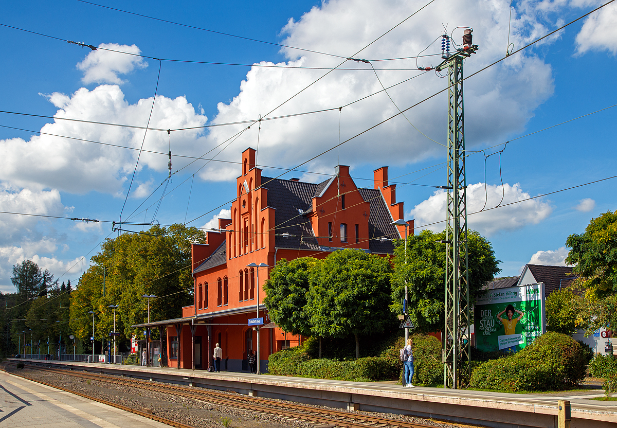 
Das Empfangsgebäude des Bahnhofs Schladern (Sieg) an der Siegstrecke im Ort Windeck-Schladern am 07.09.2020. Das im wilhelminischen Stil 1859 erbaute Ziegelgebäude steht unter Denkmalschutz.

Schlosskopie mit eigener Geschichte
Ohne Bahn kein Fortschritt. Erst mit der Bahnlinie zwischen Köln und Gießen durch das Siegtal konnte die Industrie an der Sieg von der wachsenden Wirtschaft der Industrialisierung profitieren. 1860 erhielt Schladern einen eigenen Bahnhof, der schwierigen Streckenführung durch Berge und über den Fluss zum Trotz. Doch der Aufwand lohnte sich, denn Schladern gehörte Damals zum Kreis Waldbröl und sein Bahnhof war bald Hauptumschlagplatz für Waren aus dem Oberbergischen Land. Der Bahnhof mit seinem repräsentativen Empfangsgebäude erinnert dabei auch an eine Zeit, in der man die reiselustigen Großstädter vom Rhein angemessen willkommen hieß. Mit seinem Baustil und den abgestuften Giebeln war die Ähnlichkeit des Baus mit dem ehemaligen Schloss Windeck durchaus gewollt.

Doch obwohl bereits 1870 mit der Gründung der Bröltaler Eisenbahn (Bröltalbahn) zwischen Hennef (Sieg) und Waldbröl (ab 1891 auch ab Bonn-Beuel) ein Großteil des Warenumschlages auf die neue Schmalspurbahn (Spurweite 785 mm) überging, siedelte sich rund um dem Bahnhof Schladern Industrie an: ein Ziegelwerk, ein Eisenwerk und ein großes Kupferwerk mit eigenem Gleisanschuss (zuletzt als Firma „kabelmetal“ bekannt). Mit dem Rückgang des Güterverkehrs auf der Schiene in den 1990er Jahren und dem Aus für „kabelmetal“  nahm die Bedeutung des Bahnhofs Schladern für den Güterverkehr ab, während es für Pendler (meist in den Großraum Köln) immer wichtiger wurde. Das seit 1989 unter Denkmalschutz stehende Empfangsgebäude wurde aufwendig saniert und restauriert.

Quelle: Am Gebäude angebrachte Tafel