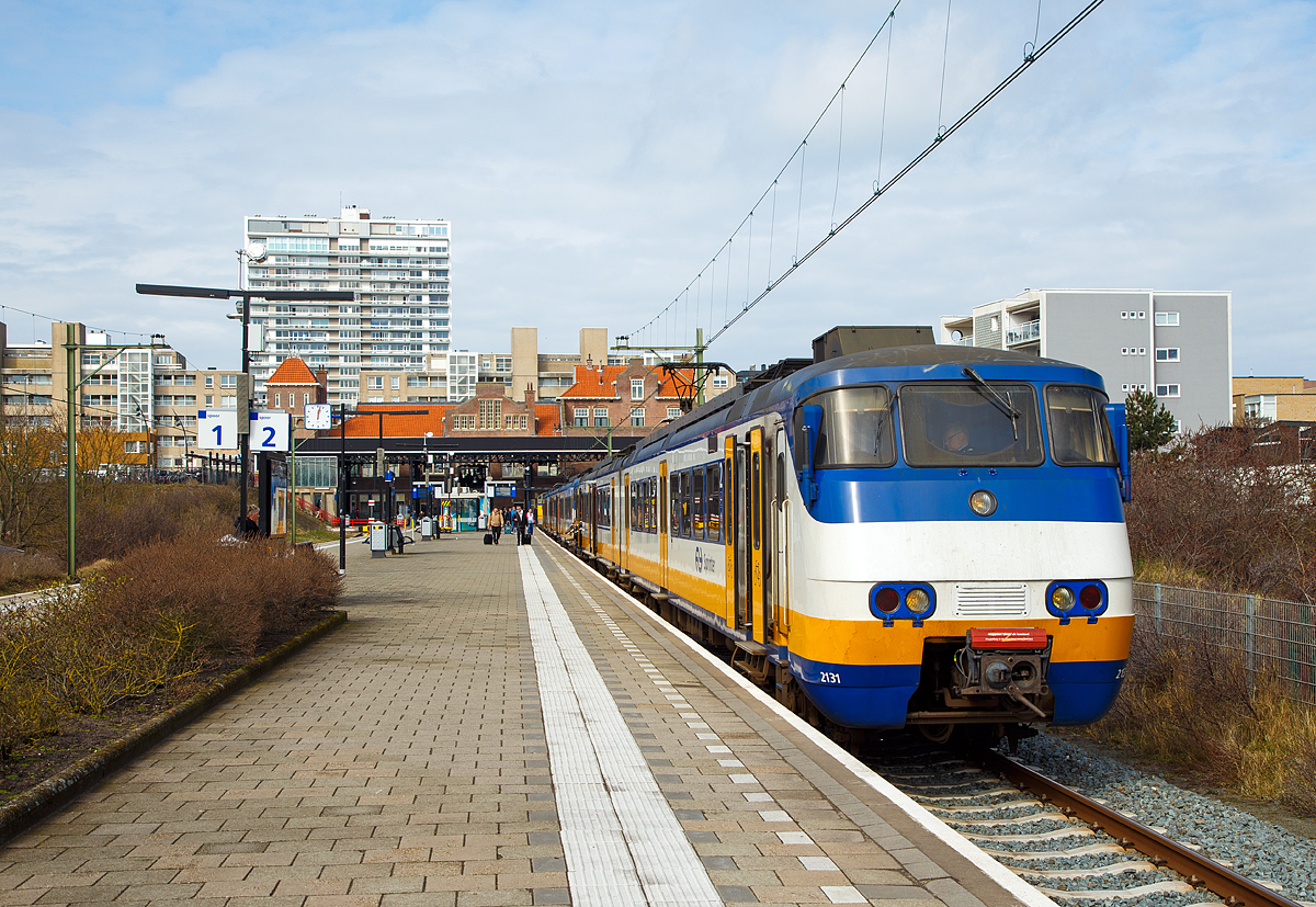 
Der kleine aber sehr schmucke Bahnhof Zandvoort aan Zee von der Gleiseite am 31.03.2018. Der Bahnhof ist ein zweigleisiger Kopfbahnhof. 

Auf Gleis 2 (Spoor 2) steht der Sprinter nach Amsterdam Centraal zur Abfahrt gerade bereit. Der Sprinter besteht aus einem zweitiligen Plan Y (Mat '74) 2131 (Series 2100) gekuppelt mit dem dreiteiligen Plan Y (Mat '74) 2967 (Series 2900). 

Diese 120 km/h schnellen Elektrischen Schnelltriebwagen wurden ab 1975 von der Waggonfabrik Talbot in Aachen für die Nederlandse Spoorwegen (NS) gebaut. 