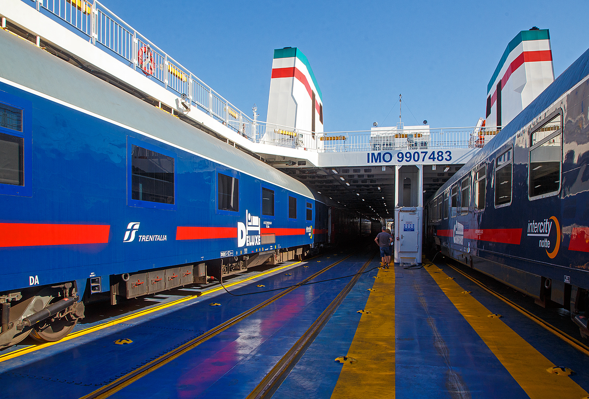 Der Trenitalia InterCity Notte ICN 1962 von Syrakus (Siracusa) nach Milano Centrale, ist am 20.07.2022 in Messina auf die RFI Eisenbahnf�hre Iginia II, verladen. Gleich geht es hin�ber zum Festland nach Villa San Giovanni.

Die Iginia ist eine Ro-Ro-Eisenbahnf�hre des italienischen Eisenbahnnetzes (der Rete Ferroviaria Italiana - RFI), die f�r den Transport von Schienenfahrzeugen, Autos und Passagieren in der Stra�e von Messina bestimmt ist. Sie ist Anfang November 2021 in Messina eingetroffen und wurde am 7. M�rz 2022 im Hafen von Messina in Dienst gestellt. Sie wurde in Genua von der ATI (Baugemeinschaft)T. Mariotti und San Giorgio del Porto gebaut. 

Das Schiff (Nave) erbte ihren Namen von der fr�heren Iginia, auch einer RFI-F�hre in der Stra�e von Messina, die am 1. Oktober 1969 in Dienst gestellt wurde und nach deren letzten Fahrt, zwischen Messina und Villa San Giovanni, am 23. Dezember 2013 endg�ltig ausgemustert wurde.

Die neue Iginia soll CO� neutral sein. Die technischen Eigenschaften sind ebenfalls hochtechnologisch und leistungsf�hig. Das Steuersystem wird durch drei Hauptmotoren und drei Azimut-Triebwerke mit variabler Steigung garantiert, w�hrend zwei Querpropeller maximale Man�vrierf�higkeit erm�glichen. Alle Be- und Entladevorg�nge von Eisenbahnwaggons werden durch die Bugluke �ber die mobile Br�cke durchgef�hrt. Radfahrzeuge hingegen befahren das Ladedeck �ber die Heckluke, �ber die Seitenluke, sowie �ber die Bugluke. 

Die F�hre ist 147 Meter lang und 19 Meter breit und hat eine maximale Kapazit�t von 27 Eisenbahnwaggons auf 4 Gleisen. Sie bietet Platz f�r 700 Personen, einschlie�lich der Besatzung. Maximaler Komfort auch f�r die Innenr�ume, mit einem Hauptsalon mit Barraum mit 339 Sitzpl�tzen, darunter 29 Sitzpl�tze f�r Personen mit eingeschr�nkter Mobilit�t, 7 Rollstuhlpl�tze, 101 Sitzpl�tze im hinteren Salon und 198 im nach au�en offenen Salon.