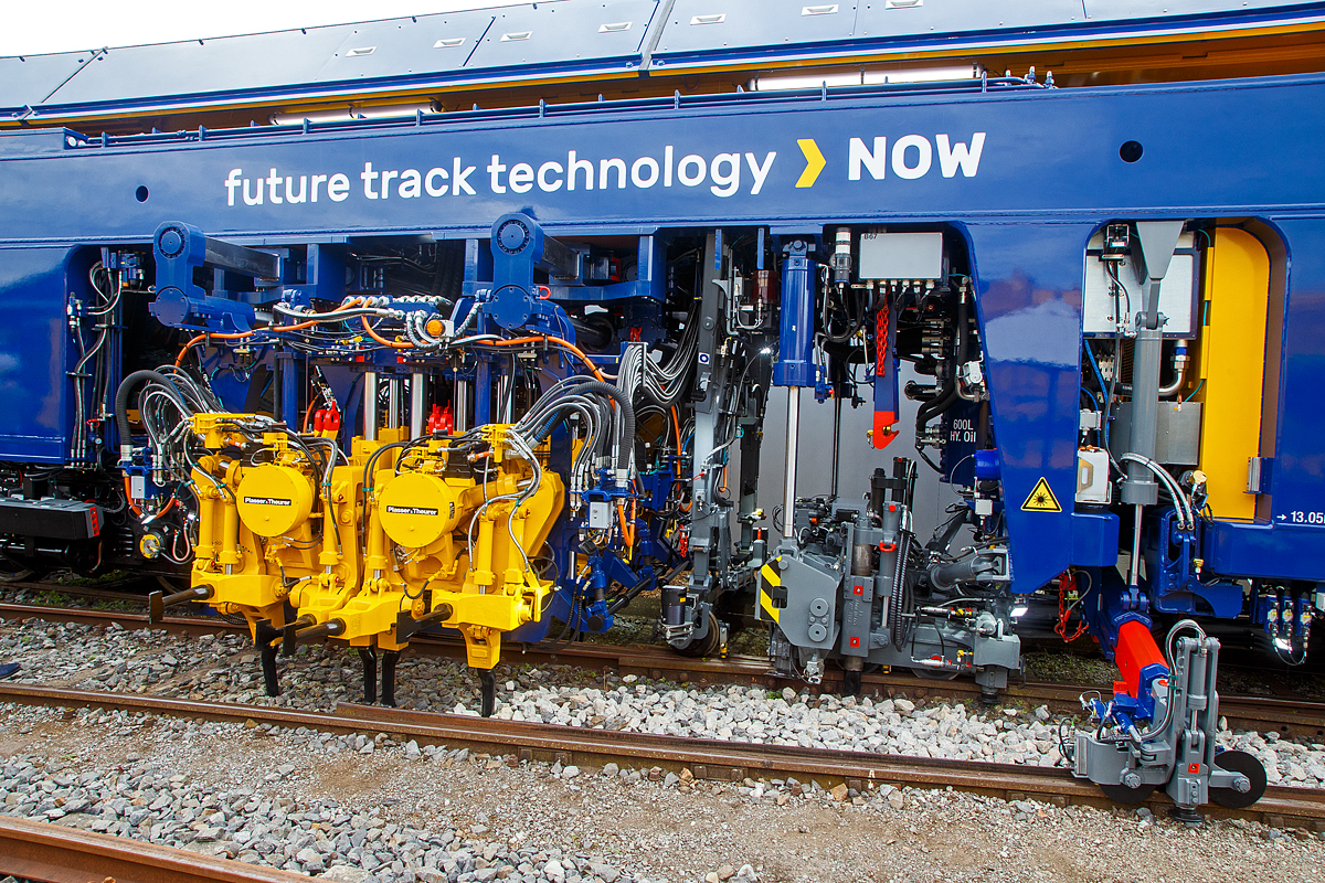 Detailbild der Plasser & Theurer UNIMAT 09-8x4/4S BR Dynamic E³, präsentiert auf der iaf 2022 in Münster (hier am 31.05.2022), eingestellt als A-PLA 99 81 9121 003-3 der Franz Plasser Vermietung von Bahnbaumaschinen. Die fast 69 m lange Maschine ist eine innovative Kombination aus Weichen- und Streckenstopfmaschine mit Planierkapazität und dynamischem Gleisstabilisator.

Rechts (in Arbeitsrichtung vorne) kombinierte Hebe- und Richtaggregat für Gleise und Weichen. Links folgt dann das 8x4 Stopfaggregat ausgestattet mit insgesamt acht unabhängigen Aggregatsegmenten mit je 4 schwenkbaren Stopfpickeln.