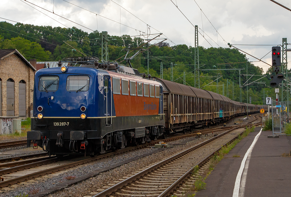 Die 139 287-7 (91 80 6139 287-7 D-BYB) der BayernBahn GmbH f�hrt am 09.06.2020, mit dem sogenannten  Henkelzug  (Langenfeld/Rhld. nach Gunzenhausen), durch Betzdorf (Sieg) in Richtung Siegen. 	

Die Lok wurde 1963 von Krauss-Maffei AG in M�nchen-Allach unter der Fabriknummer 18956 gebaut, der elektrische Teil ist von den Siemens-Schuckert-Werke (SSW) in Berlin. Als DB E10 287 wurde in Dienst gesetzt, mit der Einf�hrung des EDV-Nummernsystems wurde sie zum 01.01.1968 zur DB 110 287–0. Die Lok ist mit Einholmstromabnehmern ausger�stet, sie ist die letzte gebaute Kasten 110er. Zur 139er wurde sie erst 1994 nach einem Umbau, der Lokkasten wurde auf Drehgestelle der Baureihe 140 (E40) gesetzt und es folgte die Umzeichnung in DB 139 287-7. Zum Mai 2009 erfolgte die Z-Stellung bei der DB AG.

Zum 1.Oktober 2011 wurde die Lok durch die BayernBahn GmbH erworben und erhielt anschlie�end eine Untersuchung. Die Neulackierung in kobalt-blau/orange erhielt sie dann 2017.
