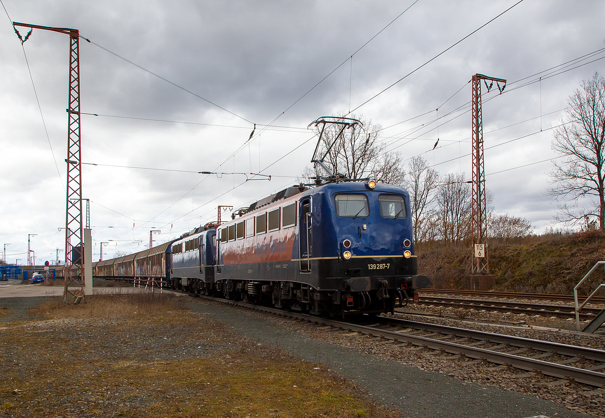 Die 139 287-7 (91 80 6139 287-7 D-BYB) mit der kalten 139 262-0 alias 110 262-3 (91 80 6139 262-0 D-BYB) beide von der BayernBahn GmbH fahren am 12.03.2021 mit dem sogenannten  Henkelzug  (Langenfeld/Rhld. nach Gunzenhausen), durch Rudersdorf (Kr. Siegen) in s�dlicher Richtung bzw. Richtung Dillenburg.

Die 139 287-7:
Vorne die 139 287-7 wurde 1963 von Krauss-Maffei AG in M�nchen-Allach unter der Fabriknummer 18956 gebaut, der elektrische Teil ist von den Siemens-Schuckert-Werke (SSW) in Berlin. Als DB E10 287 wurde in Dienst gesetzt, mit der Einf�hrung des EDV-Nummernsystems wurde sie zum 01.01.1968 zur DB 110 287–0. Die Lok ist mit Einholmstromabnehmern ausger�stet, sie ist die letzte gebaute Kasten 110er. Zur 139er wurde sie erst 1994 nach einem Umbau, der Lokkasten wurde auf Drehgestelle der Baureihe 140 (E40) gesetzt und es folgte die Umzeichnung in DB 139 287-7. Zum Mai 2009 erfolgte die Z-Stellung bei der DB AG. Zum 1.Oktober 2011 wurde die Lok durch die BayernBahn GmbH erworben und erhielt anschlie�end eine Untersuchung. Die Neulackierung in kobalt-blau/orange erhielt sie dann 2017.

Die 139 262-0 alias 110 262-3:
Die 139 262-0 wurde 1962 von Krauss-Maffei AG in M�nchen-Allach unter der Fabriknummer 18921 gebaut, er elektrische Teil ist von den Siemens-Schuckert-Werke (SSW) in Berlin. Als DB E 10 262 wurde in Dienst gesetzt, mit der Einf�hrung des EDV-Nummernsystems wurde sie zum 01.01.1968 zur DB 110 262-3. Auch sie wurde erst 1994, nach dem Erhalt von Drehgestellen der Baureihe 140 (E40) zu einer 139er. Nach dem Umbau wurde sie in DB 139 262-0 umgezeichnet. Ende April 2012 erfolgte die Z-Stellung bei der DB AG und im Mai 2015 wurde sie an die BayernBahn GmbH verkauft und erhielt anschlie�end eine Untersuchung. Die Neulackierung in stahlblau erhielt sie dann 2016.
