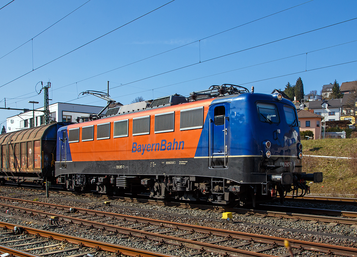 Die 139 287-7 (91 80 6139 287-7 D-BYB) der BayernBahn GmbH fährt am 24.03.2021 mit dem sogenannten  Henkelzug  (Langenfeld/Rhld. nach Gunzenhausen), durch Niederschelden (Sieg) in Richtung Siegen.

Die Lok wurde 1963 von Krauss-Maffei AG in München-Allach unter der Fabriknummer 18956 gebaut, er elektrische Teil ist von den Siemens-Schuckert-Werke (SSW) in Berlin. Als DB E10 287 wurde in Dienst gesetzt, mit der Einführung des EDV-Nummernsystems wurde sie zum 01.01.1968 zur DB 110 287–0. Die Lok ist mit Einholmstromabnehmern ausgerüstet, sie ist die letzte gebaute Kasten 110er. Zur 139er wurde sie erst 1994 nach einem Umbau, der Lokkasten wurde auf Drehgestelle der Baureihe 140 (E40) gesetzt und es folgte die Umzeichnung in DB 139 287-7. Zum Mai 2009 erfolgte die Z-Stellung bei der DB AG.

Zum 1.Oktober 2011 wurde die Lok durch die BayernBahn GmbH erworben und erhielt anschließend eine Untersuchung. Die Neulackierung in kobalt-blau/orange erhielt sie dann 2017.