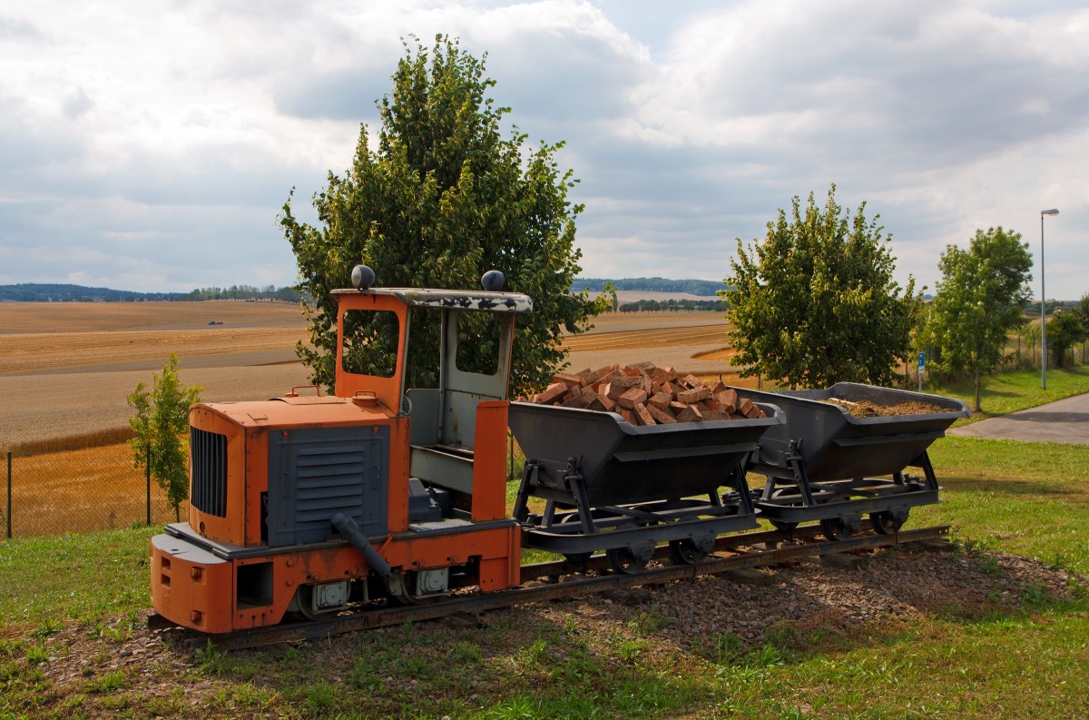 Die 600mm  LKM Ns1b  Diesel-Feldbahnlok, als Denkmallok mit zwei Loren bei Amand Umwelttechnik in Grumbach bei Freital, am 26.08.2013 aufgenommen vom Gehweg aus. 

Die Lok vom Typ Ns 1 b wurde 1960 vom VEB Lokomotivbau Karl Marx Babelsberg (LKM) unter der Fabriknummer 260103 gebaut und an den VEB Ziegelwerk in Grumbach geliefert. 

Diese kleinste Lok des LKM-Typenprogramms entspricht in Aufbau, Größe und Leistung der Jung-Lok EL 105, sogar das Getriebe beider Loks ist austauschbar. Mit ihrem geringen Gewicht und dem kurzen Achsstand war sie auch auf Gleisanlagen mit kleinem Schienenprofil und schwachem Unterbau zu fahren. Der ursprüngliche stehende Einzylindermotor wurde später (wie bei vielen Ns 1 b) durch einen Vierzylinder-V-Motor ersetzt, was Improvisationen an der Auspuffanlage erforderlich machte: An beiden Seiten der Motorverkleidung wurden die Bleche aufgeschnitten und Auspuffrohre mit Schalldämpfern durchgeführt.

Technische Daten:
Hersteller:  LKM
Fabriknummer:  247418
Baujahr:  1957
Spurweite: 600 mm (Lieferbar war 485 mm ဓ 600 mm)
Bauart:  B-dm
Leistung:  15 PS Nenndrehzahl:  1500/min
Dienstgewicht:  2,8 t
Länge über Puffer:  2.320 mm
Breite:  1.020 mm
Höhe:  2.355 mm (mit Führerhaus)
Achsstand:  720 mm
Zugkraft:  500 kg
Geschwindigkeit:  8 km/h
Kleinster bef. Halbmesser:  7,5 m
Treibraddurchmesser:  376 mm
Leistungsübertragung:  mechanisch, Kette
Übersetzungsstufen:  2
Bremse:  Handhebelbremse
Kupplungstyp:  Ketten-Kupplung

Obwohl von der Type NS 1 ca. 700 Stück gebaut wurden, hat ihre Zahl nach der deutschen Einheit erheblich abgenommen. Während die Stillegung von Feldbahnen in der BRD seit den 60er Jahren allmählich verlief, vollzog sich dieser Prozess in den neuen Bundesländern durch Werksschließungen oder Umstellung der Förderung auf LKW oder Bandförderung innerhalb weniger Jahre. 