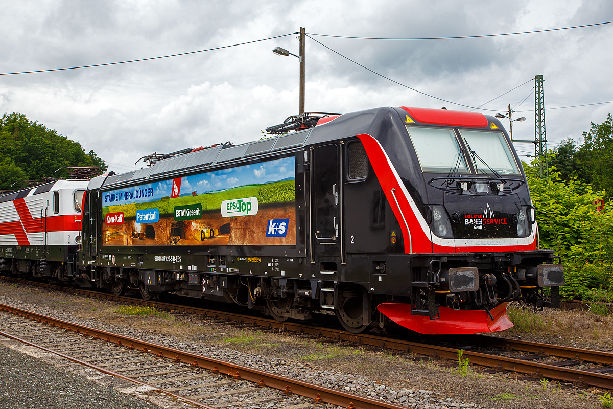 Die Bombardier TRAXX F160 AC3 LM, 187 420-5 (91 80 6187 420-5 D-EBS) der EBS - Erfurter Bahnservice GmbH steht am 05.07.2021 in Scheuerfeld (Sieg) beim Kleinbahnhof der WEBA (Westerwaldbahn), f�r ihre n�chste Aufgabe der Abfuhr von schweren Holzz�gen, bereit.

Die Bombardier TRAXX F160 AC3 LMD wurde 2019 von Bombardier in Kassel unter der Fabriknummer 35595 gebaut. Nach meiner Sichtung hat die Lok die Zulassung f�r Deutschland (D) und �sterreich (A). F�r Ungarn und Rum�nien sind die Zulassungen noch nicht erteilt (H und RO sind durchgestrichen).

Wie die Vorg�ngerinnen AC1 und AC2 ist die AC3 f�r den Betrieb unter 15 Kilovolt bei 16,7 Hertz, sowie unter 25 Kilovolt bei 50 Hertz Wechselstrom ausgelegt, und verf�gt unver�ndert �ber eine Dauerleistung von 5.600 kW und eine Anfahrzugkraft von 300 kN. Von den Traxx 2E �bernommen wurde der Maschinenraum mit Seitengang um das sogenannte Powerpack, bestehend aus Stromrichter und Hochspannungsger�st, womit erstmals alle Varianten dasselbe Layout verwenden.

Neu ist die Kopfform der Traxx-3-Lokomotiven, im Wesentlichen ein auf dem Lokkasten aufgesetztes GFK-Modul. Zudem wurden die Lokomotiven erstmals ab Werk konstruktiv f�r den Einbau der Zugbeeinflussung ETCS vorbereitet. Neuerungen betreffen die verf�gbaren Drehgestelle: zu den bisherigen Varianten „F140“ mit Tatzlagerantrieb und Zulassung f�r maximal 140 km/h, und „P160“ mit Hohlwellenantrieb und Zulassung f�r maximal 160 km/h, werden die Traxx-3-Lokomotiven offiziell auch als Variante „F160“ mit Tatzlagerantrieb und Zulassung f�r maximal 160 km/h angeboten.

G�nzlich neu sind die optional verf�gbaren Last-Mile-Module, die es als Last-Mile-Diesel (LMD) mit zus�tzlicher Last-Mile-Battery (LMB) gibt. Das LMD besteht aus einem Dieselhilfsmotor und einem Kraftstofftank, um auch nicht-elektrifizierte Streckenabschnitte und Anschlussgleise befahren zu k�nnen. Der Dieselmotor von Deutz verf�gt �ber einen Hubraum von 7.150 cm�, erbringt eine Leistung von 230 kW (180 kW am Rad), mit Batterieunterst�tzung 290 kW und erf�llt die Stage-IIIB-Abgasnorm. Im Dieselbetrieb werden alle vier Fahrmotoren betrieben, die Anfahrzugkraft betr�gt dabei mit Batterieunterst�tzung unver�ndert 300 kN, ohne Batterie 260 kN. Ohne Anh�ngelast ist damit eine H�chstgeschwindigkeit von 60 km/h m�glich, bei 2000 Tonnen Last noch 40 km/h. Der Tankinhalt von 400 Litern reicht f�r bis zu acht Stunden Dieselbetrieb, kurze Strecken k�nnen auch ausschlie�lich mit der eingebauten Batterie zur�ckgelegt werden. Der �bergang vom elektrischen zum Dieselbetrieb kann w�hrend der Fahrt erfolgen. F�r den Rangierbetrieb ist zudem eine Funkfernsteuerung erh�ltlich.

Erstmals wurde der Lokkasten nicht mit glatten Seitenw�nden gefertigt, sondern konstruktiv deutlich g�nstiger, sind die Seitenw�nde der AC3 vertikal gesickt und die Seitenfl�chen erhielten sogenannte Flex-Panels, eine Vorrichtung zum Einspannen von Planen. Diese w�rden die Sicken verdecken, und w�ren kosteng�nstiger als Umlackierungen oder Umbeklebungen. Die Nutzung der Flex-Panels wurde jedoch in der Schweiz umgehend untersagt.

TECHNISHE DATEN:
Hersteller:  Bombardier Transportation
Spurweite:  1.435 mm (Normalspur)
Achsanordnung: Bo’ Bo’
L�nge �ber Puffer: 18.900 mm
Drehzapfenabstand: 10.440 mm
Achsabstand im Drehgestell: 2.600 mm
Treibraddurchmesser:  1.250 mm (neu) / 1.170 mm (abgenutzt)
H�he:  4.283 mm
Breite:  2.977 mm
Lichtraumprofil: UIC 505-1
Dienstgewicht:  87 t
Fahrmotoren: 4 Asynchronmotoren
Bremse: Elektrische Bremse (SW-GPR-E mZ)

Daten im Oberleitungsbetrieb:
H�chstgeschwindigkeit: 160 km/h
Dauerleistung: 5.600 kW 
Kurzzeitleistung  Power Boost : 6.000 kW
Anfahrzugkraft: 300 kN
Dauerzugkraft: 252 kN bei 80 km/h
Stromsystem:  15 kV 16,7 Hz~ und 25 kV 50 Hz~

Daten im Dieselbetrieb (Last-Mile):
Nenndrehzahl: 1.800 U/min
H�chstgeschwindigkeit:  60 km/h
Dauerleistung: 230 kW (180 kW am Rad),
Tankinhalt:  400 l