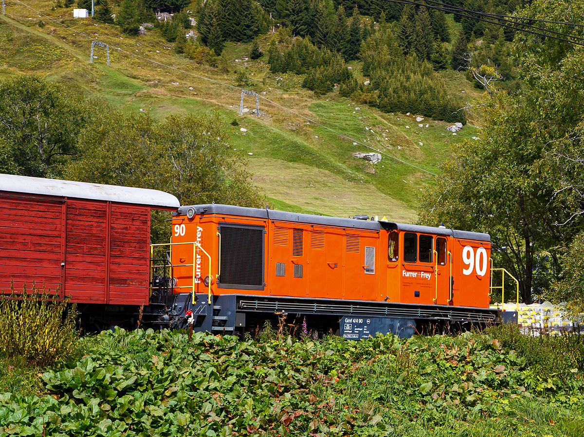 Die Die Furrer + Frey Gmf 4/4 90 abgestellt am 07.09.2021 beim DFB Bahnhof Realp  (1.538 m ü. M.). 

Eine ehemalige modernisierte und umgespurte rumänische FAUR L 45 H (Baujahr 1969 unter Fabriknummer 20867 in Spurweite 760 mm), die ex CFR 87-0023-9 (C.F.R. steht für Căile Ferate Române der staatlichen Eisenbahngesellschaft Rumäniens.

Weil es etwas länger ist fange ich mit der Zusammenfassung und den Technischen Daten an, wer es ausführlich mag kann sehr gerne weiterlesen.

Zusammenfassung:
Der Fahrleitungsbauer Furrer + Frey in Bern hat im Oktober 2014 eine vierachsige Diesellokomotive aus Rumänien mit rund 500 kW Leistung an der Welle nach Umbau und Hauptrevision erfolgreich in Betrieb genommen. Die Arbeiten hatte das Werk Krieglach der Tecsol GmbH in der Steiermark in weniger als zehn Monaten ausgeführt. Dabei wurde die Lokomotive von bosnischer Spur (760 mm) auf Meterspur umgebaut und mit einem modernen Dieselmotor ausgerüstet. Nach erfolgreicher dynamischer Inbetriebsetzung bei der MGB ist die Gmf 4/4 90 seit Mitte
Oktober 2014 für Einsätze auf den meterspurigen  Adhäsions-Bahnnetzen in der Schweiz bereit.

TECHNISCHE DATEN der Adhäsions-Diesellokomotive Gmf 4/4 90
Spurweite:  1.000 mm
Achsanordnung:  B’ B’ (4 Triebachsen)
Länge über Puffer:12.000 mm
Breite über Rahmen: 2.440 mm
Breite über Kasten: 2.200 mm
Höhe: 3.320 mm
Drehzapfenabstand: 5.500 mm
Achsabstand im Drehgestell :1.700 mm
Raddurchmesser:  750mm (neu) / 710 mm (abgenutzt)
Dienstgewicht: 40 t
Maximale Radsatzlast: 10 t
Antrieb: dieselhydraulisch
Leistung Hauptdieselmotor:  520 kW bei 2100 U/min, gedrosselt auf 490 kW bei 1800 U/min 
Leistung Hilfsdieselmotor: 50 kW bei 1500 U/min
Anfahrzugkraft bis 10 km/h:  90 kN
Höchstgeschwindigkeit: Schnellgang 50 km/h / Rangiergang 22 km/h (55 km/h geschleppt)
Kleinster befahrbarer Kurvenradius: 45 m
Kraftstoffvorrat: 970 Liter
Anhängelasten: bis 70 ‰ mit bis 50 t bei 10 km/h

Seit mehr fast Jahren projektiert und baut die in Bern ansässige Firma Furrer + Frey AG Fahrleitungen für normal- und schmalspurige Eisenbahnen, Bergbahnen, Trambahnen und Trolleybusse im In- und Ausland. 2013 standen für die kommenden Jahre bei mehreren Tunnelgewerken schweizerischer Meterspurbahnen Sanierungen und Arbeiten zur Erhöhung der Sicherheit an, die generell einen größeren Bedarf an meterspurigen thermischen Diensttriebfahrzeugen auslösten. In diesem Hinblick auf die damit anstehenden Erneuerungen und Neubauten von Fahrleitungen hatte sich F+F deshalb im Herbst 2013 entschieden, eine leistungsfähigere thermische Lokomotive Gmf 4/4 zu beschaffen. Umfangreiche Marktabklärungen zeigten, dass im gewünschten Zeitraum von weniger als einem Jahr einzig die Beschaffung einer gebrauchten und entsprechend den Bedürfnissen von F+F um zu bauenden Maschine kostengünstig und erfolgreich umzusetzen war.

Im Herbst 201 3 konnte die TecSol GmbH in Anger (Steiermark) kurzfristig eine vierachsige Umbau-Diesellokomotive rumänischer Herkunft anbieten, die die geforderten Eckwerte erfüllte. Die aus dem Jahr 1969 stammende Lokomotive vom Typ  Faur L45H mit der Fabriknummer 20867 ist eine von insgesamt 334 Exemplaren, die FAUR in Bukarest hergestellt hatte. Sie wurde 2014 in Krieglach (Steiermark) hauptrevidiert, remotorisiert und von bosnischer Spurweite (760 mm) auf Meterspur umgebaut. 

Von der ursprünglichen Lokomotive wurden der Rahmen, die Vorbauten, das Mittelführerhaus, das Verteilgetriebe und die beiden kardanisch angetriebenen Drehgestelle beibehalten. Die übrigen Komponenten, wie Dieselmotor mit Partikelfilter und Generatoren, Kühlanlage inklusive Kühlerventilator, 01- und Wasserpumpen, Hilfsdieselmotor, Generator-Gruppe mit Partikelfilter, Dieselölbehälter, Bordnetzumrichter, Kompressor, Vakuumpumpe, Druckluftgerüst, Magnetschienenbremsen und die Fahrzeugleittechnik, wurden neu eingebaut.

Mechanischer Teil:
Das Untergestell ist eine Schweißkonstruktion aus Walzprofilen, Blechen und Abkantprofilen. Der Rahmen wird gebildet aus je zwei äußeren und inneren Längsträgern, zwei Hauptquerträgern, mehreren diagonal und quer angeordneten Verstärkungsträgern sowie zwei kastenförmig angebauten Endplattform-Vorbauten. Er wurde verstärkt und auf eine Längsdruckfestigkeit von 800 kN ausgelegt. Auf dem Rahmen aufgebaut ist das Mittelführerhaus, an das am Ende I ein langer Vorbau und am Ende II ein kurzer Aufbau angrenzt. 

Für Einsätze bei verschiedenen Meterspurbahnen können die modular auf angeschraubten Adapter-Wechselplatten montierten schweizerischen Zug- und Stoßvorrichtungen: 
•	Zp1 , 500/750 mm über Schienenoberkante (SOK), für Einsatz unter anderem bei der Montreux - Berner Oberland-Bahn (MOB);
•	Zp2, 620 mm über SOK, für Einsatz unter anderem bei der Matterhorn – Gotthard Bahn (MGB) und bei der Rhatischen Bahn (RhB);
•	GFN  hoch , 620/650 mm über SO K, für Einsatz unter anderem bei der Biere - Apples -Morges-Bahn (MBC-BAM), bei den Berner Oberland-Bahnen (BOB), bei der MGB
•	GFN  tief , 500 mm über SOK, für Einsatz unter anderem beim Regionalverkehr Bern - Solothurn (RBS) und bei Aare - Seelandmobil (ASm).
auf einfache Weise mit Hilfe eines Krans oder Gabelstaplers gewechselt werden.

Das Drehmoment des Dieselmotors wird über ein im Rahmen gelagertes hydraulisches Turbogetriebe (Fahrtrichtungswahl und verschleißfreie Bremse) mit darunter angebautem Nachschaltgetriebe (Auswahl für Strecken-/Rangiergang) pro Drehgestell über eine Kardanwelle auf die unter sich in den Drehgestellen ebenfalls kardanisch gekuppelten Radsätze übertragen. Das Turbogetriebe lässt dank den pro Fahrtrichtung getrennten Wandlern verschleißfreie Bremsungen zu, womit das Befahren starker Gefälle möglich ist (Steilstreckenfähigkeit).Jedes Drehgestell verfügt über zwei Bremszylinder, die auf die je einseitig pro Rad angeordnete Bremsklötze wirken. Als Feststellbremse wirkt pro Drehgestell je ein Federspeicher-Bremszylinder.

Thermischer Teil:
Die Lokomotive ist mit einem im Rahmen gelagerten sechszylindrigen Hauptdieselmotor Caterpillar C18 mit rund 500 kW Leistung an der Welle und einer Dieselpartikelfilteranlage ausgerüstet. Weiter ist ein Hilfsdieselmotor-Generator-Aggregat mit einer Leistung von 50 kVA mit Partikelfilter installiert. Damit wird die Energieversorgung 3 x 400 V auch bei abgestelltem Hauptdieselmotor gewährleistet, was bei Arbeitseinsätzen in Talrichtung markante Treibstoff-Einsparungen ermöglicht. Die Lokomotive entspricht den in der Schweiz geltenden Vorschriften für den Gesundheitsschutz auf Untertagebaustellen. Dadurch sind die Voraussetzungen für Einsätze dieser Lokomotive auch bei Arbeiten in allen Bahntunneln gegeben.

Elektrischer Teil:
Die Lokomotive verfügt über ein Steuerstromnetz 24 V DC und eine zusätzliche 12-V-Batterie für den Hilfsdieselmotor. Zudem erzeugt ein DC/DC-Wandler aus dem 24-V-Netz 110 V für die Steuerung des Kompressors. Vom Hauptdieselmotor über Keilriemen angetriebene zwei kleinere Generatoren erzeugen das Bordnetz 3 x 400 V AC. Über je einen eigenen Frequenzumrichter werden der Kompressor, die Vakuumpumpe und der Kühlerventilator frequenzvariabel betrieben. Die beiden Zusatzöl- und Zusatzkühlwasserpumpen für den hydraulischen Bremsbetrieb, die Kühlwasservorheizung des Hauptdieselmotors, die Zusatzheizung für den Führerraum sowie die beiden Umwälzpumpen für die Kühlwasservorwärmung des Hauptdieselmotors und die Umwälzpumpe für die Führerraumheizung werden mit konstanter Frequenz von 50 Hz ab dem Bordnetz versorgt. Alternativ wird das Bordnetz über die Fremdeinspeisungsstecker ortsfest gespeist. Die 24-V-Batterieladung erfolgt von der Lichtmaschine des Hauptdieselmotors. Möglich ist aber auch von der Sammelschiene 3 x 400 V über einen Transformator 400 V / 230 V oder über die einphasige Fremdeinspeisung mit 230 V AC. Die 12-V-Batterieladung erfolgt von der Lichtmaschine des Hilfsdieselmotors oder über die 230-V-Fremdeinspeisung. Da der Hilfsdieselmotor mit 12 V angelassen wird, könnte die Lokomotive bei leeren Batterien auch mit einem Überbrückungskabel von jedem Auto aus wieder gestartet werden.

Stirnseitig ist an beiden Vorbauten je eine Kamera zur besseren Beobachtung des Fahrweges mit Bildübertragung auf einen Monitor pro Führerpult installiert. Die eingebaute Funkfernsteuerung  LocControl 100  erlaubt dem Lokomotivführer die Bedienung auch außerhalb des Führerstandes. Zwei gelbe Leuchten auf dem Dach zeigen den aktiven Funkfernsteuerbetrieb an. Vor Beginn einer Bewegung geben Rückfahrwarner beidseitig in der Gleisachse drei kurze Töne zur Warnung von Personen im Gleisfeld ab. Blaue Leuchten auf dem Dach zeigen zudem Störungen oder zwingend erforderliche Handlungen des Lokomotivführers vor der Weiterfahrt an.

Pneumatischer Teil und Bremsen:
Die Lokomotive ist grundsätzlich druckluftgebremst, sie kann sowohl mit Vakuum als auch mit Druckluft gebremste Anhängelasten mitführen. Die Druckluftbremse der Lokomotive wirkt über ein Pilotventil auch vakuumgesteuert als automatische Bremse von der Vakuum-Hauptleitung her. Die Lokomotive verfügt über Klotzbremsen mit zwei Bremszylindern pro Drehgestell und je einer Samson-Bremssohle mit 3 % Phosphorgehalt pro Rad. Diese werden über die automatische Druckluftbremse (wahlweise mit 5 oder 4 bar Regeldruck), über die elektrisch gesteuerte direkte Bremse (Rangierbremse), über die Vakuumbremse mit einem Regeldruck von - 52 cm Hg oder über die Federspeicher-Feststellbremse zur Wirkung gebracht. Als Feststellbremse sind zwei Federspeicherzylinder in den beiden Vorbauten integriert. Pro Drehgestell ist ein Steuerventil zur automatischen Druckluftbremse vorhanden. Zusätzlich bremst eine verschleißfreie hydraulische Retarderbremse das Fahrzeug und ermöglicht seine Steilstreckenfähigkeit. Die Ausführungsbestimmungen zur schweizerischen Eisenbahnverordnung verlangen beim Befahren von Strecken mit unabhängigem Bahnkörper und mehr als 60‰ Neigung (unter anderem MOB, Berninabahn der RhB) eine Sicherheitsbremse, die von der Reibung zwischen Rad und Schiene unabhängig ist. Zur Erfüllung dieser Forderung dient eine Magnetschienenbremse.

Inbetriebnahme:
Im Herbst 2014 folgten zwei sehr intensive Wochen mit dynamischen Inbetriebsetzungsfahrten auf dem Netz der MGB zwischen Ackersand , Visp, Brig und Grengiols, sowie am Nätschen unterhalb der 2.033 Meter hohen Station Oberalppass. Dabei konnten die einwandfreie Funktion der Lokomotive festgestellt und die nötigen Feineinstellungen vorgenommen werden. Bremswegmessungen und Lastfahrten mit 50 t Anhängelast auf den bis zu 70 ‰ steilen Abschnitten der MGB wurden Anfang Oktober ebenfalls erfolgreich absolviert. Am 10. Oktober 2014 kontrollierte das Bundesamt für Verkehr (BAV) die Lokomotive im Rahmen der technisch-betrieblichen Sicherheitsprüfung zwischen Brig und Ackersand. Wenige Tage nach der erfolgreichen Abnahme durch das BAV und nach zwei Tagen Triebfahrzeugführerschulung ging die Lokomotive in Einsatz.

Quelle: Furrer + Frey (mit Eisenbahn-Revue 12/2014)
 Gmf 4/4 90 abgestellt am 07.09.2021 beim DFB Bahnhof Realp  (1.538 m ü. M.). 

Eine ehemalige modernisierte und umgespurte rumänische FAUR L 45 H (Baujahr 1969 unter Fabriknummer 20867 in Spurweite 760 mm), die ex CFR 87-0023-9 (C.F.R. steht für Căile Ferate Române der staatlichen Eisenbahngesellschaft Rumäniens.

Weil es etwas länger ist fange Zusammenfassung und den Technischen Daten an, wer es ausführlich mag kann sehr gerne weiterlesen.

Zusammenfassung:
Der Fahrleitungsbauer Furrer + Frey in Bern hat im Oktober 2014 eine vierachsige Diesellokomotive aus Rumänien mit rund 500 kW Leistung an der Welle nach Umbau und Hauptrevision erfolgreich in Betrieb genommen. Die Arbeiten hatte das Werk Krieglach der Tecsol GmbH in der Steiermark in weniger als zehn Monaten ausgeführt. Dabei wurde die Lokomotive von bosnischer Spur (760 mm) auf Meterspur umgebaut und mit einem modernen Dieselmotor ausgerüstet. Nach erfolgreicher dynamischer Inbetriebsetzung bei der MGB ist die Gmf 4/4 90 seit Mitte
Oktober 2014 für Einsätze auf den meterspurigen  Adhäsions-Bahnnetzen in der Schweiz bereit.

TECHNISCHE DATEN der Adhäsions-Diesellokomotive Gmf 4/4 90
Spurweite:  1.000 mm
Achsanordnung:  B’ B’ (4 Triebachsen)
Länge über Puffer:12.000 mm
Breite über Rahmen: 2.440 mm
Breite über Kasten: 2.200 mm
Höhe: 3.320 mm
Drehzapfenabstand: 5.500 mm
Achsabstand im Drehgestell :1.700 mm
Raddurchmesser:  750mm (neu) / 710 mm (abgenutzt)
Dienstgewicht: 40 t
Maximale Radsatzlast: 10 t
Antrieb: dieselhydraulisch
Leistung Hauptdieselmotor:  520 kW bei 2100 U/min, gedrosselt auf 490 kW bei 1800 U/min 
Leistung Hilfsdieselmotor: 50 kW bei 1500 U/min
Anfahrzugkraft bis 10 km/h:  90 kN
Höchstgeschwindigkeit: Schnellgang 50 km/h / Rangiergang 22 km/h (55 km/h geschleppt)
Kleinster befahrbarer Kurvenradius: 45 m
Kraftstoffvorrat: 970 Liter
Anhängelasten: bis 70 ‰ mit bis 50 t bei 10 km/h

Seit mehr fast Jahren projektiert und baut die in Bern ansässige Firma Furrer + Frey AG Fahrleitungen für normal- und schmalspurige Eisenbahnen, Bergbahnen, Trambahnen und Trolleybusse im In- und Ausland. 2013 standen für die kommenden Jahre bei mehreren Tunnelgewerken schweizerischer Meterspurbahnen Sanierungen und Arbeiten zur Erhöhung der Sicherheit an, die generell einen größeren Bedarf an meterspurigen thermischen Diensttriebfahrzeugen auslösten. In diesem Hinblick auf die damit anstehenden Erneuerungen und Neubauten von Fahrleitungen hatte sich F+F deshalb im Herbst 2013 entschieden, eine leistungsfähigere thermische Lokomotive Gmf 4/4 zu beschaffen. Umfangreiche Marktabklärungen zeigten, dass im gewünschten Zeitraum von weniger als einem Jahr einzig die Beschaffung einer gebrauchten und entsprechend den Bedürfnissen von F+F um zu bauenden Maschine kostengünstig und erfolgreich umzusetzen war.

Im Herbst 201 3 konnte die TecSol GmbH in Anger (Steiermark) kurzfristig eine vierachsige Umbau-Diesellokomotive rumänischer Herkunft anbieten, die die geforderten Eckwerte erfüllte. Die aus dem Jahr 1969 stammende Lokomotive vom Typ  Faur L45H mit der Fabriknummer 20867 ist eine von insgesamt 334 Exemplaren, die FAUR in Bukarest hergestellt hatte. Sie wurde 2014 in Krieglach (Steiermark) hauptrevidiert, remotorisiert und von bosnischer Spurweite (760 mm) auf Meterspur umgebaut. 

Von der ursprünglichen Lokomotive wurden der Rahmen, die Vorbauten, das Mittelführerhaus, das Verteilgetriebe und die beiden kardanisch angetriebenen Drehgestelle beibehalten. Die übrigen Komponenten, wie Dieselmotor mit Partikelfilter und Generatoren, Kühlanlage inklusive Kühlerventilator, 01- und Wasserpumpen, Hilfsdieselmotor, Generator-Gruppe mit Partikelfilter, Dieselölbehälter, Bordnetzumrichter, Kompressor, Vakuumpumpe, Druckluftgerüst, Magnetschienenbremsen und die Fahrzeugleittechnik, wurden neu eingebaut.

Mechanischer Teil:
Das Untergestell ist eine Schweißkonstruktion aus Walzprofilen, Blechen und Abkantprofilen. Der Rahmen wird gebildet aus je zwei äußeren und inneren Längsträgern, zwei Hauptquerträgern, mehreren diagonal und quer angeordneten Verstärkungsträgern sowie zwei kastenförmig angebauten Endplattform-Vorbauten. Er wurde verstärkt und auf eine Längsdruckfestigkeit von 800 kN ausgelegt. Auf dem Rahmen aufgebaut ist das Mittelführerhaus, an das am Ende I ein langer Vorbau und am Ende II ein kurzer Aufbau angrenzt. 

Für Einsätze bei verschiedenen Meterspurbahnen können die modular auf angeschraubten Adapter-Wechselplatten montierten schweizerischen Zug- und Stoßvorrichtungen: 
•	Zp1 , 500/750 mm über Schienenoberkante (SOK), für Einsatz unter anderem bei der Montreux - Berner Oberland-Bahn (MOB);
•	Zp2, 620 mm über SOK, für Einsatz unter anderem bei der Matterhorn – Gotthard Bahn (MGB) und bei der Rhatischen Bahn (RhB);
•	GFN  hoch , 620/650 mm über SO K, für Einsatz unter anderem bei der Biere - Apples -Morges-Bahn (MBC-BAM), bei den Berner Oberland-Bahnen (BOB), bei der MGB
•	GFN  tief , 500 mm über SOK, für Einsatz unter anderem beim Regionalverkehr Bern - Solothurn (RBS) und bei Aare - Seelandmobil (ASm).
auf einfache Weise mit Hilfe eines Krans oder Gabelstaplers gewechselt werden.

Das Drehmoment des Dieselmotors wird über ein im Rahmen gelagertes hydraulisches Turbogetriebe (Fahrtrichtungswahl und verschleißfreie Bremse) mit darunter angebautem Nachschaltgetriebe (Auswahl für Strecken-/Rangiergang) pro Drehgestell über eine Kardanwelle auf die unter sich in den Drehgestellen ebenfalls kardanisch gekuppelten Radsätze übertragen. Das Turbogetriebe lässt dank den pro Fahrtrichtung getrennten Wandlern verschleißfreie Bremsungen zu, womit das Befahren starker Gefälle möglich ist (Steilstreckenfähigkeit).Jedes Drehgestell verfügt über zwei Bremszylinder, die auf die je einseitig pro Rad angeordnete Bremsklötze wirken. Als Feststellbremse wirkt pro Drehgestell je ein Federspeicher-Bremszylinder.

Thermischer Teil:
Die Lokomotive ist mit einem im Rahmen gelagerten sechszylindrigen Hauptdieselmotor Caterpillar C18 mit rund 500 kW Leistung an der Welle und einer Dieselpartikelfilteranlage ausgerüstet. Weiter ist ein Hilfsdieselmotor-Generator-Aggregat mit einer Leistung von 50 kVA mit Partikelfilter installiert. Damit wird die Energieversorgung 3 x 400 V auch bei abgestelltem Hauptdieselmotor gewährleistet, was bei Arbeitseinsätzen in Talrichtung markante Treibstoff-Einsparungen ermöglicht. Die Lokomotive entspricht den in der Schweiz geltenden Vorschriften für den Gesundheitsschutz auf Untertagebaustellen. Dadurch sind die Voraussetzungen für Einsätze dieser Lokomotive auch bei Arbeiten in allen Bahntunneln gegeben.

Elektrischer Teil:
Die Lokomotive verfügt über ein Steuerstromnetz 24 V DC und eine zusätzliche 12-V-Batterie für den Hilfsdieselmotor. Zudem erzeugt ein DC/DC-Wandler aus dem 24-V-Netz 110 V für die Steuerung des Kompressors. Vom Hauptdieselmotor über Keilriemen angetriebene zwei kleinere Generatoren erzeugen das Bordnetz 3 x 400 V AC. Über je einen eigenen Frequenzumrichter werden der Kompressor, die Vakuumpumpe und der Kühlerventilator frequenzvariabel betrieben. Die beiden Zusatzöl- und Zusatzkühlwasserpumpen für den hydraulischen Bremsbetrieb, die Kühlwasservorheizung des Hauptdieselmotors, die Zusatzheizung für den Führerraum sowie die beiden Umwälzpumpen für die Kühlwasservorwärmung des Hauptdieselmotors und die Umwälzpumpe für die Führerraumheizung werden mit konstanter Frequenz von 50 Hz ab dem Bordnetz versorgt. Alternativ wird das Bordnetz über die Fremdeinspeisungsstecker ortsfest gespeist. Die 24-V-Batterieladung erfolgt von der Lichtmaschine des Hauptdieselmotors. Möglich ist aber auch von der Sammelschiene 3 x 400 V über einen Transformator 400 V / 230 V oder über die einphasige Fremdeinspeisung mit 230 V AC. Die 12-V-Batterieladung erfolgt von der Lichtmaschine des Hilfsdieselmotors oder über die 230-V-Fremdeinspeisung. Da der Hilfsdieselmotor mit 12 V angelassen wird, könnte die Lokomotive bei leeren Batterien auch mit einem Überbrückungskabel von jedem Auto aus wieder gestartet werden.

Stirnseitig ist an beiden Vorbauten je eine Kamera zur besseren Beobachtung des Fahrweges mit Bildübertragung auf einen Monitor pro Führerpult installiert. Die eingebaute Funkfernsteuerung  LocControl 100  erlaubt dem Lokomotivführer die Bedienung auch außerhalb des Führerstandes. Zwei gelbe Leuchten auf dem Dach zeigen den aktiven Funkfernsteuerbetrieb an. Vor Beginn einer Bewegung geben Rückfahrwarner beidseitig in der Gleisachse drei kurze Töne zur Warnung von Personen im Gleisfeld ab. Blaue Leuchten auf dem Dach zeigen zudem Störungen oder zwingend erforderliche Handlungen des Lokomotivführers vor der Weiterfahrt an.

Pneumatischer Teil und Bremsen:
Die Lokomotive ist grundsätzlich druckluftgebremst, sie kann sowohl mit Vakuum als auch mit Druckluft gebremste Anhängelasten mitführen. Die Druckluftbremse der Lokomotive wirkt über ein Pilotventil auch vakuumgesteuert als automatische Bremse von der Vakuum-Hauptleitung her. Die Lokomotive verfügt über Klotzbremsen mit zwei Bremszylindern pro Drehgestell und je einer Samson-Bremssohle mit 3 % Phosphorgehalt pro Rad. Diese werden über die automatische Druckluftbremse (wahlweise mit 5 oder 4 bar Regeldruck), über die elektrisch gesteuerte direkte Bremse (Rangierbremse), über die Vakuumbremse mit einem Regeldruck von - 52 cm Hg oder über die Federspeicher-Feststellbremse zur Wirkung gebracht. Als Feststellbremse sind zwei Federspeicherzylinder in den beiden Vorbauten integriert. Pro Drehgestell ist ein Steuerventil zur automatischen Druckluftbremse vorhanden. Zusätzlich bremst eine verschleißfreie hydraulische Retarderbremse das Fahrzeug und ermöglicht seine Steilstreckenfähigkeit. Die Ausführungsbestimmungen zur schweizerischen Eisenbahnverordnung verlangen beim Befahren von Strecken mit unabhängigem Bahnkörper und mehr als 60‰ Neigung (unter anderem MOB, Berninabahn der RhB) eine Sicherheitsbremse, die von der Reibung zwischen Rad und Schiene unabhängig ist. Zur Erfüllung dieser Forderung dient eine Magnetschienenbremse.

Inbetriebnahme:
Im Herbst 2014 folgten zwei sehr intensive Wochen mit dynamischen Inbetriebsetzungsfahrten auf dem Netz der MGB zwischen Ackersand , Visp, Brig und Grengiols, sowie am Nätschen unterhalb der 2.033 Meter hohen Station Oberalppass. Dabei konnten die einwandfreie Funktion der Lokomotive festgestellt und die nötigen Feineinstellungen vorgenommen werden. Bremswegmessungen und Lastfahrten mit 50 t Anhängelast auf den bis zu 70 ‰ steilen Abschnitten der MGB wurden Anfang Oktober ebenfalls erfolgreich absolviert. Am 10. Oktober 2014 kontrollierte das Bundesamt für Verkehr (BAV) die Lokomotive im Rahmen der technisch-betrieblichen Sicherheitsprüfung zwischen Brig und Ackersand. Wenige Tage nach der erfolgreichen Abnahme durch das BAV und nach zwei Tagen Triebfahrzeugführerschulung ging die Lokomotive in Einsatz.

Quelle: Furrer + Frey (mit Eisenbahn-Revue 12/2014)
