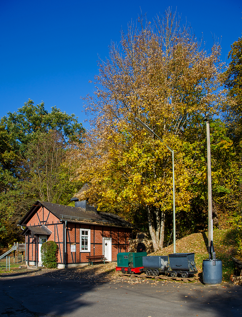 Die DIEMA Feldbahnlok vom Typ DL 6, Fabriknummer 1983, Baujahr 1956, Leistung 18 KW, Gewicht 1.115 kg, von 700 auf 600 mm um gespurt, als Denkmallok am 28.10.2021 mit zwei Grubenwagen beim Wodanstolln in Neunkirchen-Salchendorf. Wobei eigentlich ganz stilecht bzw. geschichtlich richtig ist dieses Denkmal nicht, denn die Lok ist eine Feldbahnlok. Bei den Siegerländer Erzgruben kamen aber Gubenloks zum Einsatz. 

Die DL 6 der Diepholzer Maschinenfabrik Fritz Schöttler (Diema) ist eine Diesellokomotive für Feldbahnen. Mit einem Gewicht von etwa 1 t, einer Länge von ca. 1,7 m und einem Achsstand von 0,5 m gehört sie zu den kleinsten Lokomotiven überhaupt. Die DL 6 entstand 1955 als kleinere und leistungsschwächere Version der DL 8. Insgesamt wurden 220 Exemplare gebaut, womit die DL 6 zu den erfolgreichsten Diema-Konstruktionen gehört. Eingesetzt wurden die Lokomotiven vor allem von kleinen Torfabbaubetrieben. Die letzte Lokomotive wurde im September 1970 ausgeliefert.

Die Lokomotiven sind auf einem geschweißten Außenrahmen aufgebaut. Die Breite des Rahmens hing von der Spurweite ab, insbesondere gab es eine Version für die in den Niederlanden verbreitete 700-mm-Spur, zu diese die Lok hier gehört. In der DL 6 kommen luftgekühlte Einzylinder-Dieselmotoren zum Einsatz. Die Leistungsübertragung erfolgt über einen Keilriemen vom Motor auf ein mechanisches Zweiganggetriebe und von dort aus über Rollenketten auf die beiden Achsen. Diese waren zunächst über Evolutfedern abgestützt, später wurden Schraubenfedern eingebaut.

Der Fahrersitz ist, wie bei Lokomotiven dieser Kategorie üblich, quer zur Fahrtrichtung eingebaut, so dass der Fahrer seine Position bei Fahrtrichtungswechseln nicht ändern muss. Motor und Getriebe nebst Schalthebeln befinden sich dabei rechts vom Fahrer, der Bremshebel links. Wobei bei dieser Lok der Fahrersitz fehlt.
