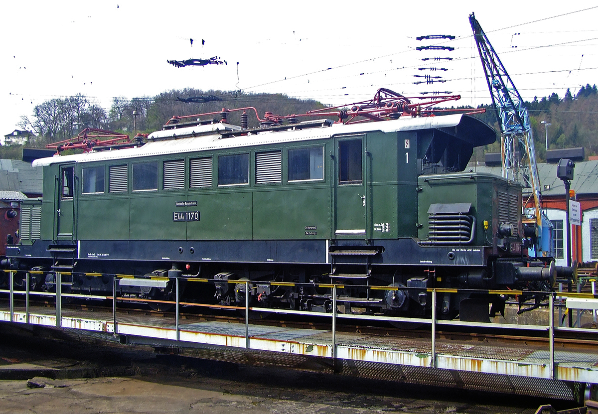 Die E 44 1170, ex DB 145 170-7, ex E 44 170W, wird am 12.04.2010 auf der Drehscheibe im Südwestfälische Eisenbahnmuseum in Siegen präsentiert. Leider eine meiner wenigen brauchbaren Aufnahmen von ihr.

Die Lok wurde 1944 von Krauss-Maffei in München unter der Fabriknummer 25575, der elektrische Teil ist von SSW (Siemens-Schuckertwerke), und wurde an die Deutschen Reichsbahn als E 44 107W geliefert. 

Die von der Deutschen Reichsbahn beschafften Lokomotiven der Baureihe E 44 wurden als Universalloks für den Personen- und Güterverkehr in Süd- und Mitteldeutschland eingesetzt. Die Elektrolokomotiven der Baureihe E44 waren die ersten E-Loks in Deutschland, die in größerer Stückzahl (187 Stück) gebaut wurden. Diese von den Siemens-Schuckertwerken als Universalloks konzipierten Lokomotiven prägten von 1933 bis in die 80er Jahre den Eisenbahnverkehr hauptsächlich in Süd- aber auch in Mitteldeutschland aufgrund ihrer Robustheit und Zuverlässigkeit. 1984 rollte letzte E44 der DB aufs Abstellgleis.
Einige Exemplare der E44 wurden für den Betrieb auf der steigungsreichen Höllentalbahn mit einer zusätzlichen elektrischen Widerstandsbremse ausgerüstet. Von den hiervon bestellten 40 Lokomotiven wurden zwischen 1943 und 1951 32 Stück gebaut.

Diese Loks wurden mit einem „W“ nach bzw. später mit einer „1“ vor der Loknummer gekennzeichnet, wie diese Lok hier (E44 170W, E44 1170) und ab 1968 als DB-Baureihe 145 bezeichnet. Die E44 1170 stand von 1944 bis 1983 im Dienst der Deutschen Bundesbahn, wobei sie die längste Zeit in Freiburg beheimatet war. Nach ihrer Ausmusterung war sie lange Zeit betriebsfähige Museumslok des Bw Freiburg und wurde regelmäßig vor Sonderzügen im Höllental und auf der Dreiseenbahn eingesetzt. 1996 wurde sie endgültig abgestellt und 2002 nach Siegen zu den Eisenbahnfreunden Betzdorf abgegeben. Seit 2010 ist sie nun im Fahrzeugbestand der IG 3seenbahn.

Die E 44 stellen einen Meilenstein der E-Lokentwicklung dar, denn hier wurde erstmals bei einer größeren Streckenlokomotive auf Vorlaufachsen und Stangenantrieb verzichtet. Insgesamt wurden 187 Maschinen gebaut, von denen jedoch etliche durch Kriegshandlungen einen Totalschaden erlitten und deshalb ausgemustert werden mussten. Die Mehrzahl der Lokomotiven kam zur Deutschen Bundesbahn. Diese baute sogar sieben Loks nach. Die DB rüstete mehrere Maschinen für den Wendezugbetrieb aus, kenntlich gemacht durch ein G hinter der Loknummer. Die E 44 mit elektrischer Bremse wurden durch ein W hinter der Loknummer kenntlich gemacht. 

TECHNISCHE DATEN:
Spurweite: 1.435 mm (Normalspur)
Achsformel:  Bo’Bo’
Länge über Puffer:  15.290 mm
Drehzapfenabstand: 6.300 mm
Drehgestellachsstand: 3.500 mm
Treibraddurchmesser : 1.250 mm
Eigengewicht: 77,2 t
Radsatzfahrmasse: 19,5 t
Höchstgeschwindigkeit:  90 km/h
Stundenleistung:  2.200 kW
Dauerleistung: 1.860 kW
Anfahrzugkraft: 196 kN
Stromsystem:  15 kV 16⅔ Hz
Anzahl der Fahrmotoren:  4
Antrieb: Tatzlager-Antrieb
