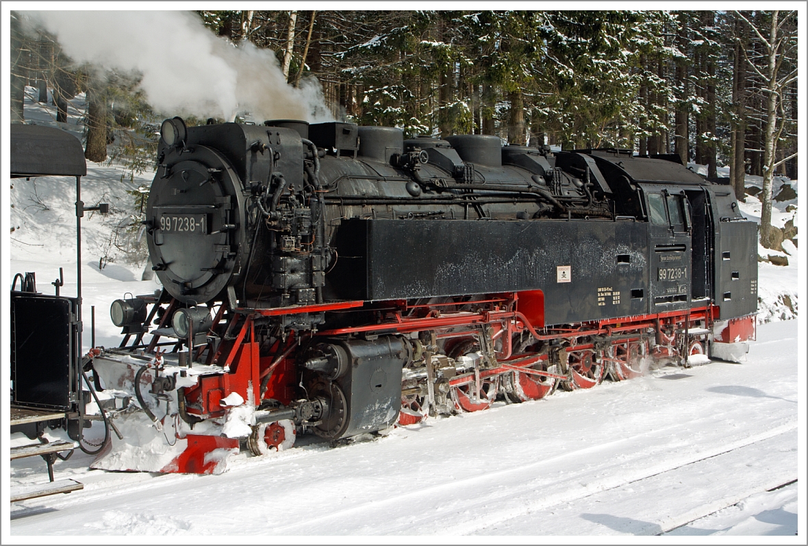 Die Neubaulokomotive 99 7238-1 der HSB (Harzer Schmalspurbahnen GmbH) hat am 23.03.2013 ihren Sonderzug vom Brocken zum Bahnhof Schierke hinab gebracht. 
Die Spuren von dem viele Schnee Mitte M�rz von auf dem Brocken sind (1,5 m) deutlich zu sehen.

Die Neubaumaschinen 99 231 bis 99 247 wurden in den 50er Jahren f�r die Schmalspurbahnen Eisfeld - Sch�nbrunn, Gera-Pforten - Wuitz - Mumsdorf und die Harzquer- und Brockenbahn durch den VEB Lokomotivbau  Karl Marx  in Babelsberg gebaut. Dies war unbedingt n�tig, da der Lokomotivpark dieser Bahnen v�llig �beraltert war. Au�erdem ging ein Teil der Maschinen im Krieg verloren. 

Die Konstruktion der Neubaumaschinen lehnt sich sehr stark an die der Einheitslokomotiven 99 221 bis 99 223 an. Von diesen ist aber nur die 99 222 erhalten geblieben. In vielen Konstruktionsmerkmalen weicht die Neubaulok jedoch von ihren Vorbildern ab. So wurde zum Beispiel der Rahmen als Blechrahmen ausgef�hrt. Die technologischen M�glichkeiten der Nachkriegszeit lie�en die Ausf�hrung als Barrenrahmen nicht zu. Der Kessel ist vollst�ndig geschwei�t, wobei der Langkessel aus einem einzigem Kesselschuss besteht. 
Nach der Einstellung des Betriebes auf der Eisfeld   Sch�nbrunner Strecke gelangten auch die 99 231, 99 235, 99 236 und 99 237 in den Harz. In einigen Details mussten diese Maschinen ver�ndert werden. Der Grund hierf�r besteht in den engen B�gen der Harzstrecken. Die Einheitslokomotiven  99 222 kam bereits 1966 in den Harz.

Anfang der 70er Jahre erfolgte eine Umnummerierung der Lokomotiven. Aus der 99 231 wurde die 99 7231 usw.. Dies sollte sich zwischenzeitlich noch einmal �ndern, als Ende der 70er Jahre alle Neubaumaschinen auf �lhauptfeuerung umgestellt wurden. Nun wurde aus der 99 7231 die 99 0231 usw.. Dies war f�r diese Lokomotiven eine nicht besonders positive Ma�nahme. Bei dem Umbau glaubte man, Brennstoff-Einsparungen vornehmen zu k�nnen. Die Einsparung eines zweiten Brenners erkaufte man sich aber mit Kesselsch�den. 

Im Rahmen der �labl�sung in der damaligen DDR baute man die Maschinen wieder auf Rostfeuerung um. Ein Segen f�r die Loks aber auch f�r die Umwelt, denn nicht verbranntes �l sickerte nicht mehr in die Gleise und in den Boden. 
Heute ist die Arbeit des Heizers zwar etwas beschwerlicher aber besonders in den Sommermonaten ist die Hitze lange nicht so gro� wie damals mit dem geheizten �ltender und dem harten �lfeuer. 

Nun haben die Maschinen wieder ihre 99 72er Nummer. Obwohl die Deutschen Reichsbahn dazu �berging Schmalspurdampflokomotiven mit 099 zu bezeichnen und mit einer neuen Betriebsnummer zu versehen, wurde auf den Harzer Schmalspurbahnen die alte Reichsbahnbezeichnung beibehalten.

Technische Daten dieser Loks:
Hersteller: VEB Lokomotivbau  Karl Marx  in Babelsberg 
Baujahre: 1954 - 1956
Achsfolge: 1'E1' 
Gattung: K57.10 
Spurweite: 1.000 mm (Meterspur) 
L�nge �ber Puffer: 12.500 mm
Kessel�berdruck : 14 bar
Leistung: 515 kW (700 PS)
H�chstgeschwindigkeit: 40 km/h (Vor- und R�ckw�rts)
Dienstgewicht: 64,5 t (bei vollen Vorr�ten)
Kohlevorrat: 4,0 t
Wasservorrat: 8 m�
Achslast: 9,5 t
