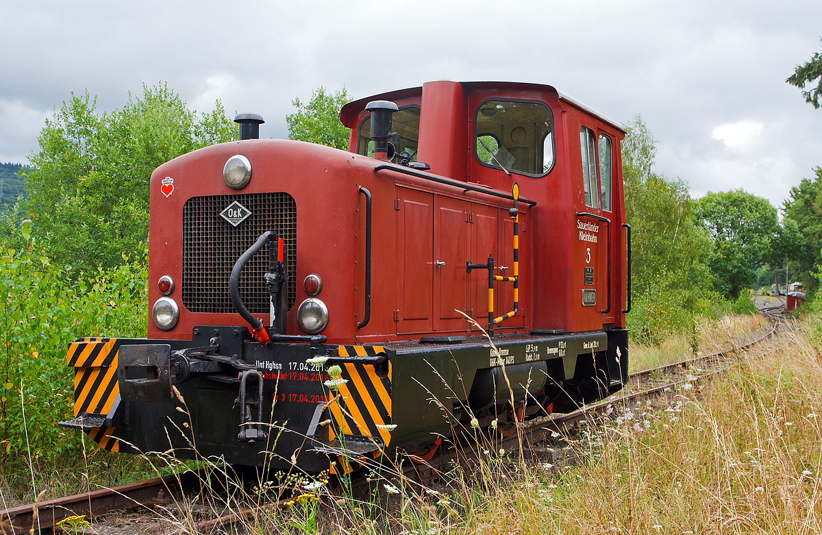 
Die O+K Lok V3  NAHMER  der Sauerländer Kleinbahn (MME Märkische Museums-Eisenbahn), ex V3 der Hohenlimburger Kleinbahn AG (HKB) ist am 18.08.2013 am Gleisende beim Bahnhof Hüinghausen zur Gleissicherung abgestellt.

Die Firma Orenstein und Koppel (O&K), Werk Dortmund-Dorstfeld lieferte 1960 insgesamt 5 baugleiche, zweiachsige dieselhydraulische Lokomotiven (1.000 mm Spurweite) des Typs MV8 mit Endführerstand, an die Hohenlimburger Kleinbahn AG. Die Lokomotiven waren mit einer pneumatischen Mehrfachsteuerung ausgerüstet, da die Züge ins Nahmertal größtenteils mit 2 Maschinen gefahren werden mussten. Die Kraftübertragung auf die Räder erfolgt über Blindwelle und Kuppelstangen. Bis zur Betriebseinstellung der HKB am 23.12.1983 waren die Maschinen im Einsatz. Am 28.07.1984 gelangte die Lok Nr.3 in den Besitz der Märkischen Museumseisenbahn (MME). Dort erhielt sie in Erinnerung an ihre alte Heimat den Namen  NAHMER , nach dem gleichnamigen Bach in dessen Tal die Bahn verlief. 

Technische Daten: 
Fabriknummer: 25988 
Spurweite: 1.000 mm 
Länge über Puffer: 5.900 mm 
Achsabstand: 1.500 mm 
Dienstgewicht: 20.700 kg 
Motor: Orenstein & Koppel wassergekühlter 6 Zylinder 4-takt Dieselmotor 116 V6 D 
Hubraum: 10,85l 
Motorleistung: 140 PS (103 kW) bei 1.500 U/min 
Getriebe: Voith L22 nV Zweigang-Turbogetriebe (Wandler+Kupplung) 
Höchstgeschwindigkeit: 17,5 km/h