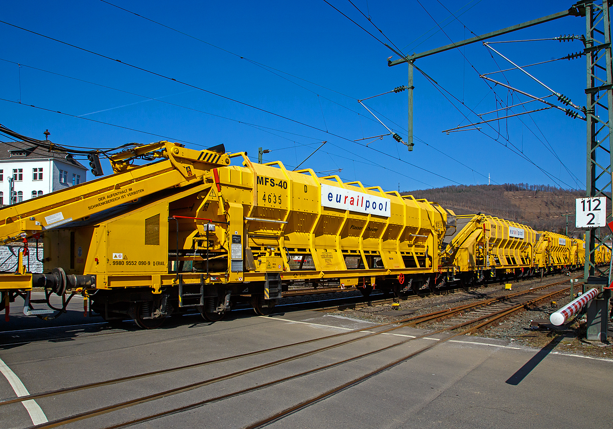 Die Plasser & Theurer Materialförder- und Siloeinheit MFS 40 D (mit schwenkbarem Entladeband), Nr. 4635 der eurailpool GmbH, Schweres Nebenfahrzeug Nr. 99 80 9552 090-9 D-ERAIL, am 24.03.2021 bei der Zugdurchfahrt in Niederschelden (Sieg), hier passiert er gerade den Bü 343 (Km 112,183 der Siegstrecke KBS 460).

Die Einheit wurde 1992 von Plasser & Theurer unter der Fabriknummer 4635 gebaut.

Die Materialförder- und Siloeinheiten dienen sowohl der Materialversorgung als auch zum Abtransport der Aushubmassen ohne Benutzung des Nachbargleises. Die Beladung erfolgt mittels Radlader oder Bagger über eine Beladestation oder direkt in die MFS. Der Abraum wird über schwenkbare Förderbänder auf Zwischenlagerplätze oder K-Wagen entladen.

TECHNISCHE DATEN:
Spurweite: 1.435 m
Anzahl der Achsen: 6 in 2 Drehgestellen
Länge über Puffer: 18.300 mm
Drehzapfenabstand: 11.000 mm
Achsabstand im Drehgestell: 3.400 mm (2 x 1.700 mm)
Fassungsvermögen: 40 m³
Eigengewicht: 40.000 kg
Nutzlast: 53,3 t ab Streckenklasse C
Motorleistung: 50 kW (für Antrieb der Förderbänder)
Höchstgeschwindigkeit: 100 km/h (geschleppt)
Bremse: KE-GP
Feststellbremse: Ja
Kleinster bef. Halbmesser:  R 120 m
