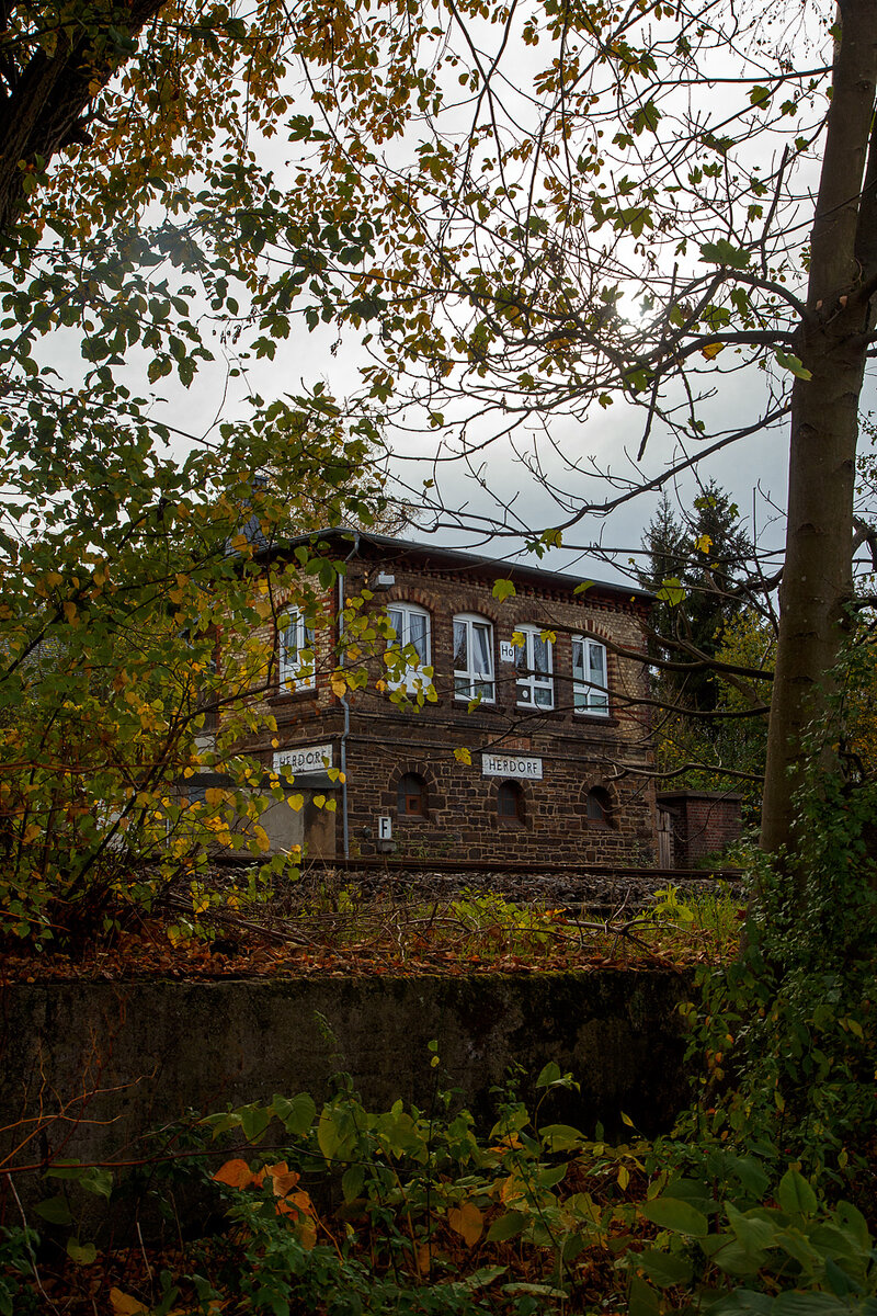 Ein etwas anderer Blick auf das1901 gebaute mechanische Weichenwärter Stellwerk Herdorf Ost (Ho), an der Bahnstrecke Betzdorf - Haiger (KBS 462 „Hellertalbahn“), hier am 03.11.2022.

Ja, in Herdorf gibt es immer noch den Luxus von zwei in Betrieb befindlichen Stellwerken das Stellwerk Herdorf Fahrdienstleiter (Hf) und das hier zusende Weichenwärter Stellwerk Herdorf Ost (Ho). Sie liegen in Sichtweite ca. 600 m entfernt, Hf beim Bahnhof und hier Ho in der Nähe zum Abzweig zur Anschlussstelle KSW (ex Freien Grunder Eisenbahn). Bis in die 1960-Jahre waren die Aufgaben des Weichenwärters noch sehr umfangreicher. Die Strecke war noch eine zweigleisige Hauptstrecke. Ursprüngliche Planungen sahen sogar vor, sie im Rahmen der Elektrifizierung der Siegstrecke ebenfalls zu elektrifizieren. Diese Erwägungen wurden aber leider nicht weiter verfolgt. Zudem gab es noch Anschlussstellen zur Herdorfer Friedrichs Hütte und zu den Eiserfelder Steinwerken AG.

Da die Stellwerkstechnik in Herdorf noch rein mechanisch ist, werden beide noch benötigt, bzw. ein Umbau auf ein Stellwerk ist wohl zu aufwendig.