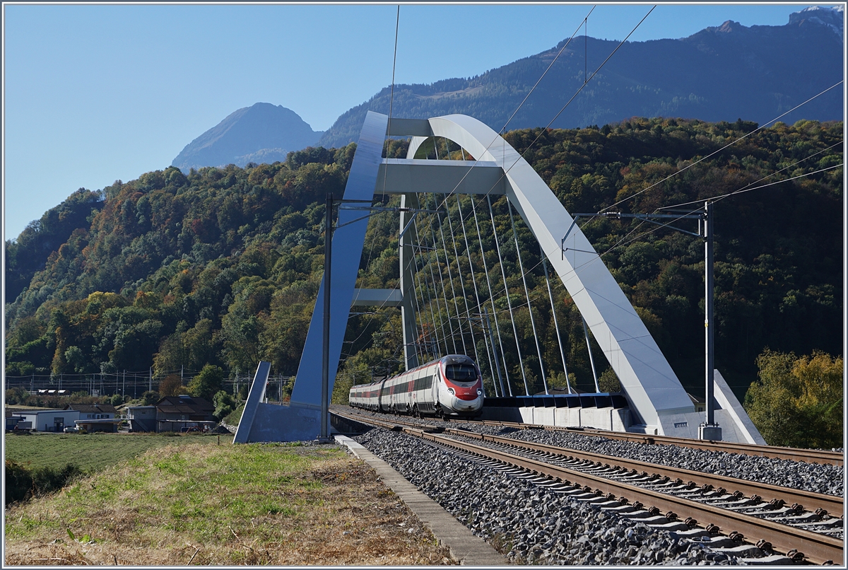 Fast 23 Meter über die Gleise wölbt sich die beiden Bögen der SBB Brücke  Massogex , die zwischen Bex und St-Maurice über die Rhone führt. Die Brücke weist eine Spannweite von  125.8 Meter auf und gilt als längste Stählerne Eisenbahnbrücke der Schweiz. Sie ersetzt seit 2016 die beiden aus den Jahren 1903 und 1924 stammenden eingeleisigen Stahlbrücken. (Tech. Ang. Quelle: TEC21 Nr 41).
Das Bild zeigt einen SBB ETR 610 der Als EC 32 von Milano nach Genève unterwegs ist.
11. Okt. 2017