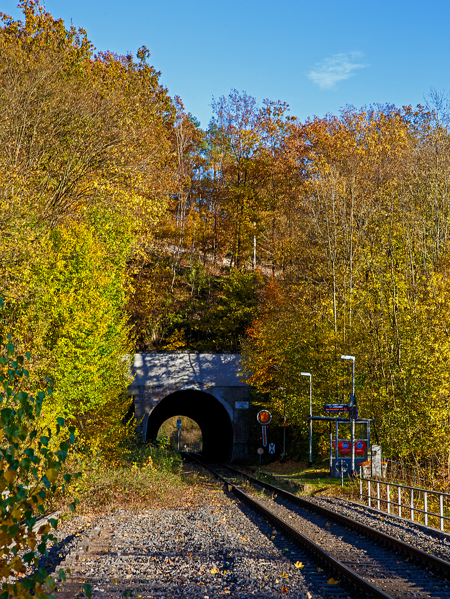 Herbstzeit im Hellertal.....
Der Bedarfs-Haltepunkt Herdorf-Königsstollen dahinter der Herdorfer Tunnel (137 m lang) bei km 88,6 der Hellertalbahn - KBS 462 (Bahnstrecke Köln-Deutz – Betzdorf – Herdorf – Haiger – Gießen). Vorm Tunnel das (Form) Vorsignal für das Einfahrtsignal vom Bahnhof. Es zeigt Vr 0 „Halt erwarten“ (Die runde Scheibe steht senkrecht, der Flügel zeigt er senkrecht nach unten). 

Die Hellertalbahn wurde als Teil der Deutz-Gießener Eisenbahn gebaut, die in den Jahren 1859 bis 1862 als Hauptbahn von Köln-Deutz nach Gießen in mehreren Etappen durch die Cöln-Mindener Eisenbahn errichtet wurde. Aufgrund der Verkehrsentwicklung und der militärischen Bedeutung 1870/71 wurde die Strecke 1871 zweigleisig ausgebaut. 

Damals war diese Strecke noch die Hauptstrecke. Der Niedergang der Hellertalstrecke begann im Jahre 1915, als die durch den Rudersdorfer Tunnel verlaufende Alternative eröffnet wurde, erst ab da gab es eine direkte Verbindung zwischen Siegen und Haiger. Sowohl der hochwertige Reiseverkehr als auch der Großteil des Güterverkehrs nutzten nunmehr die direkte und günstiger trassierte Dillstrecke in Richtung Gießen und weiter ins Rhein-Main-Gebiet. 

Im Hellertal wurde aber noch Eisenerz abgebaut und auf die Bahn verladen. Auch gab es in Herdorf eine Stahlhütte. So war der Niedergang des Siegerländer Erzbergbaus Anfang der 1960er Jahre dann der große Niedergang der Stecke. Zudem wurden die Ruhr-Sieg- , die Sieg- und die Dillstrecke elektrifiziert. So wurde die Strecke Mitte der 1960er Jahre als Nebenstrecke zurückgestuft, folgte im Jahre 1965 die Demontage des zweiten Gleises im Bereich Herdorf–Haiger. Im Jahr 1987 wurde das zweite Gleis auf dem Abschnitt Betzdorf–Herdorf stillgelegt. Hier im Bild kann man (links) noch das zweite Gleis erahnen.

Heute erinnern nur noch die durchgehende Kilometrierung von Köln-Deutz und die gemeinsame Streckennummer an die alte Streckenführung.