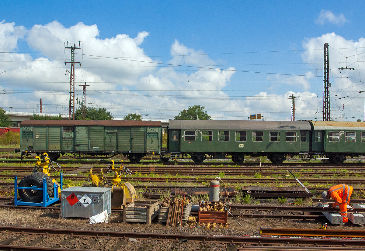 In Hanau am 27.08.2014 aus einem Zug heraus:
Links der zweiachsige ehemaliger Bahnpostwagen der Deutschen Post (DP) der DDR, 75 80 9229 054-6 D-MH, ex 50 50 09-10 076-7, ex DEW 1264 Post aa-c, ex DP/DR 83 076, ex Post 2ss-t (Deutschen Bundespost), der Museumseisenbahn Hanau e.V. (fr�her Dampfbahnfreunde Kahlgrund e.V.).

1983/84 importierte die DP aus Rum�nien 140 zweiachsige Bahnpostwagen, die f�r den Rollbeh�lterverkehr in schnellfahrenden Reisez�gen (D-, E-, Post- und Gex-Z�ge) bestimmt und dementsprechend mit Dampfheizleitung, Zugsammelschiene und mit Bremsen der Bauart KE-GP A ausger�stet waren. Die zul�ssige Hg betrug 120 km/h. Nach �bernahme und Umzeichnung in Post 2ss-t/12 im Jahre 1990 trennte sich die Deutsche Bundespost bis 1994 von diesen Wagen. Im Wandel des Gesamtdeutschen Bahnverkehrs war kein Platz mehr f�r Bahnpostwagen. Innerdeutsch wird heute die Post mit LKW´s transportiert.

TECHNISCHE DATEN Bahnpostwagen:
Hersteller: MEVA in Turnu Severin (Rum�nien), heute Astra Rail Industries
Baujahr: 1984
Spurweite: 1.435 mm
Anzahl der Achsen: 2
L�nge �ber Puffer: 14.270 mm
Achsabstand: 8.000 mm
H�chstgeschwindigkeit: 100
Eigengewicht: 13.200 kg
Ladegewicht: 22 t
Bremse: KE-GP


Und rechts der dreiachsige B3yg ex DB Umbauwagen, ex DB 88 701 Ffm, der Museumseisenbahn Hanau e.V., kurzgekuppelt mit dem ex DB 88 166 Ffm.

Der Umbauwagen wurde 1957 vom AW Hannover aus dem Untergestell des Abteilwagen C3yg-*/54 (ex DB 049 655, ex DB Opp 70037, ex DRB Opp 847), der 1903 von der Waggonfabrik Breslau gebaut wurde, umgebaut.

Bei der DB war er von 1957-1966 als 88 701Ffm der Gattung B3yg-54 und von 1967 bis 1977 der Gattung B3yg761 unterwegs, bis 1990 war er Bahnhofswagen Heilbronn, sp�ter ging er zu den Dampfbahnfreunde Kahlgrund e.V., seit 2010 hat er die NVR-Nr. 75 80 2329 040-9 D-MH. Der Wagen wurde im Fr�hjahr 2020 optisch und technisch aufgearbeitet und komplett neu lackiert. Er bildet mit dem B3yg-54 Wagen 88 166 Ffm eine Einheit als kurzgekuppeltes 3yg-P�rchen.

TECHNISCHE DATEN Umbauwagen:
Umbauer: AW Hannover
Umbaujahr: 1957
Spurweite: 1.435 mm
Anzahl der Achsen: 3
L�nge �ber Puffer: 13.300 mm
Achsabstand: 7.500 mm (2x 3.750 mm) 
H�chstgeschwindigkeit: 100
Eigengewicht: 18.300 kg
Sitzpl�tze: 62

