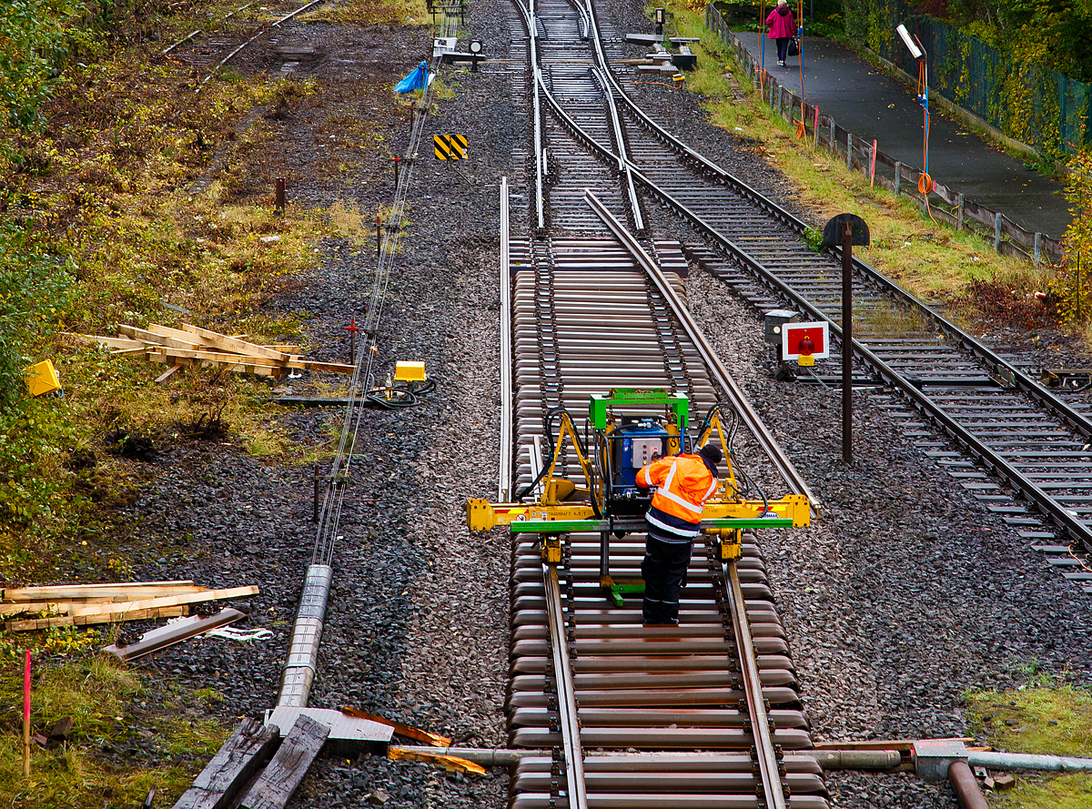 
Mittels einer hydraulischen Schienenumsetzmaschine vom Typ Giesmar MPRM 1032 werden am 15.10.2020 in Herdorf die letzten Meter Schienen auf die Schwellen gesetzt.

Die Schienenumsetzmaschine ist eine selbstangetriebene hydraulisch angetriebene Einheit zum Verlegen und Entfernen von langgeschweißten Schienen mit einem Bediener. Das Gerät stützt sich auf den Schwellen ab, die Schienen werden aufgenommen und können dann bis zu 500 mm angehoben werden. Nun erfolgt die seitliche Verschiebung und die Schienen werden auf die richtige Position auf der Schwelle abgelegt. Das Gerät ist geeignet für Scheinen mit einem Metergewicht von 37 bis 70 kg, die max. Hubkraft beträgt 4.500 kg. Es ist zudem möglich einen hydraulischen Schienenzieher ATR 6 anzuschließen. Das Eigengewicht von dem Gerät beträgt ca. 1.065 kg. 

Der hydraulische Antrieb erfolgt mittels einer HATZ-Hydraulikpumpen-Einheit (Hatz-Außenzahnradpumpe und Dieselmotor). Die Pumpe wird angetrieben von einem HATZ luftgekühltem Einzylinder-4-Takt Dieselmotor mit Direkteinspritzung und horizontale Kurbelwelle vom Typ 1D42C. 
