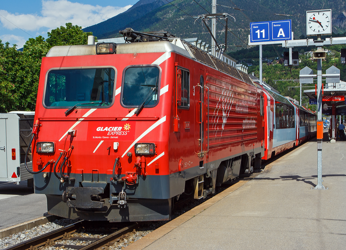 
Neue Version in 1200px....
Die MGB HGe 4/4 II - 3   Dom  (ex BVZ 3   Dom )  steht am 28.05.2012 mit Glacier Express im Bahnhof (-vorplatz) von Brig. 

Der Taufname  Dom  bezieht sich auf den in den Walliser Alpen liegenden Berg Dom (4.545 m ü. M.). Die MGB HGe 4/4 II - 3  Dom  wurde von SLM (Schweizerische Lokomotiv- und Maschinenfabrik) in Winterthur 1990 unter der Fabriknummer 5421 gebaut und an die Brig-Visp-Zermatt-Bahn (BVZ) geliefert. Der elektrische Teil ist von ABB.

Die HGe 4/4 II ist eine schmalspurige (1.000 mm) gemischte Zahnrad- und Adhäsions-Lokomotive. Eine erste Serie von fünf Lokomotiven wurde gemeinsam von der Furka-Oberalp-Bahn (FO) sowie von der SBB für die Brünigbahn, die heute zur Zentralbahn (zb) gehört, beschafft. Da sich dieser Lokomotivtyp bewährte, wurden weitere elf Lokomotiven bestellt, und schließlich gab auch noch die Brig-Visp-Zermatt-Bahn (BVZ) fünf Loks in Auftrag.

Die HGe 4/4 II bespannt vor allem schwere Personenzüge, zum Teil im Pendelzugbetrieb. Bei der Zentralbahn bespannte sie bis 2012 alle Schnellzüge von Meiringen nach Luzern, bei der Matterhorn Gotthard Bahn die Züge des Glacier-Express. Weiter führen die Loks Pendelzüge Brig–Visp–Zermatt und seit der Eröffnung des Tunnels nach Engelberg Pendelzüge Luzern–Engelberg. Außerdem werden aushilfsweise Autopendelzüge durch den Furkatunnel geführt. Schließlich gehören neben weiteren Personenzügen auch diverse Güterzüge Visp–Zermatt sowie bis 2013 Disentis–Sedrun (NEAT-Baustelle) zum Aufgabengebiet.

Konstruktion:
Der Lokomotivkasten ist ein Stahlblechkasten mit gesickten Seitenwänden. Die asymmetrische Frontscheibe aus beheizbarem Verbundglas verbessert die Sicht für den Lokomotivführer. Die drei Dachelemente sind aus Aluminium. Die Pufferkräfte werden über Verstrebungen auf den ganzen Kasten übertragen, weshalb auf seitliche Maschinenraumöffnungen verzichtet werden musste. Der gesamte Kasten hat ein Gesamtgewicht von nur 5,9 Tonnen. Er kann ohne bleibende Deformation eine zentrale Druckkraft von 1000 kN aufnehmen.

Die Drehgestelle sind als geschweißte Hohlträgerkonstruktion mit zwei Längsträgern und einem kräftigen mittleren Querträger sowie zwei Kopftraversen ausgeführt. Sie haben einen Achsstand von 2980 mm, und die Flexicoilfedern stützen den Kasten auf die seitlich an die Längsträger angeschweißten Federwannen. Die Zug- und Druckkräfte werden durch seitlich angeordnete Stangen mit Sphärolastiklagern übertragen. Wegen des kurzen Achsstands sind die Fahrmotoren oberhalb des Drehgestellrahmens angebracht.

Für den Antrieb wurde erstmals der Differentialantrieb eingebaut, der es ermöglicht, im Zahnstangenbetrieb auch einen Anteil der Zugkraft über den Adhäsionsantrieb aufzubringen. Dies setzt wiederum eine Schlupfbegrenzung im Differentialgetriebe voraus, um ein Schleudern oder Gleiten der Räder zu verhindern. Da die zweilamellige Abtzahnstange (System Abt) der FO nicht die gesamte Zugkraft aufnehmen kann, ist die Mithilfe des Adhäsionsantriebs notwendig; dieser übernimmt einen Drittel der Zugkraft. Hätte sich der Antrieb nicht bewährt, wäre es zumindest am Brünig mit der Riggenbachzahnstange möglich gewesen, auf einen abkuppelbaren Adhäsionsantrieb zu wechseln. Dies war aber nicht notwendig, da das Differentialgetriebe zur vollen Zufriedenheit funktionierte.

Bremssysteme:
Dank der elektrischen Rekuperationsbremse ist eine gleichmäßige Beharrungsbremse bei der Talfahrt möglich.
Daneben ist eine normale automatische Druckluftbremse eingebaut, welche auch als Bremssystem I bezeichnet und im Regelbetrieb zum Halten des Zuges verwendet wird. Sie ist als Klotzbremse ausgeführt.
Weiterhin ist noch das Bremssystem II installiert, welches für Zahnradbahnen vorgeschrieben ist und es ermöglichen soll, den Zug nur mit Hilfe der Lokomotive im Zahnstangenabschnitt zum Halten zu bringen, wenn das erste Bremssystem ausfallen sollte. Dieses ist als federspeichergestütztes Bandbremssystem ausgelegt, welches direkt auf das Zahnrad wirkt. Bei Einsatz dieser Bremse treten enorme Kräfte auf, welche nur unter Kontrolle sind, wenn die Anhängelast bei der Talfahrt nicht zu groß ist.
Schließlich ist eine direkt wirkende Rangierbremse vorhanden, die sich der Bremsklötze des Bremssystems I bedient.
Die Lokomotive hat keine Handbremse, sondern wird mit Federspeicherbremsen gesichert.

Technische Daten, der HGe 4/4 II MGB (ex FO bzw. BVZ), die der zb weichen ab:
Spurweite: 1.000 mm
Achsformel: Bo'Bo'
Dienstgewicht: 64 t 
Achslast: 16 t
Länge über Puffer: 14'.776 mm 
Höchstgeschwindigkeit Adhäsion: 100 km/h
Höchstgeschwindigkeit Zahnrad: 40 km/h
Stromsystem: 11 kV 16.7 Hz
Anzahl der Motoren: 4
Adhäsions-Antrieb: Gelenkwelle
Antrieb Zahnrad: Differentialantrieb
Zahnradsystem:  Abt (zweilamellig)
Stundenleistung: 1.932 kW
Dauerleistung: 1.875 kW
Anfahrzugkraft: 230 kN (Adhäsion) / 280 kN (Zahnrad)
Anzahl Bremssysteme: 4
Bremsen: Rekuperation, Klotz, Federspeicher, Bandbremse
Anhängelast: 130 t (125 ‰)