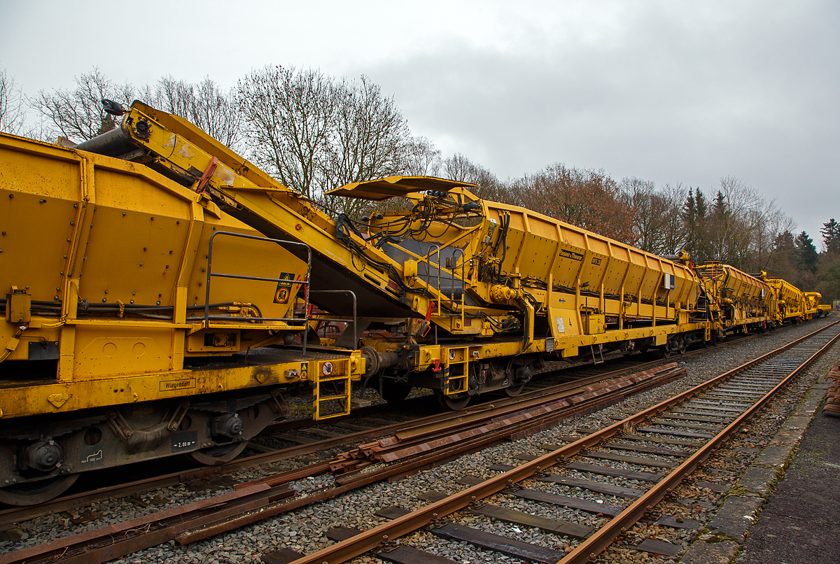 Plasser & Theurer Material-, Förder- und Siloeinheiten MFS 38 (teilweise auch BSW 2000 - Bunker-Schüttgut-Wagen genannt) der HERING Bahnbau, Burbach, Nr. 4, Schweres Nebenfahrzeug Nr. D-HGUI 99 80 9552 122-0, ex 97 19 22 551 17-3, ist am 20.12.2020 auf dem Betriebshof der Westerwaldbahn (WEBA) auf der Bindweide bei Steinebach/Sieg abgestellt.

Diese MFS 38 wurde 1993 von Plasser & Theurer unter der Fabriknummer 2158 gebaut, wobei als Fahrgestell ein vierachsiger ehemaliger Drehgestell-Flachwagen der Gattung Rs 680 (ex SSlmas 53), der 1962 von M.A.N. im Werk Nürnberg unter der Fabriknummer 146718 gebaut wurde, Verwendung fand. Diese Wagen wurden Plasser & Theurer vom Kunden beigestellt. Bei einem Drehgestell konnte ich als Hersteller LHB (Linke-Hofmann-Busch, Salzgitter) ausmachen (Baujahr 1965, Fabriknummer 3109).

TECHNISCHE DATEN:
Maschinenart: Material-Förder-Siloeinheit MSF 38
Hersteller: Plasser & Theurer
Spurweite: 1.435 mm (Normalspur)
Anzahl der Achsen: 4 (in 2 Drehgestellen)
Länge über Puffer:19.900 mm
Gesamtlänge mit Übergabeband: 23.550 mm
Drehzapfenabstand: 13.000 mm
Achsabstand im Drehgestell: 2.000 mm
Laufraddurchmesser: 1.000 mm (neu)
Drehgestell-Bauart: Minden Dorstfeld-Drehgestell 931 / 932
Breite: 2.890 mm
Höhe: 4.280 mm
Eigengewicht: 38 t
Max. Zuladung (Nutzlast): 42 t
Ladevolumen: 38 m³
Höchstgeschwindigkeit: 100 km/h (geschleppt)
Kleister befahrbarer Gleisbogen: R=120 m (angeschrieben)
Bremse: KE – GP
Motor: luftgekühlter Deutz Dieselmotor vom Typ F6L 912 F
Leistung: 82 kW
Dieseltankvolumen: 750 l
Übergabeband: +/- 45 Grad schwenkbar.
Entladezeit: 3,5 Minuten
Entladeabstand von Gleismitte: max. 4,5 m
Die Förderbänder sind in folgenden Geschwindigkeiten regelbar:
