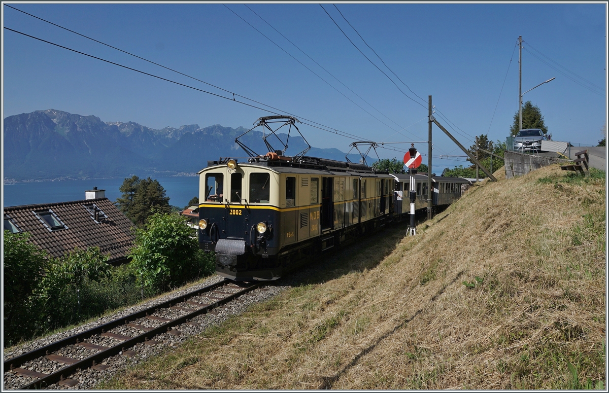 Zugunsten der Aussicht wählte ich hier die Schattenseite des Zuges, welcher der MOB DZe 6/6 2002 kurz nach Blonay in Richtung Chamby zieht. Im Hintergrund rechts des Zuges ist das Einfahrsignal von Blonay zu erkennen, eine Hippsche Wendescheibe, genannt nach seinem Erbauer, dem Elektriker und Uhrenmacher Matthäus Hipp, geboren in Blaubeuren (1813), der dann beruflich in der Schweiz tätig war. 
Der Blick gleitet des weitern weit über den Genfersee zu den Savoyer Alpen. 

4. Juni 2022