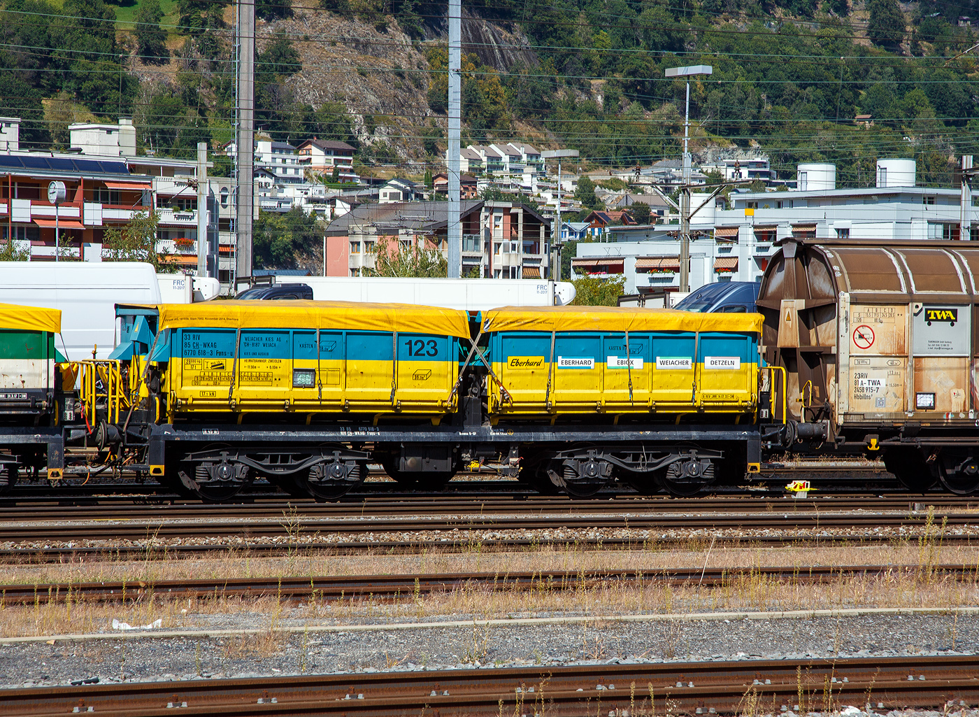 4-achsigiger offener Drehgestell-Schüttgutkippwagen mit zwei Mulden (Zweiseiten-Kastenkipper), 33 85 6770 618-3 CH-WKAG, der Gattung Fans-u, der Wagen 123, der Weiacher Kies AG (zur Eberhard Holding AG) abgestellt am 07 September 2021 beim Bahnhof Brig.

Der zweimuldige Drehgestell-Schüttgutkippwagen (Zweiseiten-Kastenkipper) ist für den Transport von feuchtigkeitsunempfindlichen Schüttgütern wie z.B. Splitt, Kies, Schotter, erdfeuchtem Sand, Bodenaushub oder Bauschutt vorgesehen. Der Wagen besitzt einen elektrohydraulischen Kippantrieb.

TECHNISCHE DATEN (laut Anschriften):
Spurweite: 1.435 mm (Normalspur)
Achsanzahl: 4 in zwei Drehgestellen
Länge über Puffer: 11.560 mm
Drehzapfenabstand: 6.100 mm
Achsabstand im Drehgestell: 1.800 mm
Laufraddurchmesser: 920 mm (neu)
Laderaum: 2 x 18,0 m³ = 36,0 m³
Entlade Kippwinkel: 55°
Höchstgeschwindigkeit: 100 km/h (beladen) / 120 km/h (leer)
Maximales Ladegewicht: 61,1 t (ab Streckenklasse D4)
Eigengewicht: 28.880 kg
Kleinster befahrbarer Gleisradius: R 45 m
Bremse: O-GP (K)
Bremssohle: Cosid 810
Intern. Verwendungsfähigkeit: RIV
Heimatbahnhof: Zweidlen (im Zürcher Unterland)

Bedeutung der Gattung Fans-u:
F = Offener Güterwagen in Sonderbauart
a = Mit 4 Achsen
n = Tragfähigkeit über 60 t
s = Höchstgeschwindigkeit 100 km/h
u = Elektro-hydraulische Kippvorrichtung

Die Züge der Weiacher Kies AG:
Kieszüge:
Die 5 Kieskompositionen der Weiacher Kies AG mit je 20 Waggons sind in der Lage, 1.100 Tonnen Kiesmaterial pro Blockzug zu befördern. Entsprechende Ladeeinrichtungen ermöglichen ein rasches Beladen (1 Stunde) der Züge im Werk. Je nach Entladeeinrichtung sind 2-4 Stunden notwendig, um einen ganzen Zug zu entladen. Eine Fahrt mit einer Zugkomposition entlastet das Straßennetz von rund 50 Lastwagenfahrten. 

Aushubzüge:
Ein beachtlicher Anteil an Aushubmaterialien für die Wiederauffüllung der Grube im Kieswerk Weiach erfolgt per Bahn. Bereits 1985 wurden leistungsfähige Aushubentladestellen und hauseigene Blockzüge angeschafft, um Aushub- und Ausbruchmaterial umweltfreundlich nach Weiach transportieren zu können. Jährlich können in Weiach bis zu 300.000 Tonnen Aushubmaterial per Bahn in die Deponie geliefert werden, was durchschnittlich 1 bis 2 Zugkompositionen pro Tag entspricht. Ohne die umweltschonende Bahn wären die riesigen Mengen gar nicht zu bewältigen. Im Bodenannahmezentrum BAZO in Oberglatt und der Bodenwaschanlage ESAR in Rümlang werden Materialien mit allen Kontaminierungssstufen per Bahn angeliefert und verarbeiten. Beton- und Mischabbruch von Baustellen werden, wenn immer möglich, per Bahn in den Aufbereitungsanlagen EbiMIK in Oberglatt und EBIREC in Rümlang transportiert.

Für den Schienenverkehr besitzt die Weiacher Kies AG 45 eigene Kippwagen vom Typ Fans-U, 19 Tams-Wagen, 20 Containertragwagen, zwei Rangierlokomotiven vom Typ Schöma CHL 350 und eine Rangierlok des Typs Fanny D850. 

Seit dem 1. Juli 2021 muss im Kanton Zürich sauberer Aushub aus Baugruben mit einem Volumen von über 25.000 m³ zwingend mit der Bahn abtransportiert werden.


Dank den großzügig angelegten Bahnanschlüssen in den Weiacher Kies AG Werken mit mehreren Gleisen und eigenen Rangierloks, können diese Einzelwagen sowie Ganzzüge mit den verschiedensten Materialien schweizweit oder international, ökologisch in ihre Werke liefern oder abtransportieren. Die Weiacher Kies AG verfügt zudem mit rund 120 Spezialcontainern über eine zusätzliche und umweltschonende Transporttechnik für eine Kombination von Bahn-LKW-Schiff.

Durch den Bahntransport wird der Straßenverkehr entlastet und die Umwelt geschont.
