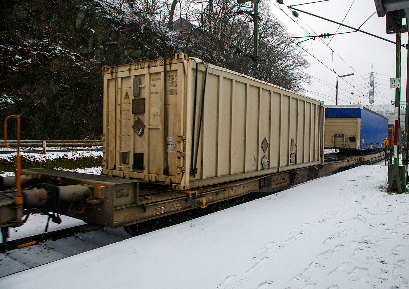 Achtachsiger niedrig gelegte Doppelwagen Jumbo II / Mega II (Trag-/Taschenwagen-Doppeleinheit) der Gattung Sdggmrrss, 33 85 493 3 329-5 CH-HUPAC, der Hupac Intermodal SA, am 19.01.2023 im Zugverband bei einer Zugdurchfahrt in Scheuerfeld (Sieg) in Richtung Köln.Hier beladen vorne mit einem Sattelzugauflieger und mit einem Container.

Diese Wageneinheiten bestehen aus einer niedrigen Tragwagenhälfte für Container und Wechselbehälter („CT“) und einer niedrigen Taschenwagenhälfte („SK“). Die beiden Wagenhälften sind mit einer, im Normalbetrieb nicht zu trennenden, (von den Waggons der RoLa, Saadkms 690, abgeleiteten) Kurzkupplung verbunden.