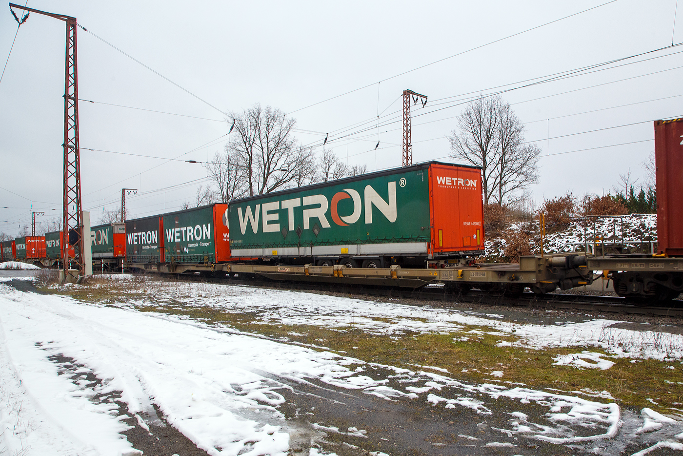 Achtachsiger niedrig gelegter Doppelwagen Mega II (Trag-/Taschenwagen-Doppeleinheit) der Serie IV, 83 85 4933 325-3 CH-HUPAC der Gattung Sdggmrrss, der HUPAC Intermodal SA, im Zugverband am 27.01.2023 bei der Zugdurchfahrt in Rudersdorf (Kr. Siegen), hier beladen mit einem Sattelauflieger und zwei Wechselbrücken.

Diese Wageneinheiten bestehen aus einer niedrigen Tragwagenhälfte für Container und Wechselbehälter („CT“) und einer niedrigen Taschenwagenhälfte („SK“). Die beiden Wagenhälften sind mit einer, im Normalbetrieb nicht zu trennenden, (von den Waggons der RoLa, Saadkms 690, abgeleiteten) Kurzkupplung verbunden. Durch die niedrig gelegte Ladefläche können C 70-400 kodifizierte Jumbo-Wechselbehälter bis Norditalien und High-Cube-Container bis Süditalien auf der Gotthardstrecke transportiert werden.

Diese Wagen der 4. Serie wurden ab 2003 von der Ferriere Cattaneo in Giubiasco (CH) gebaut.

TECHNISCHE DATEN:
Spurweite: 1.435 mm
Länge über Puffer: 36.880 mm
Drehzapfenabstand: 2 x 13.350 mm
Achsabstand im Drehgestellen: 1.800 mm
Eigengewicht: ca. 35.600 kg
Max. Zuladung bei Lastgrenze S: 92,4 t (ab Streckenklasse A)
Max. Zuladung bei Lastgrenze SS: 60,4 t (ab Streckenklasse A)
Max. Geschwindigkeit: 100 km/h / bei Lastgrenze SS und leer 120 km/h
Kleinster befahrbarer Gleisbogen: R 75 m
Intern. Verwendungsfähigkeit: Privatwagen