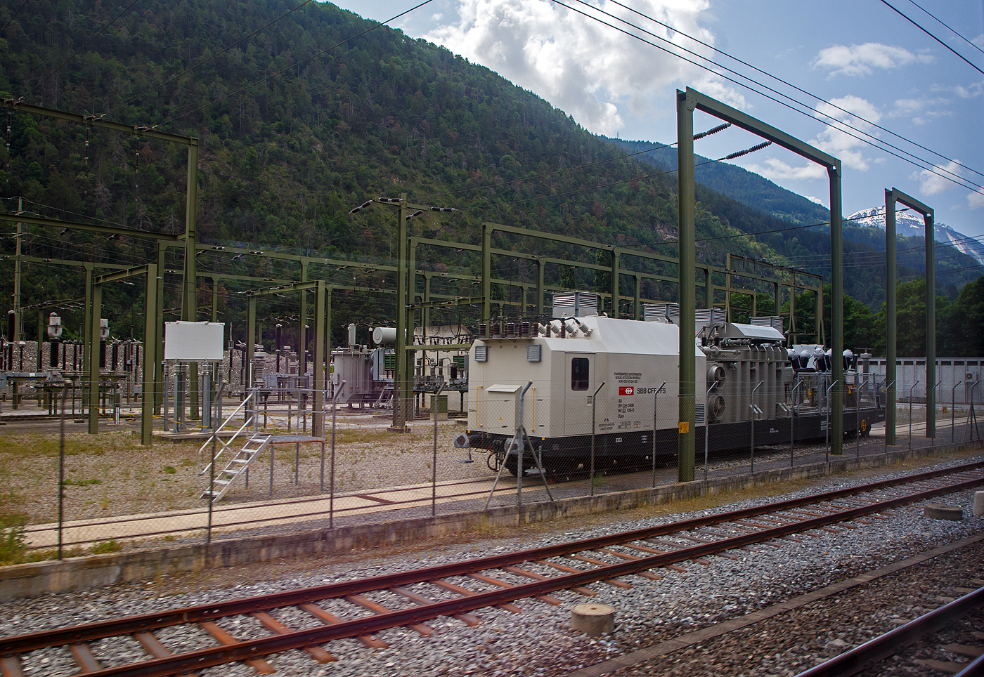 Achtachsiges SBB Fahrbares Unterwerk, Sous-Station Mobile, KW-DU H7.84/92, Xaa 80 85 94 03 106-0 CH-SBB, der SBB - Schweizerischen Bundesbahnen, ex Xa 30 85 98 00 206-x CH-SBB, am 28.05.2023 bei Gampel-Steg/Wallis (Industriezone Schnydrigen), aufgenommen aus einem Zug heraus. 

Ein fahrbares Unterwerk ist ein Umspannwagen bzw. Transformatorwagen mit Hochspannungsschaltanlage. Fahrbare Unterwerke werden insbesondere bei den SBB häufig eingesetzt. Die SBB betreiben ein eigenes Hochspannungsnetz mit einer Frequenz von 16,7 Hertz.

Von dieser dritten Serie (Xa 30 85 98 00 206 bis 209, ab 1991 umgezeichnet in Xaa 80 85 94 03 106 bis 109) Fahrbares Unterwerk wurden 4 Wagen 1985  von der Ferriere Cattaneo SA gebaut. Die 140 t und ca. 24,5 m langen Wagen laufen auf zwei vierachsigen Tiefladewagen-Drehgestelle SBB TLW 52, diese haben einern Achsstand 3 x 1.500 mm, der Laufraddurchmesser beträgt 850 mm (neu).