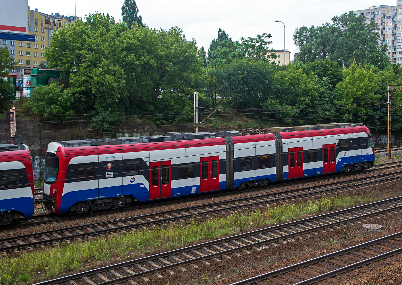 Als Detailbild der einzelne Halbzug EN97 – 011a ein Pesa 33WE der WKD (Warszawska Kolej Dojazdowa), er hat am 26 Juni 2017 gerade, gekuppelt mit dem EN97 – 011b, den Bahnhof Warszawa Ochota verlassen.

Für die Umsetzung der Erhöhung der FahrIeitungsspannung bei der WKD von 600 auf 3.000 Volt Gleichstrom lieferte PESA in 2011/12 insgesamt 14 Zweisystem-Einheiten der neuen Baureihe EN97. Technisch gesehen sind die EN97Halbzüge mit nur je einem Führerstand und am führerstandslosen Ende aneinander gekuppelt.

Bei den Halbzügen sind die beiden Endwagenkasten mit ihren Triebdrehgestellen auf einem kurzen Mittelteil aufgesattelt, welches auf einem Laufdrehgestell ruht. Jedes Drei-Wagen-Modul (Halbzug) besitzt einen geräumigen Führerstand an einem Ende des Fahrzeugs, während ein zusätzliches Bedienfeld am anderen Ende das Führen des Halbzuges erleichtert, wenn die Einheiten getrennt werden. Bei Rangierfahrten kann so ein einzelner Halbzug in jeder Richtung mit geringer Geschwindigkeit bewegt werden.  

Acht über lGBT-Umrichter angesteuerte Drehstrom-Asynchronmotoren gewährleisten eine entsprechende Beschleunigung, wobei die Drehstromtraktionsausrüstung im Wesentlichen auf dem Dach angeordnet ist. Die Fahrzeuge können bis zu 500 Personen befördern. Die zweistufige Federung besitzt Luftfedern als Sekundärfederung zur Komfort-Verbesserung. Klimatisierte Führerstände und Innenräume sowie die großzügig ausgeführten Fahrgasträume bieten komfortable Reisebedingungen. Acht breite Türen mit ihren niedrigen Einstiegsbereichen (500 mm über SOK) erleichtern das Ein-und Aussteigen. Visuelle und akustische Fahrgastinformation, Videoüberwachung innen und außen, sowie vandalismusresistente, doch durchaus dem Auge gefällige Sitze sorgen für eine komfortable und sichere Fahrt. 

Zwar bilden die EN97 heute das Rückgrat der WKD, doch nicht ganz ohne Probleme. So erfordern die Laufflächen der Räder ein häufiges Abdrehen. Dies führt zu längeren Ausfallzeiten, da die WKD keine eigene Radsatzdrehbank besitzt.

TECHNISCHE DATEN (Vollzug):
Gebaute Stückzahl: 14
Baujahre: 2011 bis 2012
Spurweite: 1.435 mm
Achsfolge: Bo’2’Bo’+Bo’2’Bo’
Länge über Kupplung: 60.000 mm
Drehzapfenabstand:
Achsabstand im Triebdrehgestell: 2.300 mm
Achsabstand im Laufdrehgestell: 2.100 mm
Lauf- und Treibraddurchmesser (neu): 850 mm
Dienstgewicht: 101,5 t
Dauerleistung: 8 x 180 kW = 1.440 kW
Höchstgeschwindigkeit: 80 km/h
Startbeschleunigung:  1,2 m/s²
Stromsystem: 600 V DC / 3000 V DC
Sitzplätze: 124
Motorentyp: TME42-26-4
