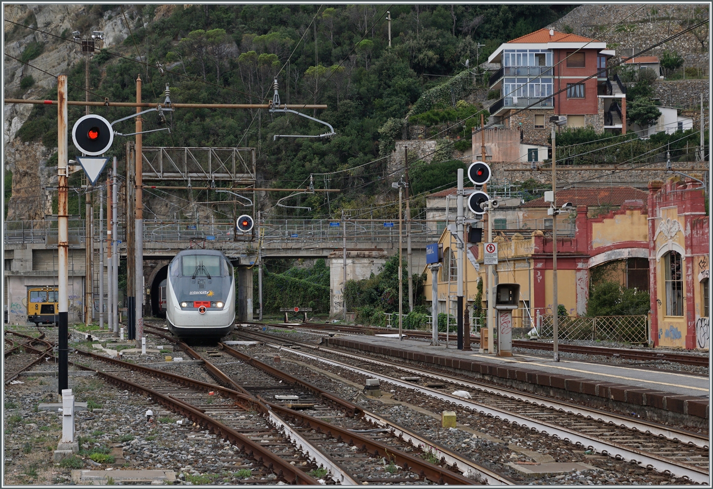 Als vor wenigen Jahren bei Cervia eine der sch�nsten Streckenabschnitte der Strecke Genova - Ventimiglia durch eine Tunnel-Variante ersetzt wurden, reiste im Vorfeld nochmals zahlreiche Fotografen an. Die 1868 er�ffnete Strecken Genova - Savona. bzw. 1972 in Betrieb genommene Fortsetzung Savona Ventimiglia f�hrte vielerorts durch eine schwierige Topografie und wurde gr�sstenteils dem Meer entlang und durch die Ortschaften trassiert. Die Strecke wurde est mit Drehstrom elektrifiziert, sp�ter als V 25 000/ 50 Hz projektiert, um dann 1964/1967 schlussendlich mit dem FS Gleichstrom 3000 versorgt zu werden. Doch bereits um diese Zeit gen�gte die Einspur-Strecke dem Meer entlang nicht mehr dem zunehmenden Verkehr, so das Ende der 1960er im Raum Genova erste Neubau Trassierungen erfolgen. 1977 folgte mit dem Abschnitt Varazzo - Finale Ligure ein erste l�nger Neubauabschnitt. Mit der Zeit folgten weiter westlich weitere, doch in Finale Ligure treffen sich nun der erste Neubauabschnitt mit dem letzten noch urspr�nglichen Streckenabschnitt. Dies ist auch das Motiv der Bilder von Finalie Ligure, hier verl�sst der FS Trenitalia IC 631 die einspurige, 1136 Meter lange  Galleria Caprazoppa . Fotostandpunkt: Bahnsteigende) 16. September 2023