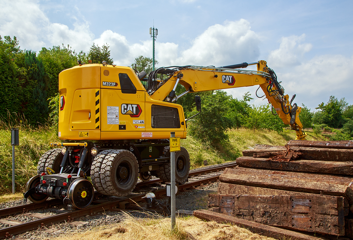 Bei dem Rangierbahnhof der KSW (Kreisbahn Siegen-Wittgenstein) in Herdorf der Betriebsstätte FGE -Freien Grunder Eisenbahn (KSW NE447 / DB-Nr. 9275) wurden und wird der Unterbau der Gleise erneuert. Der Umbau erfolgt ohne große Einschränkungen des Tagesablaufes. 

Hier stapelt der Caterpillar CAT M323F Zweiwegebagger mit hydrostatischem Schienenradantrieb (Serien-Nr. RH600 189), Kleinwagen Nr. D-ZBM 99 80 9902 521-0 der ZEPPELIN Baumaschinen GmbH (Garching), wohl ein Mietbagger, am 26.06.2023 bei der Talbahnstraße Schellen.

Hier sieht man deutlich das der Fahrantrieb auf der Schiene, nicht wie bei vielen ZW-Baggern üblich, durch die Straßenreifen sondern mittels dem hydrostatischem Schienenradantrieb erfolgt (der Bagger bzw. das Straßenfahrwerk ist über die Schienen angehoben).

Der Zweiwegebagger wurde 2022 unter der Fabrik-Nr. CAT M323FERH600189 gebaut.

Schienenradantrieb
Der CAT Zweiwegebagger mit hydrostatischem Schienenradantrieb (vom französischen Spezialmaschinenbauer UNAC) ist konsequent für den Einsatz auf der Schiene entwickelt. Mit seinem kurzen Heck, dem innovativen Radantrieb und Bremssystem für alle Gleisräder und dem ausgefeilten, aber einfach bedienbaren Kontrollsystem erschließt der Cat M323F den Anwendern entscheidende Vorteile.Anders als bei den bisher üblichen Zweiwegebaggern bewegt sich die Maschine auf der Schiene damit nicht abgesenkt auf den herkömmlichen Rädern voran, sondern ohne Bodenkontakt auf den Schienenrädern selbst. Die hohe Bodenfreiheit gewährleistet dabei, dass die Sicherheitseinrichtungen im Gleisbett beim Fahren nicht beschädigt werden. Mit dem Bremssystem im Ölbad an beiden Achsen und den Scheibenbremsen für alle Gleisräder gewährleistet der Cat M323F sicheren Vortrieb und kraftvolle Beschleunigung bis auf 20 km/h.

Klassische Zweiwegebagger sind vielfach noch mit Reibradantrieb ausgestattet. Die Reifen des Baggers werden dabei auf die Schienen oder Rolle gepresst und übertragen so die Antriebs- und Bremskräfte. Die Nachteile: hoher einseitiger Reifenverschleiß und oft Beschädigungen von Sicherheitseinrichtungen im Gleisbett.

Kurzheckbauweise
Durch den kompakten Aufbau und die geringe Heckausladung von nur
1.566 mm kann der Schienenverkehr auf dem Nachbargleis problemlos
weiterlaufen. Auch mit dem optional verfügbaren Zusatzkontergewicht bleibt der kurze Heckschwenkradius unverändert. Trotz des kompakten Hecks bietet die Maschine mit dem robusten Verstellausleger auch auf dem Gleis viel Reichweite und hohes Hubvermögen.

Die Konstruktionsweise sowie das bis zu 7,5 t schwere Kontergewicht stellen dabei sicher, dass die Maschine dennoch über eine hohe Standsicherheit, Reichweite und Hubvermögen verfügt.

Motor
Angetrieben wird der neue CAT Zweiwegebagger von einem Vierzylinder-Viertakt-Reihendieselmotor mit zwei Turboladern (Reihenturboaufladung) und Ladeluftkühlung (TTA) vom Typ CAT C4.4 ACERT TTA, Emissionen EPA Tier 4 Final (USA) bzw. Stufe V (EU) und Dieselpartikelfilter.

Motordaten:
Leistung: 129,4 kW (173 PS)
Maximales Drehmoment: 750 Nm bei 1400 U/min
Nenndrehzahl 2.200 U/min
Bohrung x Hub: 105 x 127 mm
Motorhubraum: 4,4 l
Verdichtungsverhältnis: 16,5 :1
Ansaugsystem: Turboladern und Ladeluftkühlung (TTA)
Verbrennungsverfahren: Direkteinspritzung
Abmessung: 845 x 742 x 868 mm
Gewicht (trocken) 420 kg

Der C4.4-Motor kann entweder mit extrem schwefelarmem Dieselkraftstoff oder mit B20-Biodiesel betrieben werden und erfüllt die Emissionsnormen der EU-Stufe IV. Die Leerlaufabschaltung, die automatische Motordrehzahlregelung und das bedarfsgesteuerte Kühlsystem verringern den Kraftstoffverbrauch.

TECHNISCHE DATEN:
Spurweite: 1.435 mm (Normalspur)
Eigengewicht: 23.400 kg
Höchstgeschwindigkeit: 19,9 km/h (20 km/h auf Straße)
Zul. Anhängelast: 220 t
Schienenbodenfreiheit: 195 mm
Straßenbodenfreiheit: 360 mm
Zugkraft auf Straße: 104 kN
Zugkraft auf Schiene: 45 kN

Quellen: CAT, ZEPPELIN und Anschriften
