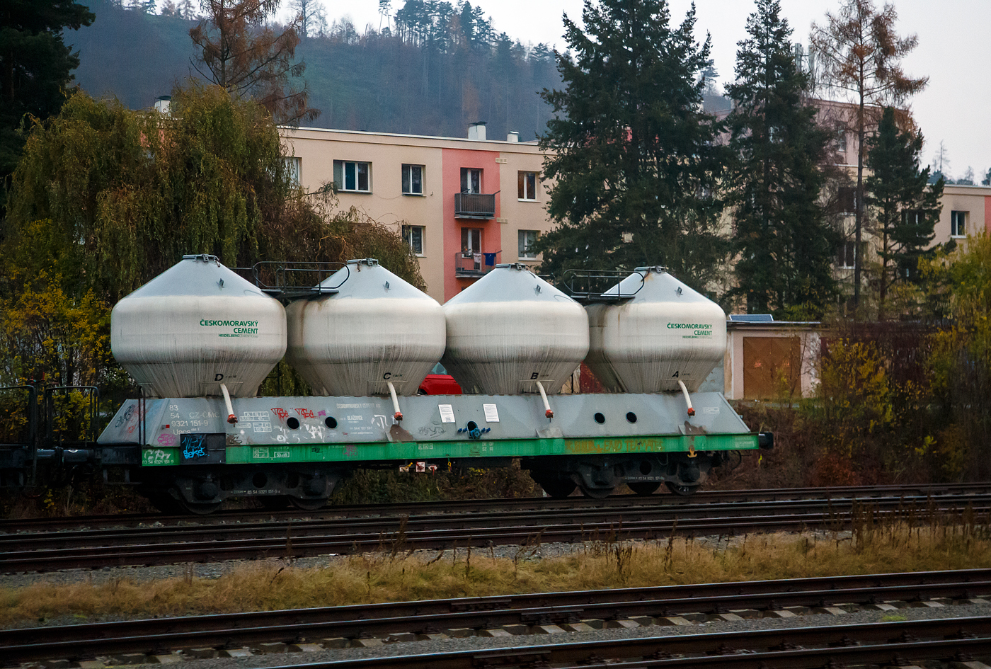 Der 4-achsiger Drehgestell-Silo-/Zementwagen 83 54 9321 181-9 CZ-CMC, der Gattung Uacs 451.1,der tschechischen Českomoravský cement, a.s., gehört zur HeidelbergCement Group, abgestellt am 24.11.2022 bei Karlštejn (deutsch Karlstein, zum Bezirk Beroun). Aufnahme aus dem Zug heraus. Die vier Behälter haben jeweils ein Ladevolumen von 13 m³ = 52 m³ Gesamtvolumen. Das max. Ladegewicht beträgt 47,6 t ab Streckenklasse B bei Lastgrenze S (100 km/h), in CZ auch 56,6 t ab Streckenklasse C bis 90 km/h möglich.

Die Bedeutung der Gattungs- und Kennbuchstaben (hier Uacs):
U - Sonderwagen 
a - mit vier Radsätzen
c - mit Entladung unter Druck
s - Höchstgeschwindigkeit 100 km/h (beladen)
