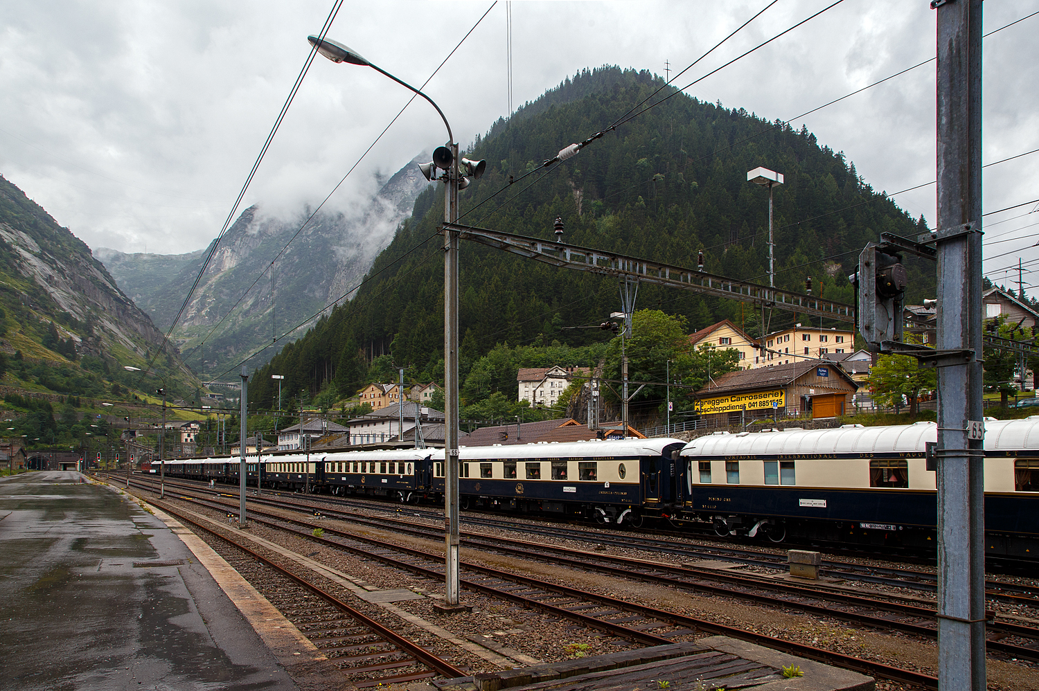 Der „König der Züge“ der Orient-Express, oder für mich der Zug der Züge. Wir hatten am Vortag bei der Ankunft im Hotel davon erfahren, das der VSOE am nächsten Tag durchfährt, so haben wir unsere Weiterfahrt über den Gotthardbahn nach Locarno und weiter mit der Centovallibahn nach Domodossola, etwas verschoben. 

Der VSOE - Venice Simplon-Orient-Express von Amsterdam über Brüssel und Paris nach Venedig hat am 02. August 2019 leider bei Regen, gezogen von einer SBB Re 8/8 (Doppeltraktion der Re 4/4 11194 und Re 4/4 11156), den Bahnhof Göschenen erreicht und steht so nun vor dem Nordportal des 15 km langen Gotthard-Scheiteltunnels. Hier fährt er aber nicht, wie es im Namen steht, durch den Simplon, sondern über den Gotthard. Der Orient-Express bestand aus einem Zug mit 18 Wagen, meinst waren es modernisierte historische ehemalige CIWL-Wagen. Ob es auch einen „Mord im Orient-Express“ gab? Das kann ich nicht sagen, hatte aber gehört das man wohl einen im Zug nachspielte.

Wer kennt den Film nicht „Mord im Orient-Express“ nach dem Roman von Agatha Christie aus dem Jahr 1934. Wo der berühmte belgische Privatdetektiv Hercule Poirot den Mord an einem reichen Amerikaner untersucht, der im berühmtesten Zug der Welt reist.

Der Venice Simplon-Orient-Express (abgekürzt VSOE), verkehrt seit 1982. Der Luxuszug wird von der Firma Belmond Ltd. betrieben. Der Zug besteht aus historischen Wagen der Compagnie Internationale des Wagons-Lits (CIWL). Es werden Fahrten in Form von Schienenkreuzfahrten über verschiedene europäische Strecken angeboten, darunter auch die historischen Strecken des früheren Simplon-Orient-Express und des Orient-Express.
