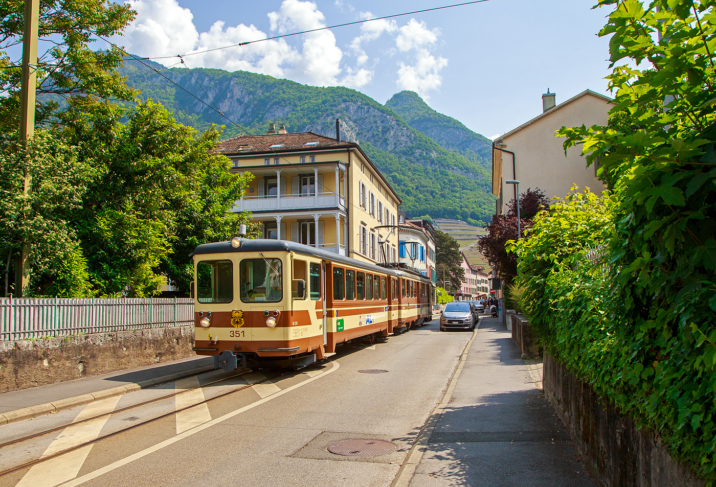 Der AL Regionalzug von Leysin nach Aigle fährt am 28. Mai 2023 (hier als Straßenbahn) durch Altstadt und erreicht bald den Bahnhof Aigle. Der Zug besteht aus dem führenden Steuerwagen AL Bt 351 „Aigle“  und dem Triebwagen AL BDeh 4/4 302 „Leysin“, beide sind noch im ursprünglichen Anstrich der AL (es sind auch die einzigen). 

In Aigle (Waadt) gibt es gleich drei Schmalspurbahnen, die seit 1999 in die Transports Publics du Chablais (TPC) fusioniert worden sind, so machten wir auf unserer Rückreise hier mal einen kurzen Zwischenhalt. Die Schmalspurbahnen sind die Aigle–Ollon–Monthey–Champéry-Bahn (AOMC), die Aigle–Sépey–Diablerets-Bahn (ASD), seit dem 22. Dezember 1913 und die Aigle–Leysin-Bahn (AL).

Die Chemin de fer Aigle–Leysin (AL), deutsch Aigle-Leysin-Bahn, war eine Eisenbahngesellschaft im Schweizer Kanton Waadt. Ihre von 1900 bis 1916 eröffnete 6,2 Kilometer lange Strecke führt von Aigle im Rhonetal hinauf nach Leysin-Grand Hôtel. Die gemischte Zahnradbahn in der Spurweite 1.000 mm (Meterspur) mit dem System Abt wird seit der Betriebsaufnahme elektrisch betrieben. Im Jahr 1999 fusionierte die AL zu den Transports Publics du Chablais (TPC).

Die Bahnstrecke Aigle–Leysin hat ihren Ausgangspunkt vor dem SBB-Bahnhof und führt als Straßenbahn auf der Rue de la Gare (Bahnhofstraße), der Avenue des Ormonts und über die Grande Eau zum Kopfbahnhof Aigle-Dépôt. Dort ändern die Züge die Fahrtrichtung, damit das Triebfahrzeug für die anschließende Bergfahrt am Ende des Zuges eingereiht ist. 

Im Keilbahnhof Aigle-Dépôt beginnt der 5,3 Kilometer lange und bis zu 230 Promille steile Zahnstangenabschnitt. Zunächst führt er durch die Rebberge und bietet den Fahrgästen einen Ausblick auf das Rhonetal. Bei der Haltestelle Pont-de-Drapel wechselt die Vegetation und das Trassee befindet sich nun im Wald. Der Zug erreicht eine Waldlichtung mit dem Bahnhof Rennaz (Leysin), wo er sich in der Regel mit dem Gegenzug kreuzt. Die Strecke führt weiter durch Wald und den 154 Meter langen Tunnel Rennaz. Ab rund 1.200 Meter über Meer fährt die Zahnradbahn durch Weiden und erreicht nach kurzer Zeit den Bahnhof Leysin-Village (Leysin-Dorf). Hier beginnt der Doppelspurabschnitt mit der 128 Meter langen Brücke Leysin nach Leysin-Feydey. Nach dem 287 Meter langen Kehrtunnel Leysin erreicht die Strecke, immer noch mit Zahnstange versehen, den Endpunkt Leysin-Grand Hôtel.


Die Triebwagen und Steuerwagen BDeh 4/4 301–302 und Bt 351–352 wurden 1966 von SIG/SAAS gebaut. 

TECHNISCHE DATEN:
Spurweite: 1.000 mm
Fahrleitungsspannung: 1.500 V =

Triebwagen: BDeh 4/4 301-302
Zahnstangensystem: Abt
Achsfolge: Bo'zz Bo'zz
Länge über Puffer: 16.100 mm
Drehzapfenanstand: 9.540 mm
Achsabstand im Drehgestell: 2.460 mm
Leistung: 596 kW (808 PS)
Treibraddurchmesser: 840 mm (neu)
Zahnrad-Teilkreisdurchmesser: 650
Höchstgeschwindigkeit: 40 km/h
Übersetzung: 1:12,2
Gewicht: 33.0 t
Sitzplätze: 48
Max. Ladegewicht: 1,5 t

Steuerwagen Bt 351–352
Anzahl der Achsen: 4
Gewicht: 11.0 t
Sitzplätze: 48
