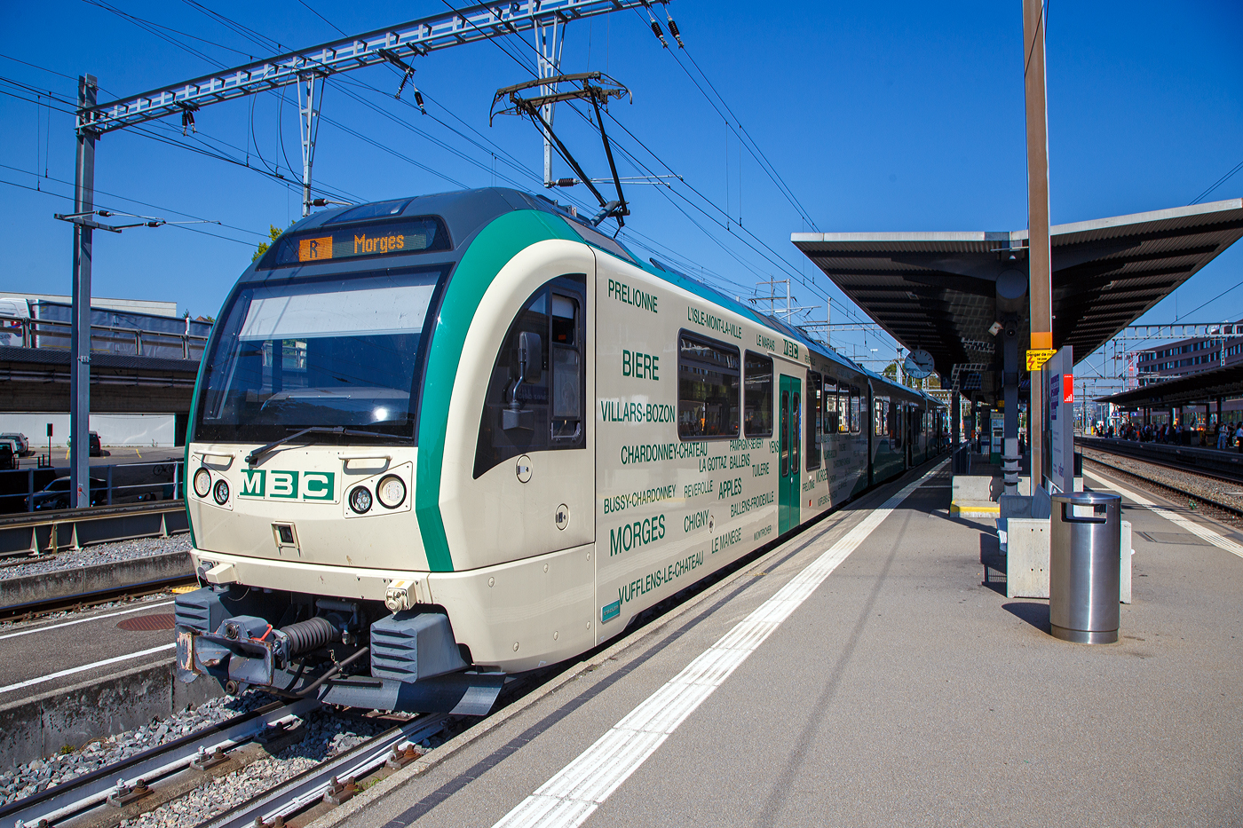 Der BAM/MBC dreiteilige elektrische Stadler Westschweizer Meterspurtriebzug, in der Komposition Be 4/4 38 + B4 2068+ Be 4/4 35, hat am 07 September 2023, als Regionalzug von Bière, den Bahnhof Morges erreicht.

Die MBC (ex BAM) hatte 2013 bei Stadler Rail 4 Fahrzeuge (dreiteilige elektrische Triebzüge Be4/4 + B + Be4/4) als Ersatz für bestehendes Rollmaterial bestellt, das das Ende seiner Lebensdauer erreicht hat. Mit dem neuen Rollmaterial konnte im Dezember 2015 der Halbstundentakt eingeführt werden. Damit wurde der Anschluss an die RE- und IR-Züge zwischen Lausanne und Genf geschaffen, die den Bahnhof von Morges im Halbstundentakt anfahren. Die Fahrzeuge mit modernem, dynamischem Design sind einladend und komfortabel. Sie entsprechen auch in technologischer Hinsicht den Betriebsbedingungen auf dieser Strecke und werden den hohen Erwartungen der Kunden gerecht. Gleichzeitig wurden Vereinfachungen bei der Instandhaltung ermöglicht. Den Fahrgästen stehen total 168 Sitzplätze zur Verfügung. Die Züge sind für eine Höchstgeschwindigkeit von 100 km/h ausgelegt.

Technische Merkmale:
• Wagenkasten aus Aluminium-Strangpressprofilen
• Luftgefederte Trieb- und Laufdrehgestelle
• Endtriebwagen können auch mit angepassten älteren Steuerwagen verkehren
• Multifunktionsabteile bei allen Einstiegen
• 3 Einstiegtüren pro Seite für schnellen Fahrgastwechsel
• Redundante Antriebsausrüstung bestehend aus 2 Antriebssträngen mit wassergekühlten IGBT-Stromrichtern
• Redundante Fahrzeugleittechnik mit Zugbus und Diagnoserechner

TECHNISCHE DATEN:
In der Komposition Be 4/4 + B + Be 4/4
Anzahl Fahrzeuge: 4 (Züge)
Hersteller: 	Stadler Bussnang AG
Baujahr: 2015
Einsatzgebiet: Morges – Apples – Bières – L’Isle
Spurweite: 1.000 mm (Meterspur)
Achsfolge: Bo‘Bo’ + 2’2’ + Bo‘Bo’
Länge über Kupplung: 60.310 mm (20.155 + 20.000 + 20.155 mm)
Fahrzeugbreite: 2.650 mm
Fahrzeughöhe: 4.020 mm
Achsabstand im Motordrehgestell: 2.000 mm
Achsabstand im Laufdrehgestell: 1.800 mm
Triebraddurchmesser:  810 mm (neu)
Laufraddurchmesser: 770 mm (neu)
Eigengewicht: 117 t
Höchstgeschwindigkeit: 100 km/h
Dauerleistung am Rad: 2 x 1.020 kW
Max. Leistung am Rad: 2 x 1.400 kW
Anfahrzugskraft: 300 kN
Anzahl der Fahrmotoren: 2 x 4
Anfahrbeschleunigung: 1.2 m/s²
Bremsleistung: 1.33 m/s²
Fahrleitungsspannung: 15.000 V, 16.7 Hz ~
Sitzplätze: 154 (2. Klasse) 
Klappsitze: 14
Stehplätze (bei 6 Pers./m²): 208
Fußbodenhöhe Niederflur am Einstieg: 380/ 480 mm
Fußbodenhöhe Hochflur: 1.000 /1.100 mm
Einstiegbreite: 1400 mm
Minimaler Kurvenradius: R 80 m (auf der Strecke)
Kupplungstyp: +GF+ 

Wie bei Stadler-Fahrzeugen üblich nimmt die Sitzanordnung auf die Fensterteilung Rücksicht, um den Fahrgästen einen ungehinderten Ausblicken zu ermöglichen. Die Fußbodenhöhe beträgt im Niederflurbereich einheitlich 480 mm. Im Türbereich senkt sie sich über eine Rampe auf 380 mm.

Allgemein:
Die STADLER Westschweizer Meterspurzüge aus den Jahren 2015/16 sind elektrische Niederflur-Triebzüge und -Triebwagen des Herstellers Stadler Rail, die bei sechs Westschweizer Privatbahnen (MBC / Travys / TPF / NStCM / MOB / CJ) mit unterschiedlichen Achsfolgen unter verschiedenen Stromsystemen im Einsatz stehen. Zudem erhielt die Appenzeller Bahnen (AB), die bekanntlich in der Deutschschweiz (Nordostschweiz) liegt, 2018 fünf ABe 4/12 die weitgehend den Meterspurzügen der TPF entsprechen.

Ausgangslage:
Für die vorhanden Pendelzüge Be 4/4 11–13 + Bt 51–53 aus dem Jahr 1981beschafften die Transports de la région Morges–Bière–Cossonay (MBC, ex BAM) bereits 2010 drei zu den vorhandenen Pendelzügen passende vierachsige Niederflurzwischenwagen B 2065–2067. Schon bei der Bestellung war vorgesehen, sie später mit passenden Triebwagen zu ergänzen, um komplett neue Züge zu erhalten. So bildeten diese den Ausgangspunkt für die Konstruktion.

2009 bestellte die Nyon-Saint-Cergue-Morez-Bahn (NStCM) bei Stadler vier zweiteilige Triebzüge ABe 4/8. Die NStCM hatte zunächst Interesse an Zügen in der Bauart der RBe 4/8 der Lausanne–Echallens–Bercher-Bahn. Der Kanton Waadt verweigerte jedoch die Finanzierung der Kleinserie und forderte aus Kostengründen eine gemeinsame Bestellung mit anderen Bahnen. Bei den Deutschschweizer Meterspurbahnen wusste man nichts von der Bestellung. Indessen verzeichneten mehrere Meterspurbahnen in der Romandie starke Nachfragesteigerungen, so dass der Kanton Waadt eine Kapazitätssteigerung und Erneuerung der auf seinem Gebiet verkehrenden Privatbahnen beschloss. Daraufhin schrieben die drei Waadtländer Meterspurbahnen MBC, Travys und Montreux-Berner Oberland-Bahn (MOB) zusammen mit den Transports publics fribourgeois (TPF) die Lieferung von 17 zwei- bzw. dreiteiligen Triebzügen aus. Trotz der Konkurrenz des Bombardier-Konzerns, der im waadtländischen Villeneuve ein Werk betreibt, erhielt Stadler Bussnang den Auftrag im Wert von 151 Millionen Franken. Damit hat der Thurgauer Hersteller bei den Schweizer Meterspurfahrzeugen seinen Konkurrenten aus dem Markt gedrängt, was ihm gute Preise bringen wird. Mit der gemeinsamen Bestellung ließen sich 28 Millionen Franken einsparen. Die NStCM schloss sich der Bestellung mit vier zweiteiligen Zügen im Wert von 66 Millionen an. Nachträglich bestellten die Chemins de fer du Jura (CJ) fünf Einteiler. Ursprünglich wollten die CJ komplette Triebzüge beschaffen, die bereitgestandenen Mittel hätten aber nur für drei Züge ausgereicht.

Die Anforderungen der Kunden sind unterschiedlich. MBC und Travys fahren mit 15.000 Volt Wechselstrom, die anderen Bahnen mit Gleichstrom. Die Strecken von MBC, Travys und MOB sind mit ihren starken Steigungen anspruchsvoll. Die MBC bestellten einen dreiteiligen und drei zweiteilige Züge, wobei die Zweiteiler mit den bereits vorhandenen Niederflurzwischenwagen zu Dreiteilern ergänzt wurden. Die Zugkraft ist so ausgelegt, dass sie für den Militärverkehr bis zu vier zusätzliche Personenwagen nach Bière befördern können. Mit den drei dreiteiligen Zügen stehen Travys zusammen mit den beiden GTW ABe 2/6 modernes Rollmaterial für die Strecke Yverdon–Ste-Croix (YSteC) zur Verfügung. Die vier leistungsstarken Zweiteiler der MOB werden wie die Allegra der Rhätischen Bahn (RhB) zur Traktion von längeren Zügen mit bis zu neun Reisezugwagen eingesetzt. Die TPF nutzen die neuen Fahrzeuge, um auf ihrem Schmalspurnetz die erste Wagenklasse einzuführen. Die als Dreiteiler abgelieferten Züge können zur Anpassung an die Verkehrsnachfrage als zwei- und vierteilige Kompositionen formiert werden. Sie lösten die BDe 4/4 und Be 4/4 aus den 1970er-Jahren ab, die nun den ausgeprägten Schülerverkehrs abdecken. Mit ihren Be 4/4 651–655 sowie fünf modernisierten Steuerwagen ABt 711–715 aus den Jahren 1985/86 und drei Mittelwagen können die CJ den Regelverkehr seit 2016 mit behindertengerechten Kompositionen abdecken. Sie verkehren vorerst auf der Strecke Tavannes–Le Noirmont. 

Die MBC und MOB vereinbarten Optionen über je eine zusätzliche Komposition, die TPF über vier und die NStCM über fünf, wobei die Bestellung der NStCM für das Jahr 2018 geplant war. Im Dezember 2019 bestellte die NStCM sechs weitere Züge, die 2022 abgeliefert wurden. sollten. Wie erst im Dezember 2022 bekannt wurde, bestellte die TPF im Jahr 2020 drei weitere Züge und im Juni 2021 noch einen zusätzlicher Zug bestehend aus ABe 2/4 – B – Be 2/4 mit den Nummern 107–110 bei Stadler. Die Lieferung der ersten drei Züge soll im November 2023 erfolgen, der vierte Zug im Februar 2024.

Quelle: Anschriften am Fahrzeug und Wikipedia
