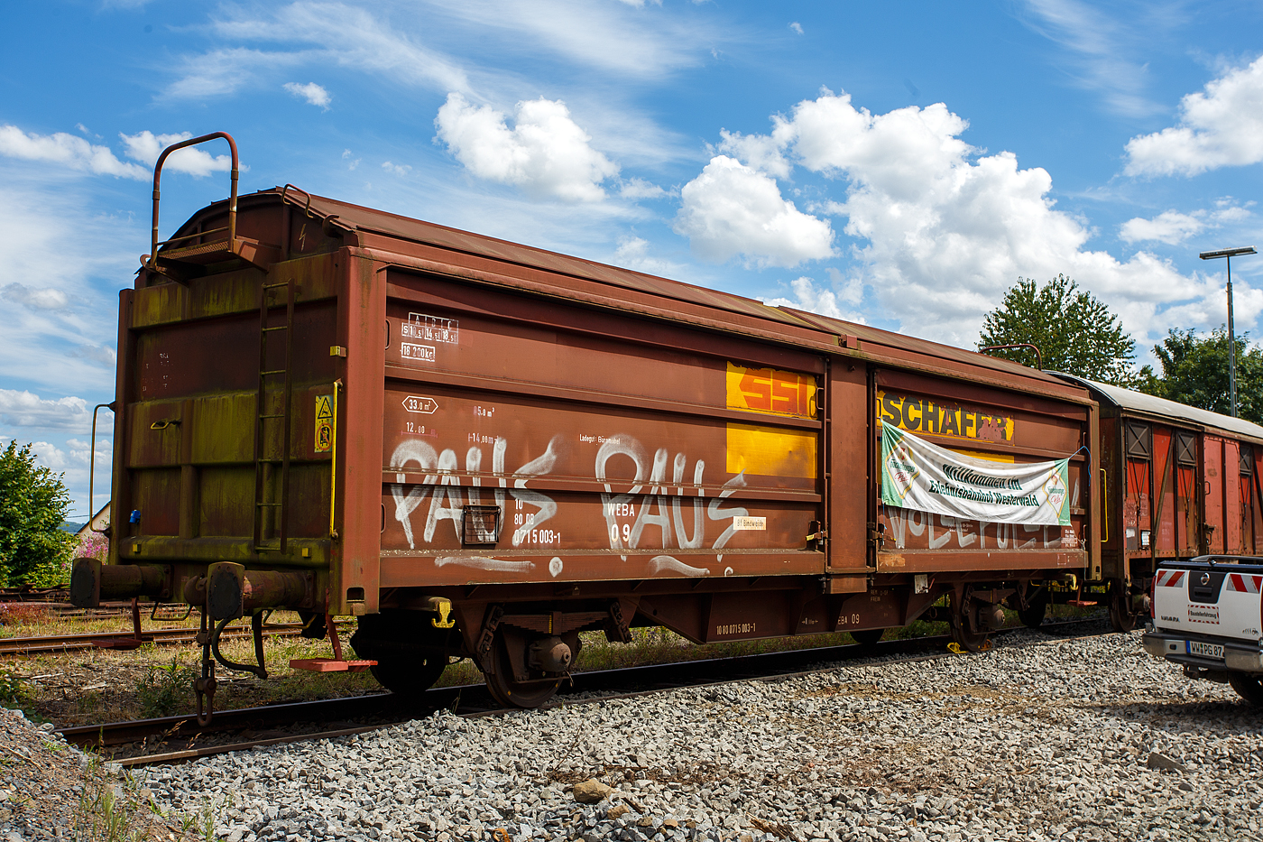 Der gedeckte zweiachsige Schiebewand-/Schiebedachwagen WEBA 09 - 10 80 0715 003-1 D-WEBA (ex 10 80 0715 003-1 D-DB) der Gattung Tbis 869 - Bauform A (für Büromöbel der SSI Schaefer Shop GmbH) ehemals der WEBA (Westerwaldbahn des Kreises Altenkirchen GmbH), ausgestellt am 07 Juli 2024 beim Erlebnisbahnhof Westerwald der Westerwälder Eisenbahnfreunde 44 508 e. V. in Westerburg, hier war Lokschuppenfest.

Beschreibung:
Die Beschaffung erster Hubschiebedachwagen begann bereits 1949. Die Wagen verfügten über ein zweiteiliges Dach, von denen ein Teil über das andere geschoben werden konnte. In der Mitte des Wagens war ein der Dachform angepasstes Querjoch angebracht, um einerseits die Spur der Dachlaufwerke halten zu können, andererseits das Dach dicht verschließen zu können. Betätigt wurde das Dach durch ein an den Kopfendenden angebrachte hoch liegende Bühne, die über Leitern erreicht wurden.

Ab 1966 wurden von der DB bei der Waggonunion Siegen (eigentlich Dreis-Tiefenbach, zuvor Siegener Eisenbahnbedarf A.G.) die ersten Wagen der Gattung Tbis 869 der Bauform A beschafft. Bei dieser Bauform konnte das Dach auch nur von einer kleinen oben liegenden Bühne an den Stirnwänden geöffnet werden. Zwei Jahre später wurde die Bauform B dieser Gattung gefertigt. Hierbei war es nun möglich das Dach mittels Handräder an einer Stirnseite der Waggons zu öffnen. Es war nun nicht mehr nötig auf das Dach zu steigen und verminderte somit auch die Unfallgefahr.

Eingesetzt wurden diese Waggons für den Transport von großen nässeempfindlichen Stückgütern (bei diesem Wagen waren es später Büromöbel), durch das öffnungsfähige Dach könnte die Ladung auch mittels Kranen schnell be- und entladen werden. Von den ca. 2.000 beschafften Fahrzeugen gelangten noch gut 1.400 zur DB AG, dort wurden sie aber zügig ausgemustert und durch neuere Bauarten ersetzt. 

TECHNISCHE DATEN:
Spurweite: 1.435 mm (Normalspur)
Anzahl der Achsen: 2
Länge über Puffer :14.000 mm
Achsabstand: 8.000 mm
Eigengewicht: 18.400 kg
Ladelänge:12.800 mm
Ladefläche: 33,0 m²
Rauminhalt: 85,0 m³
Seitenwand-Türöffnung (B × H): 5.660 × 2.100 mm
Lichte Öffnung bei geöffnetem Dach: 6.000 × 2.530 mm
Fußbodenhöhe über SO: 1.200 mm
Höchstgeschwindigkeit: 100  km/h 
Maximales Ladegewicht: 18,5 t (Streckenklasse C oder höher)
Kleinster bef. Gleisbogenradius:  35 m
Bremse: Frein O-GP 
Intern. Verwendungsfähigkeit: RIV (ursprünglich)
