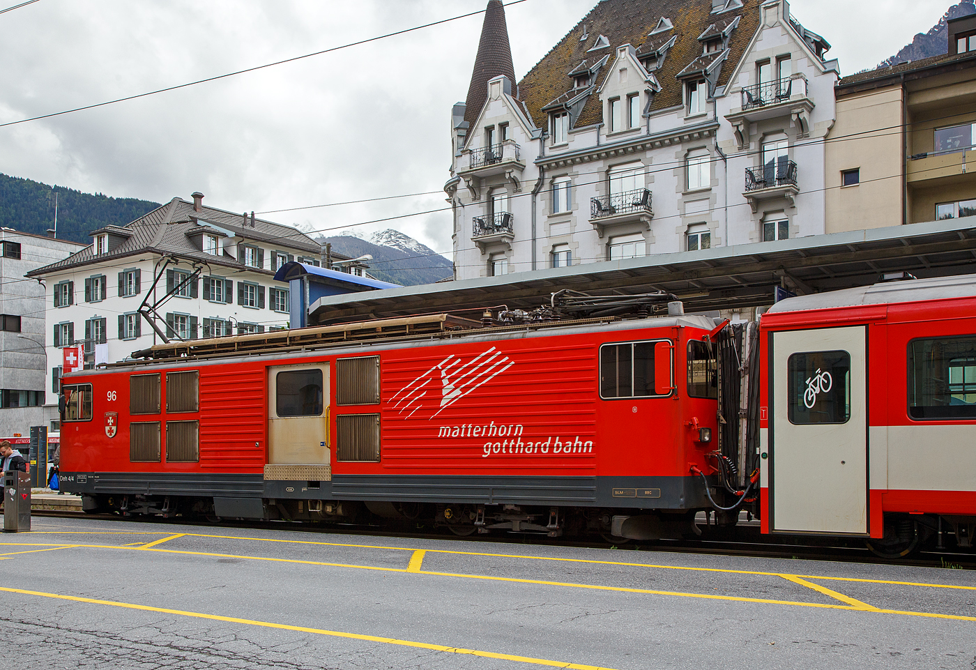 Der Gepäcktriebwagen Deh 4/4 II - 96  Münster   der Matterhorn-Gotthard-Bahn (MGB), ex FO 96  Münster   (Furka-Oberalp-Bahn), am 25.05.2023 mit einen Regionalzug von Andermatt nach Visp im Bahnhof (Vorplatz) Brig.

Der Elektrischer Zahnradtriebwagen wurde 1984 von SLM (mechanischer Teil, Lokomotivkasten) und BBC (elektrische Ausrüstung) gebaut.

Die vier 1980 bei der Furka- Oberalp-Bahn in Betrieb genommenen Gepäcktriebwagen sind für Adhäsions- und Zahnstangenstrecken konzipiert. Zwei weitere Einheiten wurden 1982 in Auftrag gegeben. Sie werden auf dem ganzen Streckennetz – maximale Steigung 179%o - als Triebfahrzeuge für Züge mit vier bis fünf Wagen eingesetzt. Der biege- und verwindungssteife, extrem leichte Kasten wurde in Stahl ausgeführt und die hohe Steifigkeit durch Strukturgebung erzielt. Dem leichten Innenausbau und der ergonomischen Führerstandgestaltung wurde ebenfalls besondere Aufmerksamkeit geschenkt.

Die Drehgestelle, die durch tiefliegende Drehzapfen über Traversen  mit dem Kasten verbunden sind, enthalten je zwei Antriebsmotoren. Die Betriebsverhältnisse erfordern drei unabhängige Bremssysteme.

Die ehemaligen Deh 4/4 I und II der FO (Furka-Oberalp-Bahn) werden im Einsatz nicht unterschieden, wenn nötig, dann anhand der Seriennummern 2.., 5.. und 9... Wobei sie sich optisch und technisch schon etwas unterscheiden. Sie werden hauptsächlich zusammen mit zwei Mittelwagen und einem Steuerwagen als fest gekuppelte Pendelzüge eingesetzt. Zwischen Disentis und Andermatt (Oberalp, 110‰) kann ein und zwischen Visp und Andermatt (Goms, 90‰) können zwei, im Sommer drei Verstärkungswagen angehängt werden. Zwischen Andermatt und Göschenen (Schöllenenschlucht, 179‰) sind keine Verstärkungswagen möglich. Die Pendelzüge sind innerhalb der Komposition mit der automatischen +GF+-Kupplung (GFN) verbunden. Für andere Verwendungen müssen die Kupplungen getauscht werden. Mindestens ein Triebwagen, früher waren dies meist Nr. 95 oder 96, dient als Ersatzfahrzeug für die übrigen Deh und wird auch allein für Überfuhren eingesetzt. Früher wurden auch Güterzüge nach Göschenen geführt.

TECHNISCHE DATEN:
Spurweite: 1.000 mm
Achsformel: Bo’Bo’
Länge über Puffer: 15.500 mm
Drehzapfenabstand: 8.800 mm
Achsabstand im Drehgestell: 2.790 mm
Größte Breite: 2.683 mm
Größte Höhe (bei abgesenkten Stromabnehmer): 3.880 mm
Leergewicht: 49,5 t (davon Mechanischer Teil 28 ,5 t)
Dienstgewicht: 51,0 t
Maximale Zuladung: 1,5 t
Gepäckraum Fläche: 10 m²
Höchstgeschwindigkeit: Adhäsion 60 km/h / Zahnstange 30 km/h
Stundenleistung: 1.032 kW
Dauerleistung: 936 kW
Stundenzugkraft am Rad: 117,2 kN
Dauerzugkraft am Rad: 101,2 kN
Maximale Zugkraft am Rad: 247,2 kN
Stromsystem: 11 kV 16,7 Hz AC
Anzahl der Fahrmotoren: 4