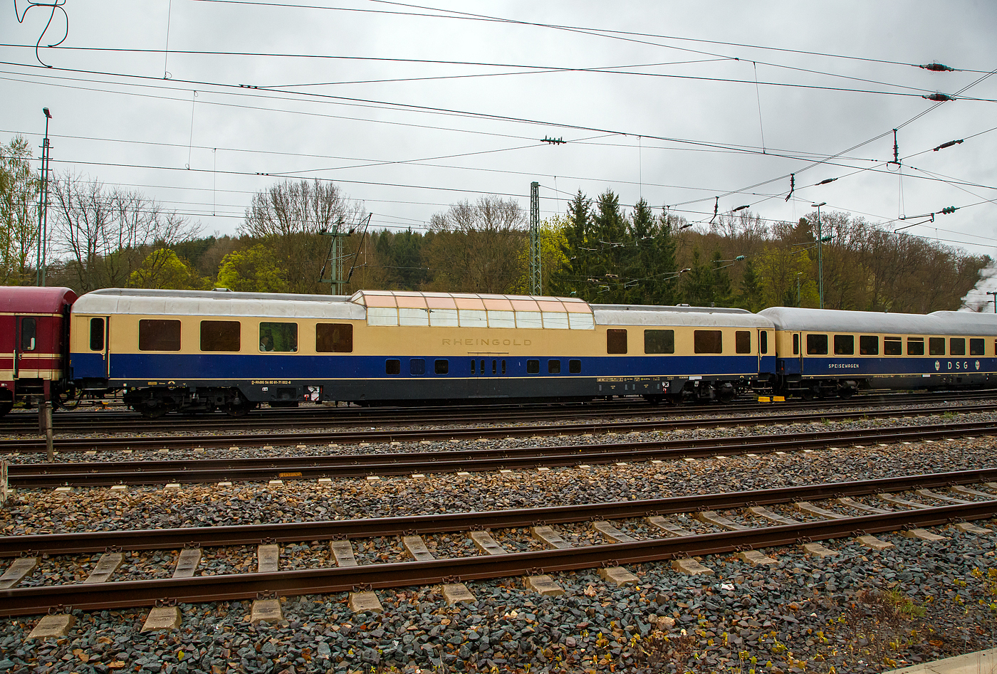 Der historische Rheingold-Aussichtswagen/Panoramawagen (DomCar) D-RhBG 56 80 81-71 002-8 der Gattung ADm, der Rheingold-Zug Betriebsgesellschaft mbH, eingereiht im Zugverband in einen Sonderzug, hier am 22 April 2017 in Au/Sieg.

Bei dem Aussichtswagen der Gattung SRmz, handelt es sich um das ehemalige DomeCar DB 10 432 AD4üm-62 als 1. Klasse Aussichtswagen für den Fernschnellzug Rheingold (F-Zug), der 1962 von Wegmann & Co. in Kassel unter der Fabriknummer 6656 gebaut wurde. Ab 1966 Deutsche Bundesbahn - DB 10 532 AD4ümh 101und später DB 61 80 88-80 002-0 ADmh 101. Fünf dieser Aussichtswagen im Stil der US-amerikanischen Domecars wurden von Wegmann für die Deutschen Bundesbahn (DB) gebaut, die sie für luxuriösen Fernschnellzug Rheingold, der ausschließlich die 1. Klasse führte, beschaffte. Zwei für jedes Zugpaar und ein weiterer Wagen dient als Betriebsreserve.

1963 wurden zwei nahezu baugleiche Wagen für den Rheinpfeil in Betrieb genommen, äußerlich an den größeren Panoramafenstern (vier statt acht) erkennbar. Sie hatten die abweichende Gattungsbezeichnung AD4üm-63, außerdem trugen sie ursprünglich statt des Rheingold-Schriftzuges die Anschrift „Deutsche Bundesbahn“. 1965 wurden beide Züge zu Trans-Europ-Express-Zügen (TEE) heraufgestuft.

Ab 1971 wurden die TEE-Züge in Deutschland weitestgehend in das neu geschaffene Intercity-Netz integriert und der fahrplanmäßige Einsatz der Aussichtswagen 1973 beendet. 1976 wurden sie an die Internationale Apfelpfeil-Organisation (IAO, mit vollem Namen IAO Internationale Apfelfahrten Organisation Helmut Th.K.Rall International Arrangements Organization GmbH & Co. KG, besser bekannt als Apfelpfeil), einen Reiseveranstalter mit Sitz in Freudenstadt-Grüntal, verkauft. Die IAO baute die Kuppeln um und verringerte deren Höhe um 20 cm, was den Fahrzeugen ein Lichtraumprofil gab, das deren freizügigen Einsatz in ganz Europa ermöglichte. Als die IAO in die Insolvenz fiel, kaufte das Reisebüro Mittelthurgau die Fahrzeuge, ertüchtigte sie für den Einsatz mit 200 km/h und vermarktete mit ihnen Schienenkreuzfahrten unter der Marke TEE Panorama. Anschließend 1999 wurden sie an die Veolia-Tochter Tågkompaniet verkauft, die sie als AFS1 bzw. AFS2 (mit Notbremsüberbrückung) mit den Nummern 201 bis 205 bezeichnete. Die Wagen wurden weiß-grün foliert und mit großen Tierbildern versehen: Vielfraß (201), Fuchs (202), Luchs (203), Elch (204) und Bär (205). So verkehrten die Wagen von 1999 bis 2003 zwischen Stockholm und Narvik.

Dann wurden die Wagen einzeln an unterschiedliche Eigentümer veräußert:
Nr. 10551 kam 2005 zu einem Reiseveranstalter in den Niederlanden.
Nr. 10552 übernahm der Freundeskreis Eisenbahn Köln und unterhält ihn betriebsfähig (dieser hier), aber nur noch für eine Höchstgeschwindigkeit von 160 km/h. 
Nr. 10553 wurde von der Vulkan-Eifel-Bahn Betriebsgesellschaft (VEB) übernommen. Im April 2011 kaufte ihn das Eisenbahnverkehrsunternehmen RailAdventure für 40.000 Euro, sanierte ihn in mehrjähriger Arbeit grundlegend und baute ihn dabei zu einem modernen Salonwagen um.
Nr.10554 wurde ebenfalls von der VEB übernommen, später von der AKE-Eisenbahntouristik gekauft und dort im AKE-Rheingold eingesetzt.
Nr. 10555 übernahm die Deutsche Bahn Stiftung, Trägerin der Museen der DB AG. Er steht als Info-Zentrum im Güterbahnhof Coburg.

LENENSLAUF von diesem Wagen (Nr. 10552):
• 1962 bis 1966 - DB 10 432 AD4üm-62
• 1966 bis 1971 - DB 10 552 AD4üm-63
• 1971 bis 1976 - DB 61 80 81-80 002-0 ADmh 101
• 1976 bis 1989 - IAO (Apfelpfeil) 51 80 09-42 912-8 WGm
• 1989 bis 1999 - RBMT (Reisebüro Mittelthurgau) 51 80 09-80 202-7 WGm 038.8, eingestellt über die SBB
• 1999 bis 2005 - TKAB AFS 1 – 202 „Fuchs“ (Veolia-Tochter Svenska Tågkompaniet AB), 
2005 bis 2008 - ADümh101 56 80 81-80 002-7 (Privateigentum, Leihgabe an FEK - Freundeskreis Eisenbahn Köln e.V.)
seit 2008 - D-RhBG 56 80 81-71 002-8 ADm der Rheingold-Zug Betriebsgesellschaft mbH

TECHNISCHE DATEN (DomeCar):
Spurweite: 1.435 mm
Anzahl der Achsen: 4 in 2 Drehgestellen
Länge über Puffer: 26.400 mm
Drehzapfenabstand: 19.000 mm
Eigengewicht: 51,4 t
Höchstgeschwindigkeit: 160 km/h (zeitweise 200 km/h)
Ausstattung: Aussichtskanzel mit 3 Tischen á 4 Personen, 3 Tischen á 2 Personen, 4 Tische für Einzelpersonen, 2 Abteile 1. Klasse mit 6 Plätzen. Bar- und Speiseraum mit 4 Tischen á 2 Personen, Bar, Sitzgruppe, WC, Abstell- und Kühlmöglichkeit im Untergeschoss.
