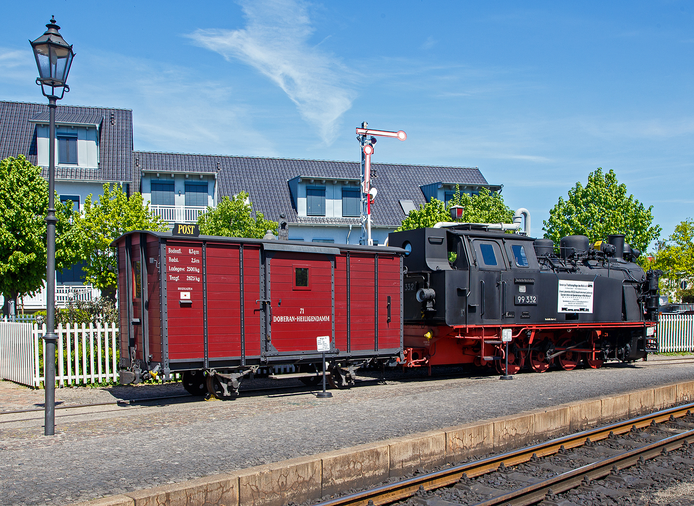 Der historische zweiachsige Postwagen 71 der damaligen DHE - Doberan-Heiligendammer-Eisenbahn (Vorgänger MBB - Mecklenburgischen Bäderbahn Molli), ex DR 98-84-01 ab-/ausgestellt im Bahnhof Ostseebad Kühlungsborn-West (bis 1938 Ostseebad Arendsee), hier am 15.05.2022. Der Wagen ist Eigentum und Leihgabe vom VTM.

Der Post-/ Packwagen wurde 1886 von der Waggonfabrik P. Herbrand & Cie. in Köln-Ehrenfeld gebaut und an die damalige Doberan-Heiligendammer-Eisenbahn (DHE) geliefert. Eine Rekonstruktion erfolgte 2000 – 2001 durch den Verein zur Traditionspflege des Molli e. V..

Die DHE wurde im März 1890 verstaatlichte und in die Großherzoglich Mecklenburgische Friedrich-Franz-Eisenbahn eingliedert. Ab dem 1. April 1920 gehörte sie zur Deutschen Reichsbahn. So kam der Molli nach der deutschen Wiedervereinigung zur DB AG. Zum 01.10.1995 wurde die Mecklenburgische Bäderbahn Molli GmbH gegründet und übernahm fortan die 15,4 km lange Strecke zwischen Kühlungsborn und Bad Doberan von der Deutschen Bahn AG.

TECHNISCH DATEN des Wagens:
Spurweite: 900 mm
Gattung: P
Anzahl der Achsen: 2
Drehzapfenabstand: 2.500 mm
Ladefläche: 8,3 m²
Tragfähigkeit: 2.625 kg

Rechts davor die Molli Museums-/Denkmaldampflok MBB 99 332, eine LKM Typ 225 PS, 900 mm Schmalspurlok, der Mecklenburgischen Bäderbahn Molli GmbH, ex DB 099 905, ex DR 99 2332, ex DR 99 332, ex Wismut 44, am 15.05.2022 beim Bahnhof Ostseebad Kühlungsborn West.

Die 900 mm-Schmalspur-Dampflok der DR-Baureihe 99.33 wurde1951 von LKM (VEB Lokomotivbau Karl Marx Babelsberg) unter der Fabriknummer 30013 gebaut und an die SDAG Wismut (Sowjetisch-Deutsche Aktiengesellschaft Wismut), für die Haldenbahn Oberschlema, (Aue) als Wismut 44 geliefert. Neben zwei weiteren Loks, wurde diese Lokomotive 1958 durch die Deutsche Reichsbahn, für die Bäderbahn Molli, erworben und nach Anpassungsarbeiten im Reichsbahnausbesserungswerk Görlitz als DR 99 332 in Dienst gestellt. Im Jahr 1961 wurden die 99 331 und die 99 332, im RAW Görlitz, auf Heißdampf umgebaut. Die 99 333 blieb eine Nassdampflokomotive und war ab Mitte der 1960er Jahre nur noch Reservemaschine. Mit der Einstellung des Güterverkehrs auf der Strecke wurden nicht mehr so viele Lokomotiven benötigt, so dass diese 1968 ausgemustert wurde.

1970 erfolgte die Umzeichnung in DR 99 2332-7 und 1992 in DR 099 905-2. Nachdem Zusammenschluss beider Deutscher Bahnen zum 01.01.94 wurde sie zur DB 099 905-2. So ging sie zum 01.10.1995, mit der Übernahme des Betriebs auf der Strecke durch die Molli - Mecklenburgische Bäderbahn Molli GmbH, an diese über. Mit der Übernahme wurde auch ein neues Betriebskonzept eingeführt, das die Unterhaltung von zwei noch vorhandenen Lokomotiven der BR 99.33 nicht mehr notwendig machte, so erfolgte zum 07.05.1996 die Außerdienststellung.

Die Schmalspur-Dampf-Lokomotiven des Typs 225 PS Schmalspur des VEB Lokomotivbau Karl Marx wurden basierend auf einem Typenprogramm für kleinere Dampflokomotiven speziell für den Einsatz bei Industriebetrieben entwickelt. Drei dieser Lokomotiven wurden 1958 durch die Deutsche Reichsbahn von der SDAG Wismut erworben. 

Konstruktive Merkmale:
Die Lokomotiven verfügen über einen geschweißten Blechrahmen. Auf dem geschweißten Langkessel sitzt vorn der Dampfdom. Auf dem hinteren Teil sitzen der Sandkasten sowie zwei Kesselsicherheitsventile der Bauart Ackermann. 1961 wurden die 99 331 und die 99 332 auf Heißdampf umgebaut. Dabei erhielten die Kessel jeweils 9 Heiz- und 64 Rauchrohre. Das außen liegende waagerecht angeordnete Zweizylinder-Triebwerk wirkt auf die dritte Kuppelachse. Die außen liegende Heusinger-Steuerung besitzt eine stark vereinfachte Kuhnsche Schleife.

Für die Zugbeleuchtung erhielten die Lokomotiven bei den Anpassungsarbeiten der Deutschen Reichsbahn einen leistungsstärkeren 5 kW Turbogenerator hinter dem Schornstein. Die ursprüngliche Handbremse wurde um eine Knorr-Druckluftbremse ergänzt. Die zweistufige Luftpumpe sitzt rechts neben der Rauchkammer. Die Lokomotiven erhielten wie auf der Bäderbahn üblich ein Knorr-Druckluftläutewerk. Gesandet werden der erste Radsatz von vorn und der letzte Radsatz von hinten.

Für den Einsatz auf der Bäderbahn wurde der obere Teil des Führerhauses stark abgeschrägt, um es an das Lichtraumprofil anzupassen. Das Dach erhielt seitliche Regenrinnen mit Ablaufrohren. Die geschweißten Wasserkästen befinden sich vor dem Führerhaus auf beiden Seiten des Kessels und fassen 3,4 m³. Der Kohlenkasten befindet sich an der Rückwand des Führerhauses und war ursprünglich, da für Braunkohlebrikettfeuerung ausgelegt, mit einem Aufbau vergrößert, der zwischen den beiden Fenstern der Rückwand eingezogen bis auf Höhe des Daches geführt wurde. Er hatte ein Fassungsvermögen von 2,2 t. Da mittlerweile die Feuerung mit Steinkohle erfolgt und bei deren höherem spezifischen Gewicht der Kohlekasten nicht voll gefüllt werden konnte, wurde dieser Aufbau bei 99 2331 bei der Hauptuntersuchung 2004 im Dampflokwerk Meiningen zur Verbesserung der Sicht bei Rückwärtsfahrt entfernt. Sein Fassungsvermögen reduzierte sich dadurch auf 1,5 t. Die, hier gezeigte Museumslok 99 2332 hat noch den ursprünglichen Aufbau.

TECHNISCHE DATEN:
Spurweite: 900 mm 
Achsformel: D h2t
Gattung:  K 44.8
Länge über Kupplung: 8.860 mm
Höhe: 3.490 mm
Achsabstand: 3 x 1.000 mm = 3.000 mm
Leergewicht: 25,0 t
Dienstgewicht: 32,4 t
Höchstgeschwindigkeit: 35 km/h
Indizierte Leistung: 460 PSi
Anfahrzugkraft: 56,39 kN
Kuppelraddurchmesser: 800 mm
Steuerungsart: Heusinger
Zylinderanzahl: 2
Zylinderdurchmesser: 370 mm
Kolbenhub: 400 mm
Kesselüberdruck: 14 bar
Anzahl der Heizrohre:  9
Anzahl der Rauchrohre: 64
Heizrohrlänge: 2.600 mm
Rostfläche: 1,6 m²
Strahlungsheizfläche:  6,04 m²
Rohrheizfläche:  36,85 m²
Strahlungsheizfläche:  6,04 m²
Rohrheizfläche: 36,85 m²
Überhitzerfläche: 18 m²
Verdampfungsheizfläche: 42,89 m²
Wasservorrat: 3,4 m³
Brennstoffvorrat: 2,2 t Kohle
